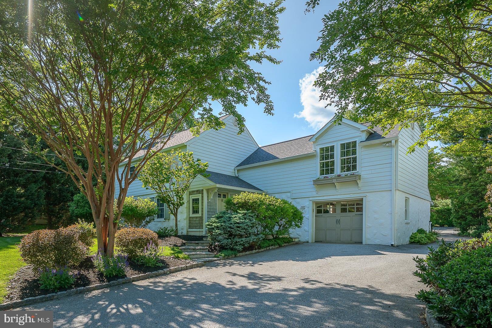 A winding flagstone path leads to the front door of this idyllic painted-white Colonial, where classic farmhouse styling is enhanced by charming cedar shake accents and beautifully curated landscaping.
Inside, a stone-floored foyer offers an immediate glimpse of the home's thoughtfully designed living spaces. Rich hardwood floors extend throughout both the first and second levels, lending warmth and continuity throughout the home. The formal living room is both sophisticated and welcoming, with moody navy walls, extensive custom shelving, and a centrally positioned fireplace that creates a natural gathering place.
A wide cased opening connects to the dining area and continues into the heart of the home—a stunning sun-filled kitchen where sea glass-hued cabinetry pairs beautifully with white quartzite countertops and brushed gold hardware. Skylights, a wall of windows, and French doors bathe the space in natural light while opening to a deep flagstone terrace designed for effortless indoor-outdoor living. A suite of premium appliances, including a Sub-Zero refrigerator and freezer, four-burner gas range with griddle, farmhouse sink, and illuminated display cabinetry, combines exceptional function with timeless style.
Just beyond, the spacious family room features a vaulted ceiling, fireplace, decorative paneling, and sliding doors that open to a second terrace shaded by mature canopy trees. A generously sized mudroom with family entrance provides direct access to the attached garage, while a beautifully appointed powder room with vessel sink completes the main level.
Upstairs, the primary suite offers a peaceful retreat. The bright white bath features a seated shower, washstand-height vanity, and window for natural light. Exceptional storage includes a wall of double closets flanking the suite entrance, along with an additional fully outfitted closet providing exceptional storage space. Three additional bedrooms share an updated  hall bath with tub shower and ample hallway storage; select family bedrooms feature carpeting underfoot, offering an added layer of comfort and coziness.
The lower level is designed for the rhythms of everyday life, offering a large recreation and television area with plenty of room for exercise equipment, hobbies, or play. A spacious laundry room is equally well considered, featuring lacquered cabinetry and expansive folding counters.
The backyard is truly one of the home's most enchanting features. A stone terrace spans the full length of the house, creating multiple spaces for dining, entertaining, and relaxing. Beyond, a storybook archway draped in climbing roses opens to lush gardens and an exceptionally deep rear lawn. With room for play, gatherings around a fire pit, and convenient shed storage, the grounds offer a rare sense of space, beauty, and possibility.
Beautifully updated yet rich in character, this is a home that feels both timeless and effortlessly welcoming—a truly idyllic setting for everyday living.