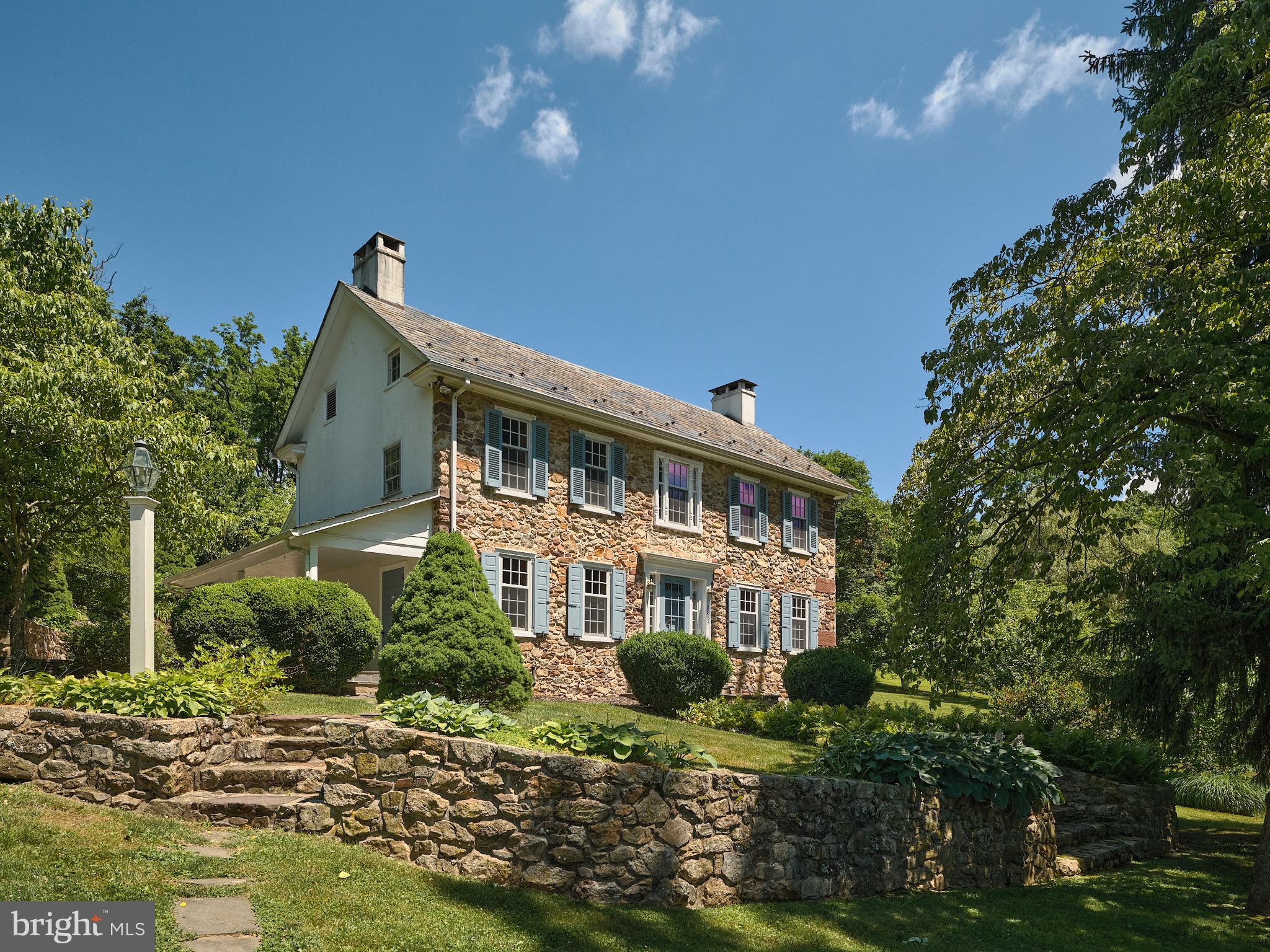 Welcome to this enchanting Bucks County stone farmhouse, gracefully standing at the top of a serene hilltop with sweeping lawns and parklike setting. The approach to the home is truly spectacular beginning with a gated stone entry with a paved driveway bordered with flowering trees that sets the tone for the elegance within. This 4 bedroom 4 bath home sits on 20 acres and is the perfect blend of historical charm and modern luxury. Step into the heart of the home- a completely remodeled kitchen and great room with vaulted ceilings with exposed beams, flooded with natural light from the large windows offering views of the gardens from every angle.  Anchored by a brick fireplace the room is spacious and inviting. The brick floored hallways offer a seamless connection to the original sections of the house dating back to 1820. Steeped in history, the rooms feature pumpkin pine floors, walk-in fireplaces, original built-ins and moldings, and beamed ceilings offering a cozy setting for intimate dinners and gatherings. The upstairs hosts two spacious bedrooms and a full bath, providing a tranquil retreat. Below the kitchen, you'll find two additional guest rooms, each with ensuite bathrooms, all recently updated for modern comfort. There is an additional loft space that could act as a 5th bedroom or office. Outside, the property features a stunning stone bank barn,  a two-car detached garage, smoke house and spring house. Multiple stone patios, and decks to enjoy year round.  The backyard is a nature lover's paradise, with multiple tiered gardens, specimen plantings, partly wooded areas, perfect for nature trails and exploration.