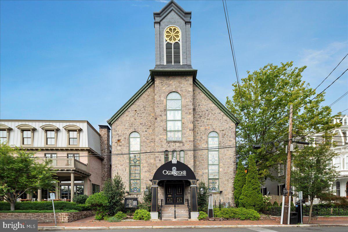The distinguished structure now home to Oldestone Steakhouse began its life in 1873–1874 as the New Hope Methodist Episcopal Church, later known as the New Hope United Methodist Church. Built on land purchased for $600, it stood between two other historic landmarks—the Logan Inn and the Crook home, now the Mansion Inn. Designed by architect James Bird and constructed with the stonework of mason Peter S. Naylor, the building was valued at $14,000 upon completion. Its Gothic sandstone façade, soaring ceilings, and intricate stained glass windows made it an architectural treasure from the day it opened.
The church replaced an earlier wood-frame Methodist church on Mechanic Street, which had fallen into disrepair. While no photographs of the original structure are known to exist, its cemetery remains adjacent to the municipal parking lot. For 125 years, the building served as a spiritual center for New Hope’s Methodist community. Its congregation included both African Methodist Episcopal members in the early 1800s and white Methodist groups by the 1830s, reflecting the religious diversity and energy of the Second Great Awakening, a revival movement that swept America between 1795 and 1835. The final service in the building was held in 1999, after which the congregation relocated to Solebury.
Following its closure as a church, the building entered a new chapter as Marsha Brown’s, a Creole-inspired fine dining restaurant that operated for nearly two decades. Known for its dramatic ambiance and refined cuisine, Marsha Brown’s became a dining destination in New Hope before closing during the COVID-19 pandemic. In 2021, the space was reimagined as Oldestone Steakhouse, a modern metropolitan steakhouse that honors the building’s architectural grandeur while offering USDA Prime steaks, fresh seafood, and craft cocktails. Many of the original features remain intact, including the stained glass windows, repurposed church pews, a striking 30-foot mural titled Redemption by Russian artist Valeriy Belenikin, chandeliers featured in John Wick 3, and a speakeasy-style jazz lounge on the third floor.  New Hope itself has a rich history dating back 10,000 years, when the Lenni-Lenape Native Americans settled along the Delaware River. In the early 1700s, William Penn authorized land sales that led to the founding of the town. Originally known as Coryell’s Ferry, the area became a vital crossing point on Old York Road, the main route between Philadelphia and New York City. George Washington lodged in New Hope the night before his famous crossing of the Delaware River in 1776 and later ordered the ferry destroyed to prevent British pursuit. The town endured shelling during the Revolutionary War, and some buildings are still said to contain unexploded ordnance in their rafters.  In the 19th century, the opening of the Delaware Canal in 1832 transformed New Hope into a thriving trade hub. Officially incorporated in 1837 after a devastating fire destroyed Benjamin Parry’s mills, the rebuilt town was seen as a “new hope” for the community, giving rise to its name. The 20th century brought a cultural renaissance, with New Hope becoming a haven for Pennsylvania Impressionist painters such as Daniel Garber and Edward Redfield, and the Bucks County Playhouse, opened in 1939, attracting theatrical luminaries including Helen Hayes, George C. Scott, and Robert Redford. In 2002, New Hope made history again by becoming the first borough in Pennsylvania to ban discrimination based on sexual orientation and gender identity. Today, the building  remains an integral part of New Hope’s living history. Preserved through the work of the New Hope Historical Society, it stands as a testament to the town’s evolution from a colonial ferry crossing to a vibrant cultural and culinary destination. Its transformation from church to celebrated restaurant captures both the spirit of preservation and the creativity that defines New Hope!