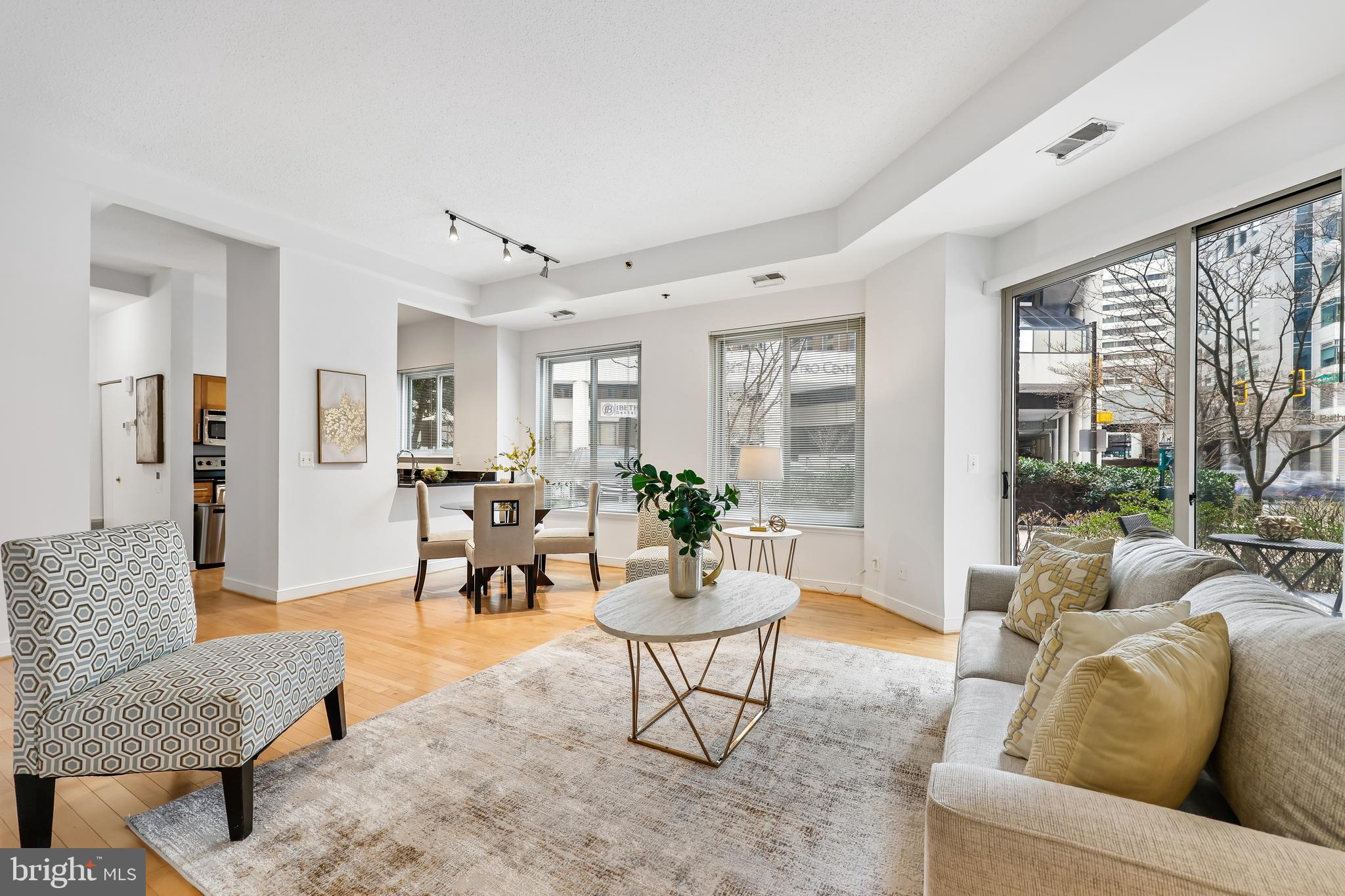 Experience effortless urban living in this thoughtfully maintained 2-bedroom, 2-bathroom main-level condo situated in the heart of downtown Bethesda. The freshly painted interior welcomes you, with soaring high ceilings and rich hardwood floors that flow through the main living area. Natural light pours into the open living and dining space through expansive windows, while a sliding glass door leads to a patio offering walkout accessibility directly to the street. The updated kitchen features stainless steel appliances and a convenient kitchen hatch, ensuring seamless entertaining and easy access to the dining area. The split-bedroom floor plan provides maximum privacy, featuring two generously sized bedrooms finished with wall-to-wall carpeting and ample closet space. This prime location offers an unparalleled lifestyle of convenience; you are positioned directly across from the Bethesda Metro station and bus terminal, and just blocks away from the area's premier dining, boutique shopping, and entertainment venues. For outdoor enthusiasts, the renowned Capital Crescent Trail is only a short distance away, offering miles of scenic walking and biking paths.
