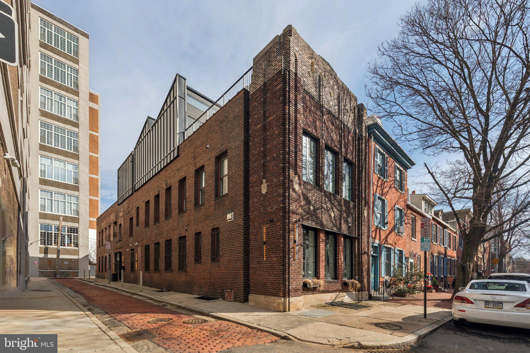Positioned on a rare corner lot in the heart of Fitler Square, 207 S 24th Street is a truly one-of-a-kind residence filled with natural light from three exposures and defined by striking architectural character. Originally reimagined from a historic brick structure, the home blends dramatic loft-like volume with warm modern finishes, featuring exposed wood beams, steel staircases, and walls of original brick. Originally reimagined from a historic brick structure, the home offers striking industrial elements; exposed original wood beams, soaring ceilings, steel staircases, and walls of brick, balanced with warm finishes and modern functionality. Enter through a welcoming foyer with terra cotta floors, built-in coat and shoe storage, a walk-in pantry, and a convenient powder room. The main living level opens into a light-filled chef’s kitchen with abundant custom cabinetry, expansive countertops, and a central island, all framed by the warmth of exposed beams above. The space flows effortlessly into a generous dining area comfortably suited for large gatherings before opening to the expansive living room, where textured plaster walls, custom built-ins, and windows on two exposures create an inviting atmosphere. This level is completed by a laundry room with a dedicated dog wash and direct access to the rare convenience of a two-car garage. A striking open steel staircase leads to a dramatic mezzanine-style flex space overlooking the levels below. With open beams and a glass-enclosed phone booth, this area serves beautifully as an office, studio, or additional lounge. Privately tucked beyond is the primary suite, featuring oversized windows, a walk-in closet, and a spa-like bathroom with plaster walls and ceiling, a clawfoot soaking tub, oversized frameless rain shower, and separate water closet. The opposite wing of this floor offers three additional bedrooms and a den. Two bedrooms share a spacious ensuite bath with double vanity and tub/shower combination, while the third bedroom enjoys its own private ensuite bath. A hall linen closet adds additional storage. The newly constructed third level creates an ideal entertaining and guest retreat with an open living area, a full bathroom with tiled shower, and an additional guest suite. Just outside the sliding glass doors is a sprawling roof deck that offers the perfect setting for outdoor dining, lounging, or entertaining. Located just steps from Fitler Square Park, the Schuylkill River Trail, neighborhood cafés, and Rittenhouse Square, this remarkable home offers a rare blend of architectural history, modern updates, and flexible living in one of Philadelphia’s most sought-after neighborhoods.