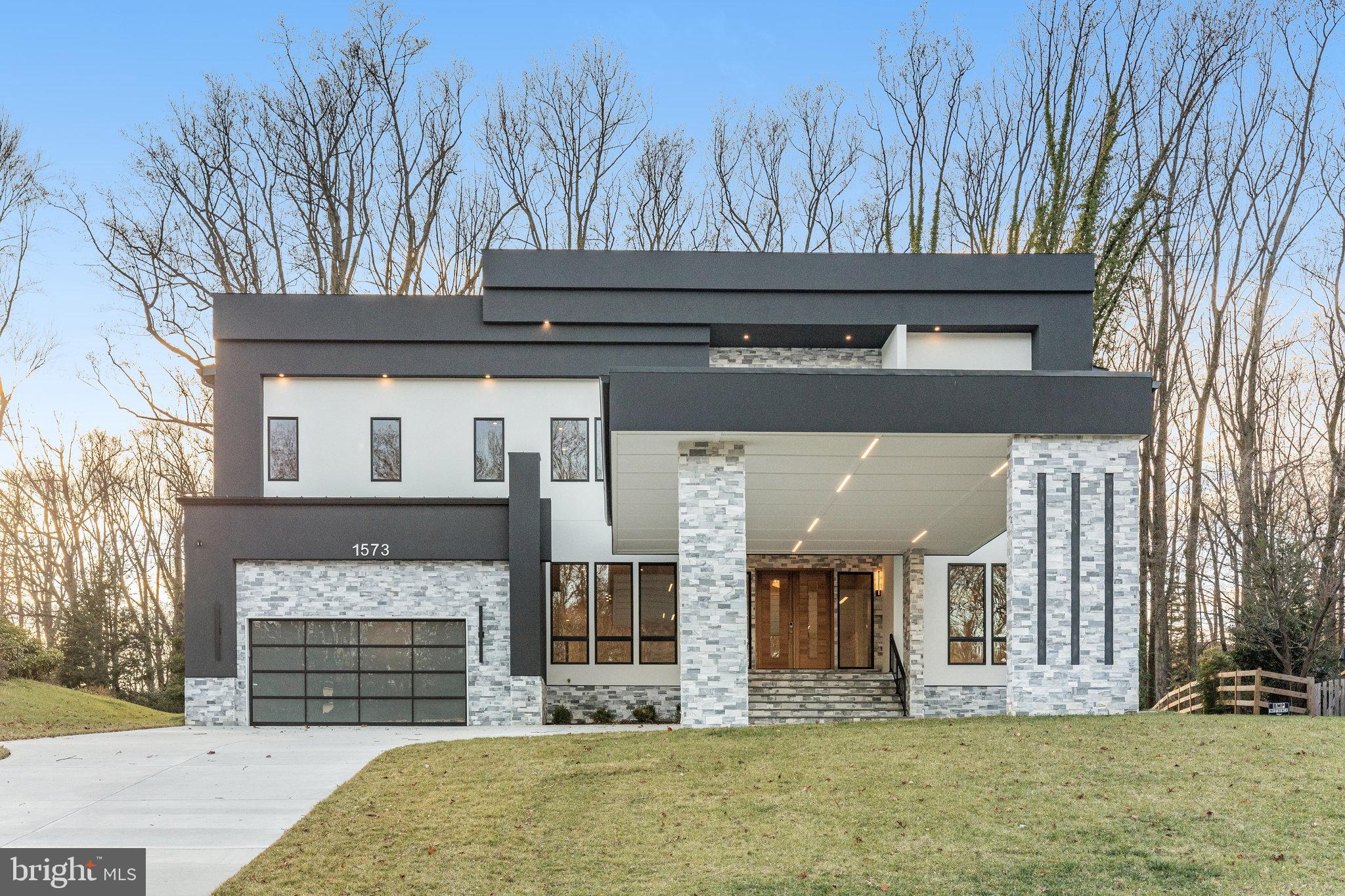 This distinctive modern home,  is a perfect blend of contrast and luxury. Spanning 10423 SqFt over three levels, it offers a spacious living environment that seamlessly combines comfort with sleek, contemporary design. The entrance sets the tone with a custom-made solid wood door, flanked by side light panels and elegant sconces, inviting you into the stylish interior. The foyer, open to the second floor, guides you inside where the open-plan kitchen and family rooms serve as the home's hub.
The kitchen features professional  appliances, including a six-burner gas stove top and wall oven, and two-tiered, white designer cabinetry with under-cabinet lighting, accented with black and brushed brass drawer pulls and knobs. The kitchen island is constructed of marble on three sides, contrasting cabinetry, and includes a prep sink, microwave, and dishwasher, all illuminated by pendant lighting with brushed brass accents. The tiered ceilings with LED recessed lighting add to the modern aesthetic.
In the family room, an elegant floor-to-ceiling stone gas fireplace with a wood mantle and side shelving serves as a focal point. French doors provide seamless connectivity to the outdoors, leading to a covered porch perfect for relaxation or entertaining. An additional entrance to the main part of the home is through the professionally appointed prep kitchen,  conveniently located next to the walk-in pantry. The car garage is accessible through the mudroom, which boasts a tiled floor, built-in bench, and coat rack. An ensuite bedroom on this level offers privacy and luxury, with a floor-to-ceiling tiled shower and custom closets.

The second-floor landing features built-in shelves and an entertainment center, with the natural finish of the shelves contrasting against dark painted accents and complemented by under-cabinet lighting. The centerpiece of the second floor is the luxuriously appointed owner's suite. This oversized bedroom includes a separate seating area and Anderson Lifestyle black double French doors that open to a large private balcony, ideal for relaxing or intimate al fresco dining. A gas fireplace with a wooden mantel, tiered ceiling with recessed lighting, a crystal tiered chandelier, and a ceiling fan add both comfort and elegance. The walk-in closets are oversized and complete with built-in shelves and drawers. The spa-like bath includes a marble floor, dual vanities with smart-controlled heating and an aroma diffuser, a standalone bathtub, and an oversized shower equipped with multiple shower heads, a seamless glass enclosure, a built-in bench, and a steam bath feature for ultimate relaxation. The laundry room is both practical and sophisticated, with tiled flooring, ample cabinetry, and a built-in drying rack. All other bedrooms on this floor are ensuite, featuring custom walk-in closets and bathrooms with tile floors and marble countertops.

The lower level offers a seamless blend of functionality and luxury, ideal for both relaxation and social gatherings. The recreation room features a sophisticated wet bar and a cozy stone fireplace, complemented by plush carpeting and elegant paneling. The media room, with its tiered seating and advanced sound system, promises an immersive cinematic experience. Additionally, the lower level includes an extra bedroom and an exercise room, catering to both comfort and wellness. A bonus room under the deck adds to the home's versatility.

The architecture of this modern home reflects a harmony between bold contrasts and luxurious simplicity. Ideally located with access to all major freeways, Tysons Metro, and Tysons Mall, this home is a prime example of contemporary living at its finest.
