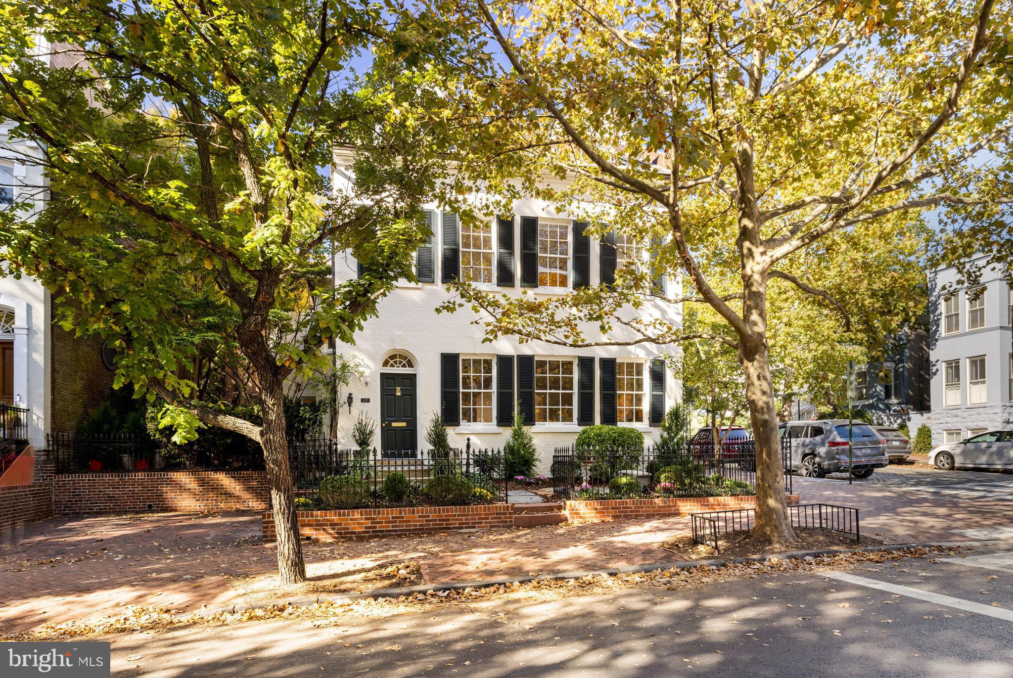 Over the last 300 years this house has served a succession of Georgetown families and has always been known as “The Yellow House.” It is easy to see why so many have called this house home for hundreds of years, with each generation contributing meaningful updates that reflect the spirit of their time, every family has left its distinct mark, enhancing the house while preserving its charm for the next owners.

The ground floor of this exceptional house is a true standout, offering impressive size, well-balanced proportions, and abundant natural light. The living room is truly noteworthy with its generous scale and abundant light. As a detached home, this room enjoys multiple exposures, maximizing natural light throughout the day. Anchored by a wood-burning fireplace framed by a period mantel, the room is further brightened by three oversized, east-facing windows that flood the space with morning sunlight. The living room flows seamlessly into a spacious library, which boasts its own wood-burning fireplace with an original mantel. Nearby, the charming dining room, with French doors opening to the terrace and garden, provides an inviting setting for entertaining, both indoor and out. The expansive eat-in kitchen is a timeless classic designed to meet the needs of the modern cook. It features a commercial-grade Wolf range with a grill and a powerful commercial hood as well as other cook-friendly features like a warming drawer, a pot-filler faucet, and a hot water dispenser. Another set of elegant French doors connects the kitchen to the terrace, creating a smooth flow between indoor and outdoor living spaces. Adjacent to the kitchen, a cozy family room is enriched by a century-old Palladian window. The home also includes the convenience of a large powder room and coat closet on the main level, along with an elevator for easy access to all floors, ensuring both comfort and accessibility throughout.

The second floor is just as remarkable as the first. The primary bedroom, located in the northeast corner, offers stunning views of Georgetown and open skies. A working fireplace adds warmth and charm to this already impressive retreat. The crown jewel is the colossal modern marble bath, an oasis of luxury that boasts two expansive vanities, a shower with multiple body spray nozzles, a grand soaking tub, and a private commode room. Off the bath, a massive double walk-in closet provides ample space. This floor also includes two additional spacious bedrooms, each with its own full bath, and a convenient upstairs laundry room, perfectly blending comfort and practicality.

Up the stairs to the third level the staircase splits in two directions—one leading east, the other west—creating distinct, private spaces. The eastern bedroom exudes charm, featuring dormer windows and an ensuite half bath that could easily be expanded into a full. A delightful touch of history remains, as Dr. Appleby’s son, whose family lived here for many years, carved his name into one of the dormers. The western bedroom is a light-filled suite, full of character and history. Once serving as the map room of World War II General Jacob “Jake” Devers. This spacious suite features two walk-in closets, large windows with dual exposures, its own private bathroom, and climate control. It’s a perfect blend of historical significance and modern comfort.

The full-sized basement has ample storage, a second laundry area, another powder room, and direct access to the convenient two-car parking. The exterior is equally impressive. The front yard enclosed by an antique wrought iron fence adds both privacy and curb appeal. The side yard and terrace provide a secluded space with easy access from the dining room and kitchen—ideal for entertaining. The terrace features mature plantings, a brick-paved courtyard, and a stylish arbor. At the rear, a private alley leads to a secure door opening to P Street, ensuring both convenience and privacy.