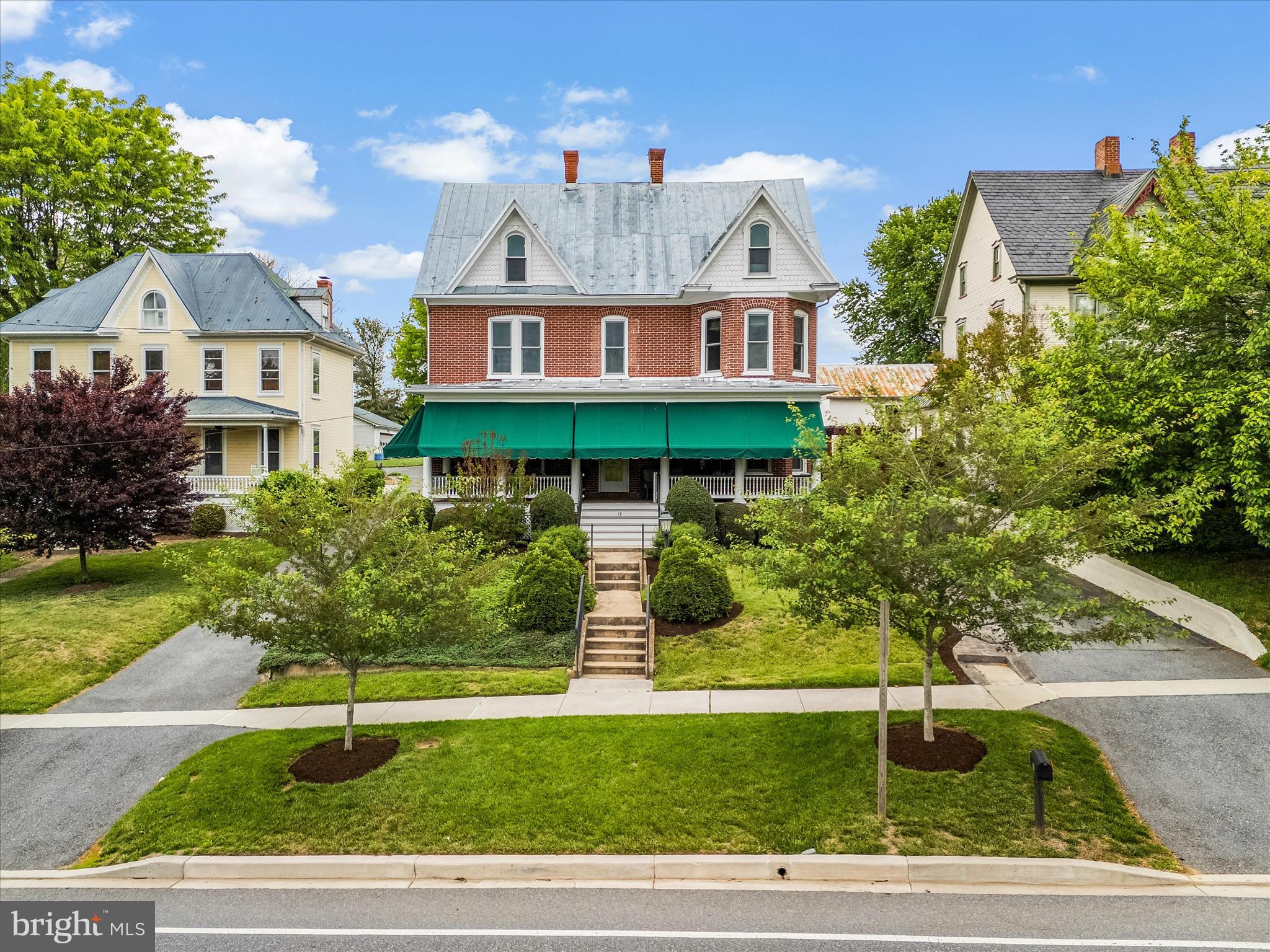 Carefully reimagined between 2018 and 2021, this historic Main Street home now lives like a luxury boutique retreat hidden in the heart of Middletown — complete with a secret speakeasy concealed behind a swinging bookshelf, a breathtaking custom kitchen addition, and a covered courtyard entertaining area anchored by a stunning stone fireplace. Rich in history yet thoughtfully transformed for modern luxury living, this extraordinary four-bedroom residence with dedicated office space blends timeless craftsmanship with sophisticated design rarely found in historic homes. Perched above historic Main Street with sunset views toward South Mountain, the home showcases soaring ceilings, original architectural details, custom Mennonite-crafted millwork, designer Circa lighting, and extensive infrastructure updates throughout.

At the heart of the home is the stunning kitchen addition featuring exposed historic brick, dramatic steel scissor-beam trusses, handcrafted cabinetry, quartz perimeter counters, granite center island, GE Monogram appliances, farmhouse sink, induction cooktop, and a dramatic picture window overlooking the beautifully landscaped courtyard and covered side porch. The original kitchen was transformed into a spacious dining room, creating exceptional flow for entertaining while preserving the home’s historic character. Outdoor living spaces feel like an extension of the home itself with stamped concrete, custom stone fireplace, a covered entertaining area, integrated storage, and beautifully landscaped gathering spaces designed for both intimate evenings and large-scale entertaining.

The front parlor was transformed into a stunning library with built-in shelving, restored historic shutters, statement lighting, and the hidden swinging bookshelf leading to the speakeasy featuring a solid wood bar, wet bar, beverage refrigerator, custom ceiling paneling, and dramatic finishes. The family room was created by opening two original parlors and is crowned by a dramatic bay window that floods the space with natural light.

Upstairs, the home offers two primary suites along with spacious secondary bedrooms featuring exceptional flexibility, including a custom Murphy bed/work table system and built-in bay window seating. A dedicated office conceals a hidden opening into an untouched portion of the original home, creating a fascinating preserved time capsule rarely found in homes of this era. A covered upper porch overlooks the courtyard below, while the redesigned laundry room introduces marble countertops, statement lighting, and additional storage.

The finished attic was transformed into a truly unique owner’s retreat featuring reclaimed oak flooring, exposed brick chimneys, preserved historic wall surfaces, dressing room, laundry chute, separate staircase access, and a spa-inspired bath with a hidden Japanese-inspired Ofuro soaking tub room.

Infrastructure improvements include dedicated high-end Carrier HVAC systems with hospital-grade filtration and smart thermostats, radiant heated floors, replaced electrical systems in 2020, updated copper plumbing, Japanese toilets, hand-tooled standing seam metal roof, replacement gutters, energy-efficient wooden sash windows, composite porch decking, central vacuum, Sonos integration, and extensive custom woodworking throughout.

Stretching from Main Street to West Green Street, the property also includes a subdivided, buildable rear lot. The purchaser of 19 E Main Street will have first right of refusal on the lot, which is also available separately, creating a rare opportunity for future expansion or investment in the heart of Middletown.

Located on one of Maryland’s historic designated Main Streets, just steps from Middletown’s restaurants, library, shops, parks, & sought-after schools, this extraordinary residence offers a lifestyle as rare as the home itself.  Owned by only three families in 100+ years, this one-of-a-kind home blends history, luxury, & craftsmanship.