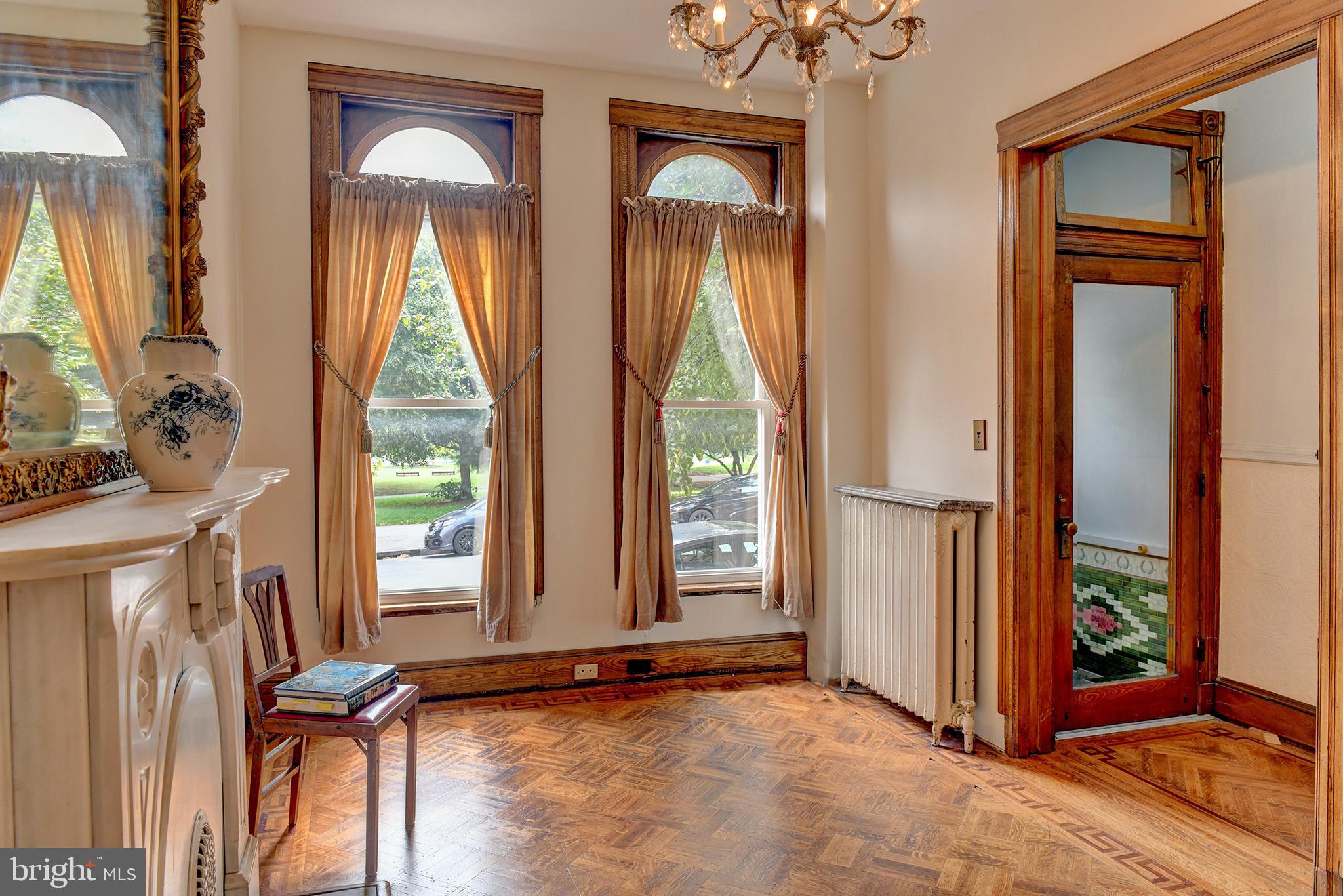 In a city crowded with countless row houses on narrow streets, you’ll appreciate this generous residence. Welcome to 2744 E Baltimore Street, an iconic home overlooking Patterson Park, where historic charm and city living come together in a way that’s increasingly hard to find.

As you enter under the bejeweled stained glass arch bearing the home’s address and step into a beautifully tiled foyer, you immediately know you’ve found something special.

The sitting room to your right showcases a stunning 5-foot Rococo gilt mirror set above a white marble fireplace—an elegant nod to the home’s turn-of-the-century origins. Hidden within the walls are beautiful oak pocket doors, and throughout, each room features its own unique hardwood floor design. Soaring ceilings and oversized proportions create a sense of space and grandeur.

Continue into the spacious dining room, where a gleaming tin ceiling makes a striking impression. This space flows seamlessly into a renovated Craftsman-style kitchen featuring milk glass inserts and the original 1919 tin ceiling—blending thoughtful updates with timeless character.

Just off the kitchen, the mudroom offers convenient laundry and access to a full bath, adding everyday functionality to the home’s historic charm.

Step outside to your private patio—perfect for summer barbecues, quiet mornings, or evening gatherings.

The second level continues the home’s historic narrative with a spacious front bedroom overlooking Patterson Park, offering ever changing, spectacular seasonal views. Two additional bedrooms—each with their own character—feature charming chandeliers, with one showcasing exposed brick for a warm, textured feel. The original bathroom is a true showpiece, complete with an oversized clawfoot soaking tub, classic tile flooring, a marble vanity, and a chandelier that evokes the elegance of the Gilded Age—a space that feels both timeless and indulgent.

The third floor offers incredible flexibility, featuring another large front bedroom with sweeping park views, along with a kitchenette and full bath—ideal for guests, extended living, extra income, or a private retreat.

Enjoy elevated city and rooftop views right from your kitchen table or even while unwinding in the bath.

This home is ready for its next chapter—an opportunity to customize and make it your own while preserving its rich character. Lovingly maintained and improved by the current owner over the past 31 years, key updates include a new boiler (2022), water heater (2023), washer and dryer (2023), windows (2022), and a remodeled kitchen (2020). Major system upgrades were completed in 2005, including plumbing and electrical, along with a roof replacement in 2014.

Park-front living isn’t just a location—it’s a lifestyle. Just outside your door, Patterson Park offers scenic walking and running trails, open green space, a lake, playgrounds, tennis and basketball courts, a dog park, community events, and iconic city views from the Pagoda. Ideally located just minutes from the waterfront, Canton, Fells Point, Johns Hopkins, and major commuter routes including I-95, I-895, and I-83, this home delivers both charm and convenience.