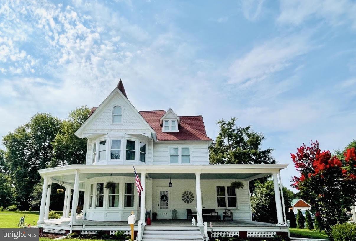 Welcome to one of Sudlersville's most extraordinary heritage homes, a magnificent Queen Anne Victorian that beautifully honors its historic character while embracing the comforts of modern living. Following an extensive 2019 renovation that left virtually no system untouched, this remarkable residence has been thoughtfully reimagined for today's lifestyle while preserving the timeless architectural details that make it truly one of a kind. Set on more than an acre beneath majestic centuries-old shade trees, this magical family estate commands attention with its soaring turret, five striking bay windows, and deep, sweeping wraparound porch that invites you to slow down and savor every season. Overlooking the neighborhood park, the setting is as enchanting as the home itself, nestled within the quintessential Hallmark town of Sudlersville, where the historic train station now serves as a museum and the soft rumble of the grain train passing through town a few times each week provides a nostalgic reminder of the community's rich heritage. Inside, soaring ceilings, exquisite millwork, and an impressive foyer introduce an unexpectedly open floor plan designed for both gracious entertaining and everyday living. The expansive kitchen is a true gathering place, featuring stunning custom cabinetry that extends to the ceiling with thoughtfully designed pull-out drawers, a dramatic designer backsplash, updated stainless steel appliances, many with transferable warranties, and a large picture window above the sink that fills the space with natural light. The kitchen flows seamlessly into the dining room, beautifully nestled within one of the home's signature bay windows. The adjoining family room creates an airy, connected living space rarely found in historic homes, while multiple rooms open directly onto the wraparound porch, blurring the line between indoor and outdoor living. A dedicated office surrounded by windows offers an inspiring workspace, and the butler's pantry with wet bar provides the perfect staging area for effortless entertaining on the porch and patios. The main-level primary suite offers exceptional convenience with a spacious ensuite bath featuring a soaking tub and separate shower, while a powder room completes the first floor. Upstairs, four additional bedrooms include a private ensuite guest suite and a beautifully appointed hall bath. Fresh new carpeting enhances the upper-level bedrooms, while two of the bedrooms are graced by the home's distinctive bay window bump-outs, creating expansive sitting areas bathed in natural light and showcasing the architectural character that makes this residence so special. A walk-up third floor offers abundant storage along with the enchanting turret room, an unforgettable space ready to become a library, reading retreat, artist's studio, or simply a breathtaking lookout over the surrounding landscape. The immaculate cellar provides exceptional storage, while the park-like grounds are designed for year-round enjoyment with patios, arbors, expansive lawns, a welcoming fire pit tucked beneath towering centuries-old shade trees, and two substantial outbuildings, including a garage and a detached studio currently used as a fitness space. Rich in history yet thoughtfully transformed for thoroughly modern living - including a Level 2 EV Tesla charger! This spectacular Queen Anne Victorian is far more than a home, it is a once-in-a-lifetime opportunity to become the next steward of one of Sudlersville's most treasured residences.