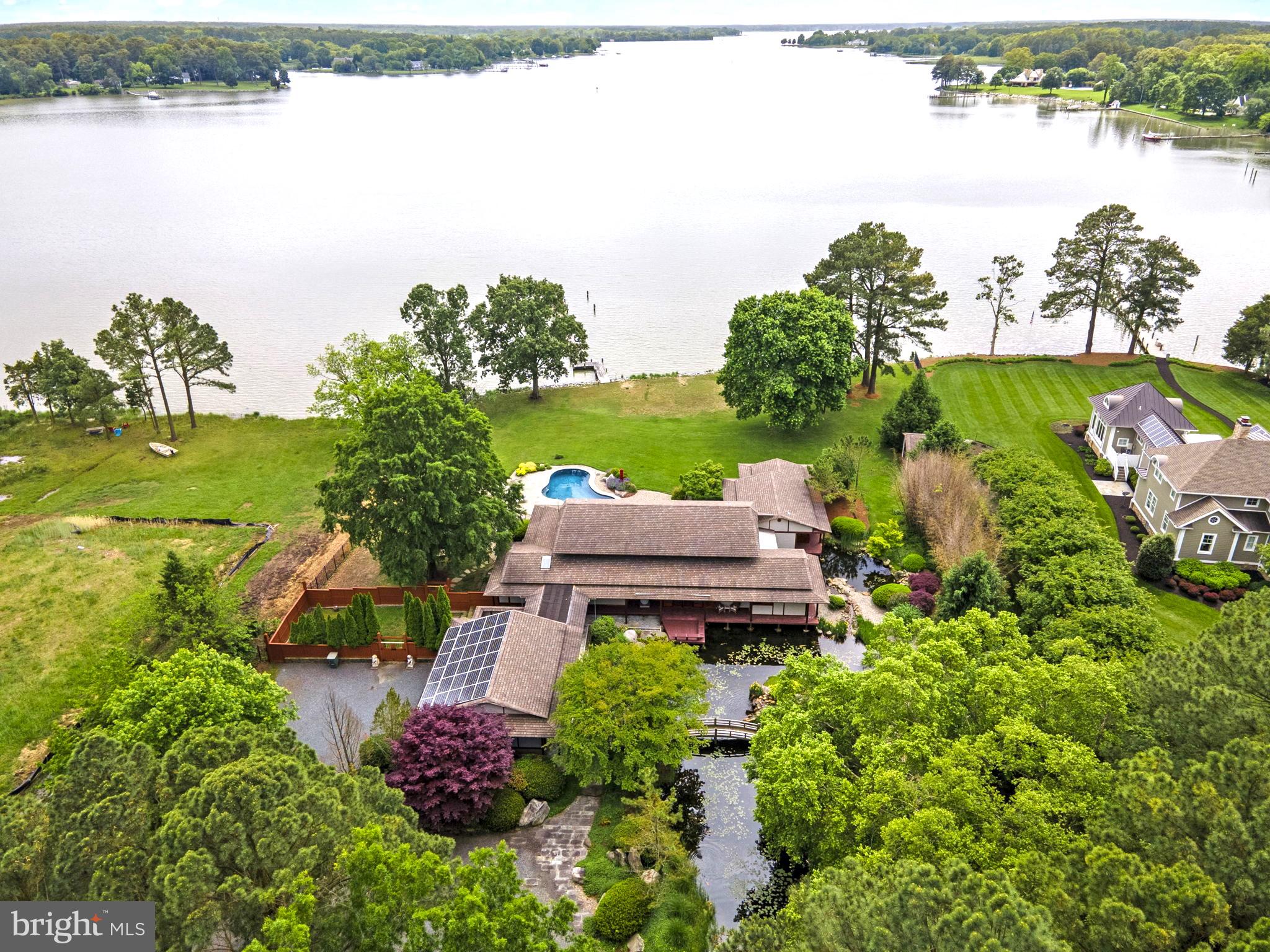 Welcome to this serene oasis nestled on the coveted Miles River, where tranquility meets luxury in this Japanese-inspired waterfront property. The meticulously crafted home has been curated to offer the ultimate in comfort, style, and refined elegance. The exterior of the home is a masterpiece of design, featuring lush gardens with native plants and flowers, trickling fountains, attractive foot bridges, and a Koi pond, creating a sense of peace, serenity, and privacy. A swimming pool, private pier with 3'+/- MLW, designated barbecue area, extensive patio, storage shed, and 2-car attached garage complete the exterior amenities. Inside, admire gleaming hardwood floors, custom cabinetry, and designer finishes throughout. The gourmet kitchen, featuring upgraded appliances, provides ample space for preparing culinary creations. Entertain guests in the luxurious living room, featuring a wet bar with wine storage, or enjoy a formal meal in the dining room, while enjoying views of the river, pool, and gorgeous grounds. The primary suite is conveniently located on the main level, offering a sumptuous ensuite bath with glass-enclosed shower and soaking tub, walk-in closet, and private waterside deck. Two additional bedrooms upstairs, each with their own private balcony and ensuite bath, and a bonus room, offer plenty of space for guests and storage.