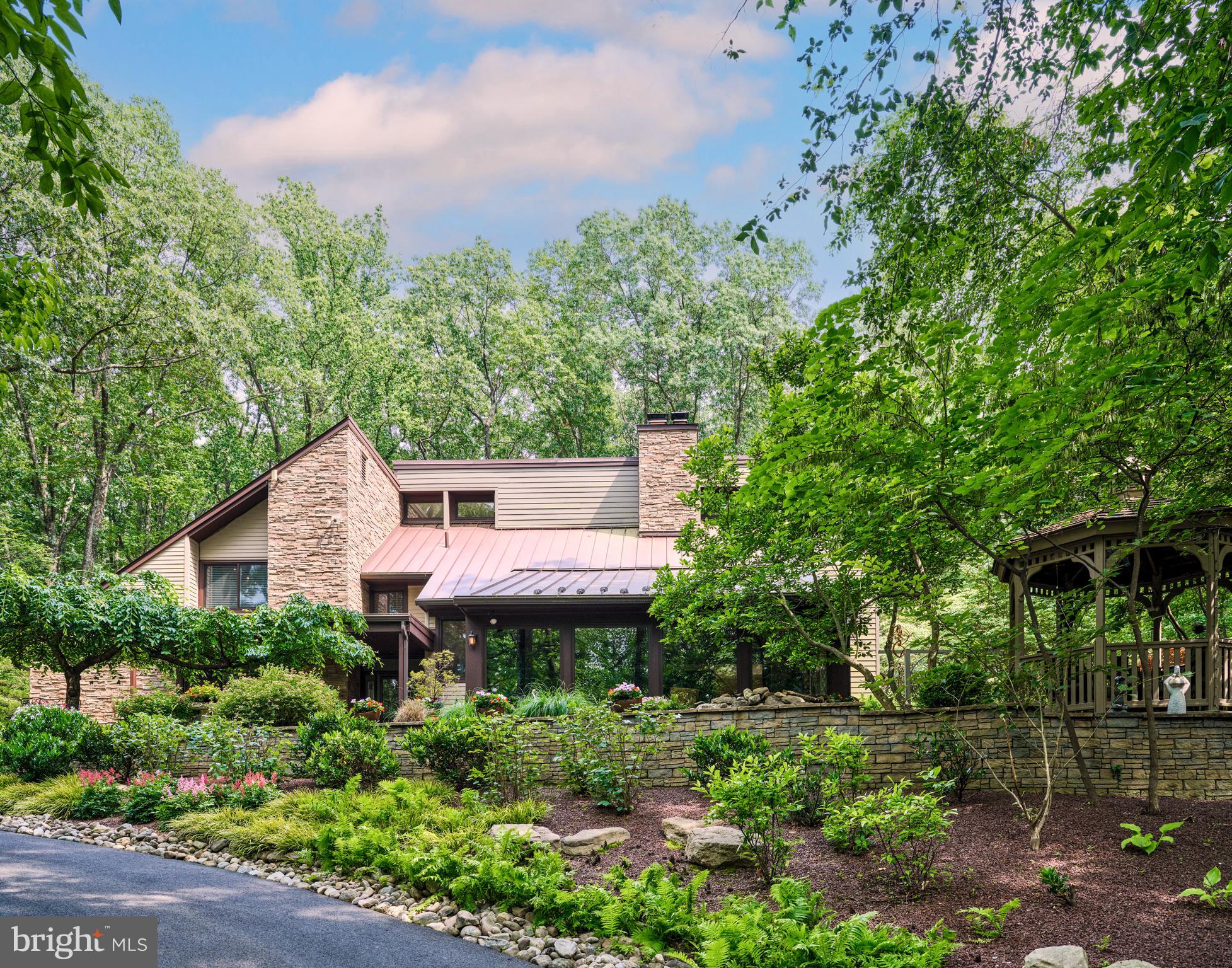 Embrace the joy of discovering "Paradise Found," a contemporary oasis nestled amidst nearly five private acres of enchantment, serenity, and natural splendor. A meandering driveway, bordered by stone terraces, mature gardens, meditation trails, and a richly populated koi pond, leads you to the hidden jewel of Ely Road in the charming town of New Hope, Pennsylvania.  As you step inside, the main floor offers a well-lit office space and an awe-inspiring two-story great room, featuring mirroring custom built book shelves that stretch from floor to ceiling. Adding a touch of rustic charm is a stone-finished wood-burning fireplace and a grand window display, allowing you to soak in the beauty of the gardens that encapsulate the property. The kitchen, both welcoming and functional, boasts a central island complete with a cooktop, a wall oven & warming drawer, a custom-made workstation, and a glass-walled sunroom offering stunning views of the pool haven. The journey upstairs brings you to the sumptuous primary suite, complete with a secluded deck off the bedroom, a luxurious bathroom w/ double vanity and glass shower, and a large walk-in closet with a private deck of its own. The second level also offers two additional, generously sized bedrooms, each adorned with skylights and equipped with their own bathrooms for ultimate convenience.  Adding to the exclusivity of the property is a custom-built wine cellar, showcasing an impressive wall of wine bottles and a full bar.  The backyard is a spectacle of its own with lush flowers and stone walls encircling the heated, saltwater pool with a cascading hot tub. Spend warm summer evenings around the outdoor fire pit, basking in the glow of an outdoor oasis illuminated by extensive landscape lighting. A freestanding garage, roomy enough for three cars, offers additional parking while providing a pristine work area for your tools and toys. This impeccably kept retreat is situated minutes away from the center of town, nestled within the prestigious New Hope-Solebury School District, and is strategically positioned nearby all primary commuter routes. If you've been on a quest for your next chapter, the one unique story that not only resonates with your head but also with your heart, then you have arrived at "Paradise Found". (Sellers are including ALL furniture and contents within home, both interior and exterior, with the sale.)