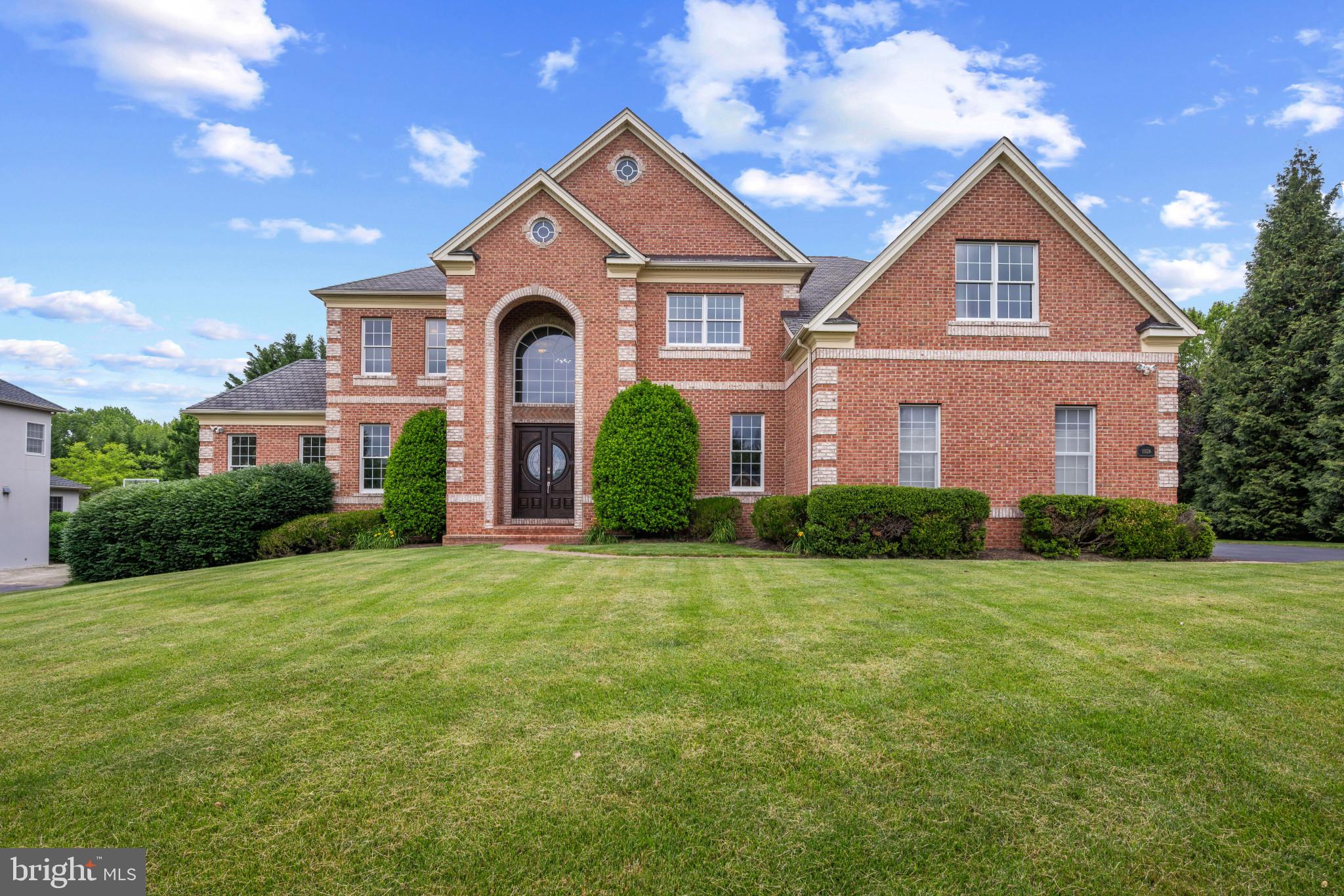 Stately all-brick Colonial residence, meticulously maintained by its original owner and showcasing exceptional craftsmanship, luxury finishes, and extensive custom millwork throughout. Offering 7,200 finished square feet, this impressive home features hardwood floors throughout the main level, a spacious driveway with ample parking, and thoughtfully designed living spaces ideal for both everyday living and grand-scale entertaining. // A dramatic two-story foyer with a sweeping curved staircase and statement chandelier creates a memorable first impression. French doors open to a distinguished study featuring floor-to-ceiling custom cherry built-in bookcases, while opposite the foyer, the formal living room flows seamlessly into the formal dining room, where elegant columns and a tray ceiling create a refined setting for entertaining. A versatile carpeted sitting room just off the living room provides additional space for relaxation or conversation. // Designed as the heart of the home, the open-concept great room offers an exceptional layout for entertaining and everyday living. The gourmet eat-in kitchen features granite countertops, a center island with breakfast bar seating and pendant lighting, a custom backsplash, abundant cabinetry, stainless steel appliances, a pantry, a writing station, and a sunlit breakfast room with the potential for future exterior access. Open to the kitchen is the impressive two-story family room, highlighted by a wood-burning fireplace, elegant columns, abundant natural light, a secondary staircase, and plush carpeting. // The luxurious owner's suite serves as a private retreat, featuring a tray ceiling, an extraordinary dual-sided walk-in closet with custom organization systems, and a spa-inspired ensuite bath complete with a frameless glass shower featuring dual showerheads, a dual-sink vanity, and a private water closet. The upper level also includes a dedicated laundry room and three generously sized secondary bedrooms with ample closet space. One bedroom enjoys a private attached bathroom, while two additional bedrooms share a dual-entry full bathroom. // The fully finished walk-up lower level expands the home's entertainment possibilities with a spacious recreation room, game area, and an impressive bar/kitchenette featuring granite countertops, a cooktop, dishwasher, and refrigerator. This level also includes a private movie theater, fitness room, versatile bonus room, full bathroom, and an unfinished storage room. Outside, beautifully maintained landscaping enhances both the expansive front yard and the large open backyard, which backs to mature trees for added privacy and a serene natural backdrop. // Additional highlights include a Generac® 20kW generator with quarterly maintenance, solar panels with a transferable electricity credit, solar panel cleaning completed in March 2026, two EV charging stations, septic system servicing completed in April 2026, chimney cleaning completed in April 2021, and interior and exterior pest treatment completed in March 2026, providing exceptional efficiency, convenience, and peace of mind.