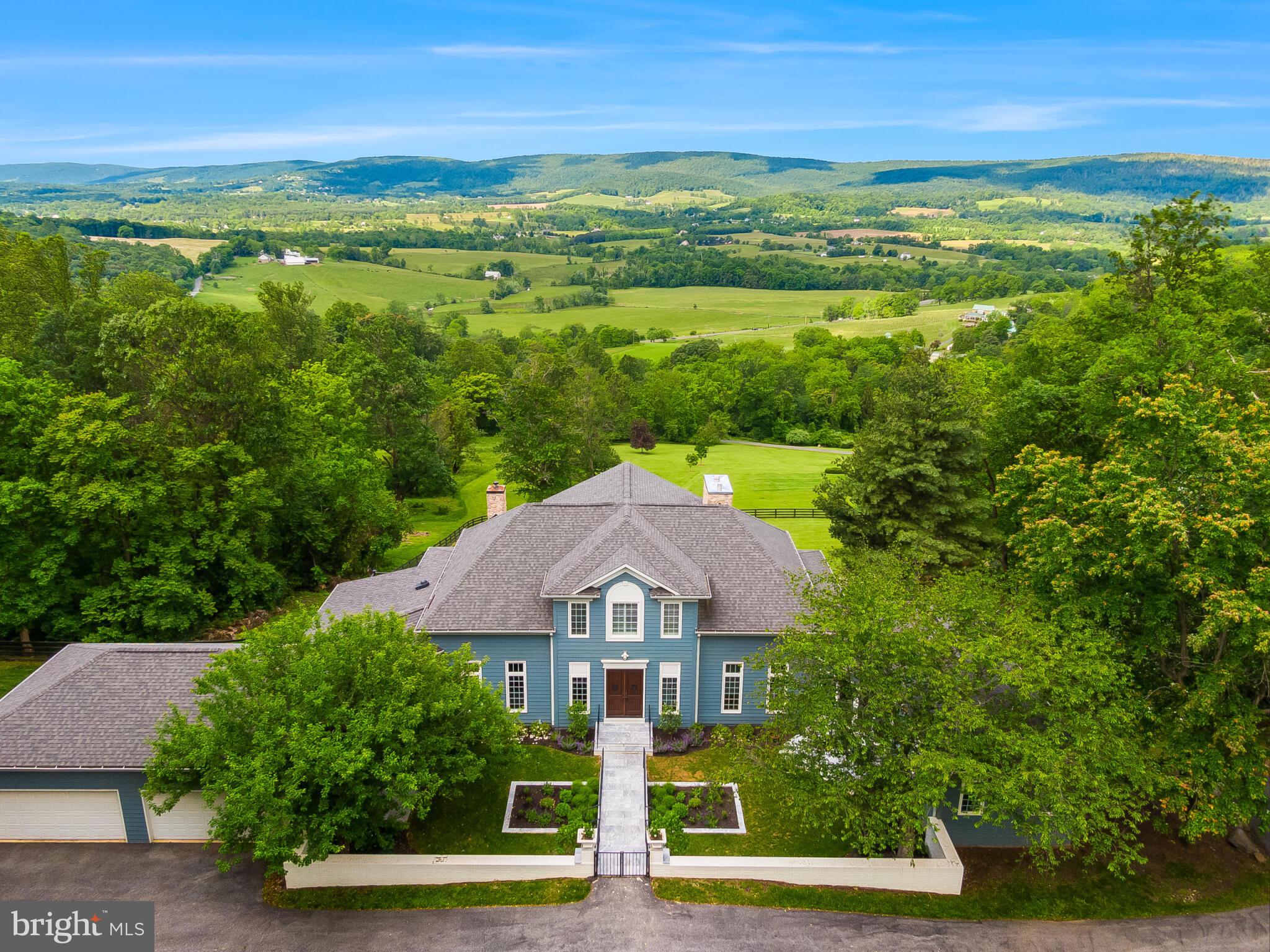 ENCHANTING FRENCH MANOR ESTATE: A LOUDOUN COUNTY TREASURE
Nestled among rolling vineyards and artisanal breweries, this extraordinary French Manor estate commands attention with its timeless elegance and unrivaled panoramic views. Set gracefully upon 10 pristine acres, the property captures the quintessential beauty of Loudoun County from every vantage point. Rising majestically above the gentle foothills of the Blue Ridge Mountains, just beyond the historic town of Hillsboro, this remarkable residence beckons with its stately presence and the awe-inspiring natural canvas that surrounds it.
Cross the threshold into a luminous sanctuary boasting 6,650+ square feet of meticulously crafted living space. The main level unfolds with warm hardwood floors that guide you through an inspired open floor plan, where living spaces flow together harmoniously while floor-to-ceiling windows frame the breathtaking landscape beyond. The heart of the home centers around a magnificent great room, where a custom fireplace creates an inviting focal point. Nearby, the gourmet kitchen stands ready to inspire culinary creativity with its professional Wolf range, bespoke cabinetry, and gleaming granite countertops. The adjacent breakfast nook offers a sunlit space for casual dining, while more formal gatherings find their perfect setting in the elegant dining room. 
The primary suite elevates luxury living to an art form, featuring a romantic fireplace, extensive custom cabinetry, and doors that open to a private terrace. Here, amidst the tranquility of nature, each morning begins with birdsong and endless views. The  renovated ensuite bathroom provides a spa-like retreat, two spacious walk-in closets, a sitting room, and a private deck serves as an extension of the living space—a perfect venue for morning meditation, afternoon conversations, or evening stargazing as the setting sun paints the mountains in amber and gold.
Ascend to the upper level to discover two generously proportioned bedroom suites, each boasting walk-in closets and private balconies that showcase the property's dramatic vistas. A comfortable loft area and full bathroom complete this level, creating an ideal retreat for visiting loved ones.
The walkout lower level represents a masterclass in versatile design, functioning seamlessly as either a sophisticated entertainment zone or a private guest apartment. This thoughtfully conceived space includes a spacious bedroom, full bathroom, recreation area, multi-purpose office, and a second kitchen. French doors reveal yet another private terrace, while cleverly designed storage solutions address practical considerations without compromising style.
The outdoor living experience is exquisite - the grounds unfold as a series of thoughtfully designed outdoor rooms: intimate patios for quiet reflection, a charming courtyard featuring a butterfly garden, secure fenced areas for beloved pets, and artfully positioned boulders throughout the expertly cleared landscape. Practical needs find their answer in the oversized four-car garage with custom storage systems and three picture-perfect outbuildings—including a delightful she-shed that offers a private retreat for creativity or relaxation.
The current stewards of this exceptional property have transformed both the structural integrity and aesthetic appeal of the residence, from reimagining the main level floor plan to adding luxurious details like automated light-filtering shades. Three state-of-the-art HVAC systems, a new septic field pump, and a high-capacity water heater ensure that the home's infrastructure matches its visual splendor.
Just beyond your private sanctuary lies the storied village of Hillsboro, a jewel of American history founded in the late 18th century and proudly listed on the National Register of Historic Places. This authentic enclave offers the perfect balance of historic charm and rural tranquility