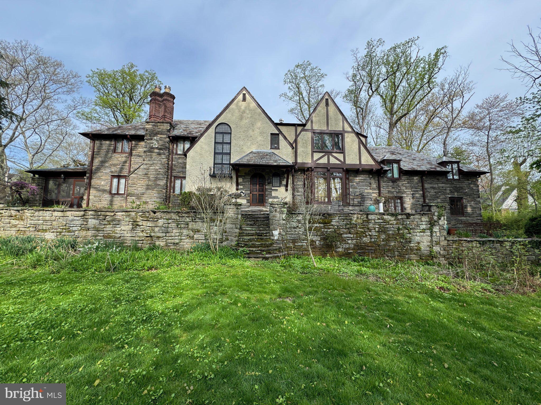 Classic Tudor home offered for sale for the first time in over 50 years. Custom built in 1927, this stunning stone and masonry mansion sits on a lush and private .57 acre corner parcel in the center of Wynnewood Valley. Outstanding classic details include all plaster walls and ceilings, custom mill work, built-ins, soaring leaded glass windows, exquisite brick estate style chimneys, grand curving main staircase, all wood doors, 2 fireplaces including custom Mercer Tile surround in living room. Updated kitchen with Sub Zero refrigerator, gas cooktop, door to back stairs and outside access to attached garage. Breakfast room with built-in bench seating and bright bay window. Cozy den off kitchen with built-in bookcases and storage and access to driveway. Formal dining room with wall of updated windows overlooking front patio and yard. Large living room with recessed lighting and Mercer tile fireplace surround and 2 doors to screened in porch. Enclosed entry vestibule with lower level access leads to two story foyer featuring a formal powder room & coat closet with doorways leading to living room, den and dining rooms; ideal for entertaining. Grand sweeping stairway to 2nd floor landing overlooking foyer below. Large primary bedroom suite with private bath and 2 closets. Three additional large bedrooms, a large office, small den, laundry room and hall bath complete second story. There is both walk-up and pull down stair access to ample attic space. Lower level has family room, great room with fireplace, wine cellar, powder room and large mechanical/storage area with direct access to rear of garage and stairs to covered breezeway between garage and rear driveway. Outside are several stone patios, stone lined driveway, wood bridge over small stream running alongside park-like grounds providing privacy and ample play space. This is a unique opportunity to own a one-of-a-kind classic Main Line Tudor estate in a coveted section of Lower Merion Township.