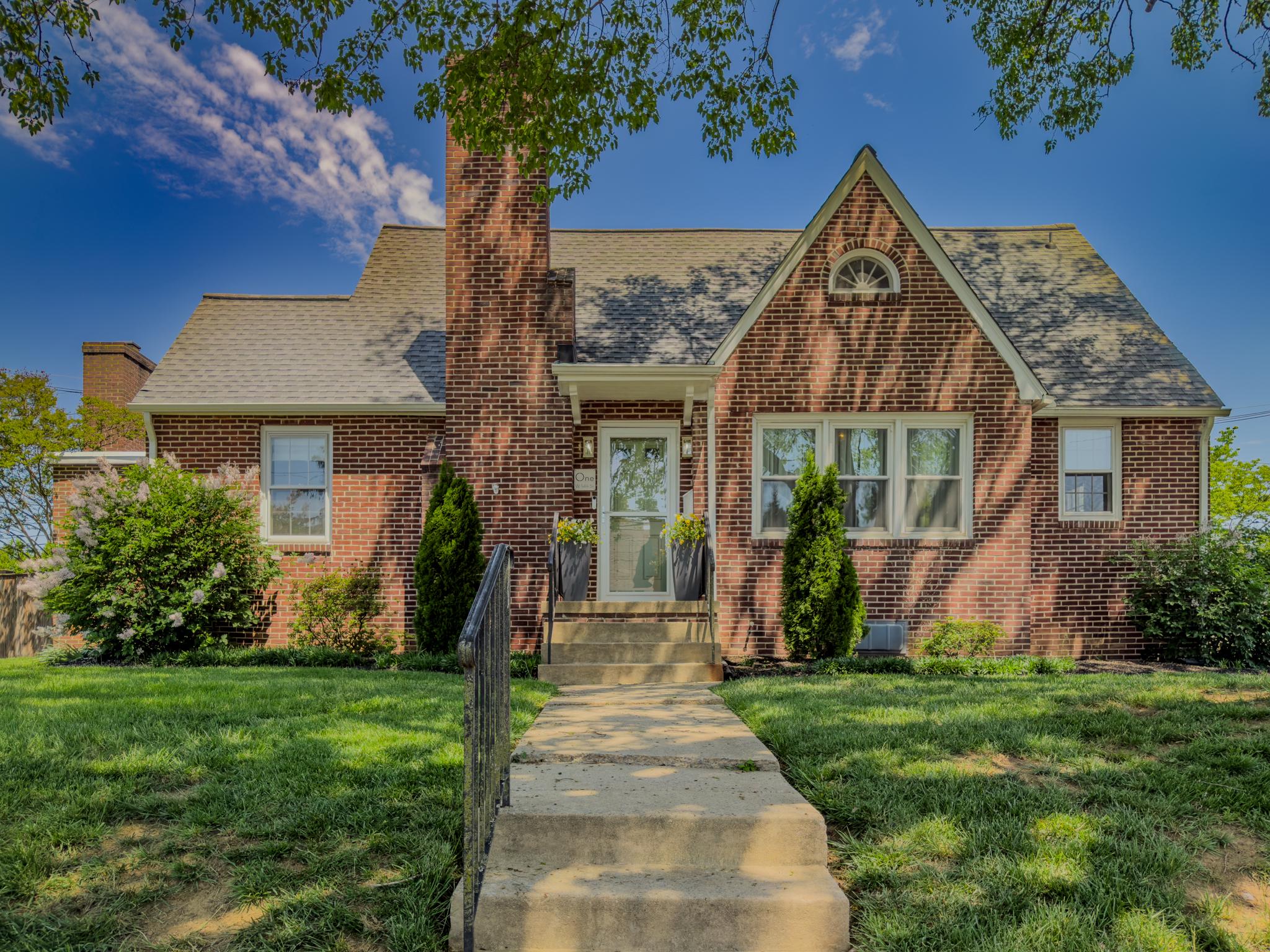 Welcome to 1 W 14th Street, a classic brick Cape Cod in The City of Frederick offering timeless character, thoughtful updates, generous outdoor space, and rare off-street parking. Set on a large lot with mature trees, established landscaping, fenced back yard, and large patio area, this home delivers the kind of indoor-outdoor lifestyle buyers hope to find near Downtown Frederick.

Inside, warm hardwood floors, arched openings, crown molding, and classic trim create an inviting first impression. The updated kitchen is the showpiece of the home, featuring a large center island, sleek light countertops, two-tone cabinetry, brass-toned fixtures and hardware, herringbone tile backsplash, statement pendant lighting, a built-in dining nook and coffee station, and a striking fireplace with dramatic stone surround.

The main level offers flexible living spaces, including a bright sitting room, a spacious family room with stone fireplace, a main-level primary bedroom, a separate office/mudroom with exterior access, and an updated full bath with a glass-enclosed walk-in shower, modern vanity, and designer finishes.

Upstairs, the home continues with additional bedrooms, a second full bathroom, hardwood floors, Cape Cod character, and a flexible landing/loft nook ideal for reading, studying, or relaxing. 

The lower level offers laundry, mechanical space, storage, and workshop potential. Outside, the fenced backyard is ready for relaxing, entertaining, gardening, pets, or play, with open lawn, privacy plantings, and a large patio area. The detached two-car garage sits on a separate parcel that is included with the sale, adding valuable off-street parking, storage, and workshop flexibility in Downtown Frederick.

Close to Downtown Frederick’s restaurants, shops, coffee spots, breweries, parks, arts, and local events, this home offers more than just a place to live. It offers a connection to the charm, convenience, and community that make Frederick such a special place to call home. Classic character, modern updates, generous outdoor space, and rare garage parking make this one worth seeing in person.
