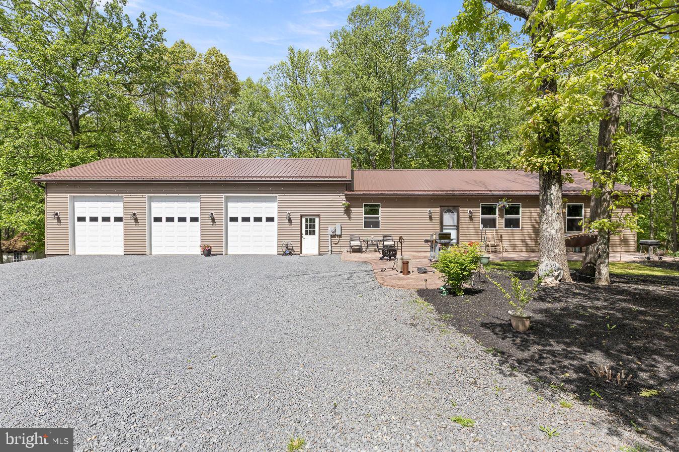 Custom-built and thoughtfully designed, this one-of-a-kind home on 5+ acres offers the perfect blend of craftsmanship, functionality, and peaceful country living tucked away in the rolling hills just outside Berkeley Springs. Built with durable 2x6 construction and heavy insulation, the home features extensive drainage around the poured foundation for long-term quality and care. Car enthusiasts, motorsports hobbyist and craftsman will love the impressive 1,500 sq ft attached garage/workshop complete with its own electrical box, multiple 220 outlets, water access, mini split system, and hydraulic lift hookup. Inside this truly warm and inviting home you will find solid wood doors, custom burnt trim throughout, luxury vinyl plank flooring and unique touches including two hidden bookshelf doors and an exquisite custom tiled shower in the primary bath. The spacious kitchen is centered around a stunning 8-foot island, perfect for entertaining and everyday living. The primary bedroom is on the main level, with 2 other bedrooms in the basement as well as a 4th room, great for an office/gym/hobby room. Outside, the property truly shines. Surrounded by natural beauty and open skies, the setting offers privacy, quiet, and the freedom to enjoy your hobbies without compromise. Enjoy the stamped concrete patios in the front and rear of the home, both with the footers already in place to add a covered porch and a deck, a RV hookup, and roofline outlets for hassle-free holiday lighting!  Walkout access from the garage, dining room and primary bedroom to your future deck adds convenience and connection to the outdoors. Located just minutes from Sleepy Creek Wildlife Management Area, you'll enjoy hiking, camping, fishing, swimming and boating. Whether you're looking for privacy and NO HOA, workshop space or a home designed with custom details throughout, this property is perfect as a primary residence, weekend retreat, or enthusiast getaway within easy reach of the DC and Northern Virginia metro areas. Schedule your showing today!