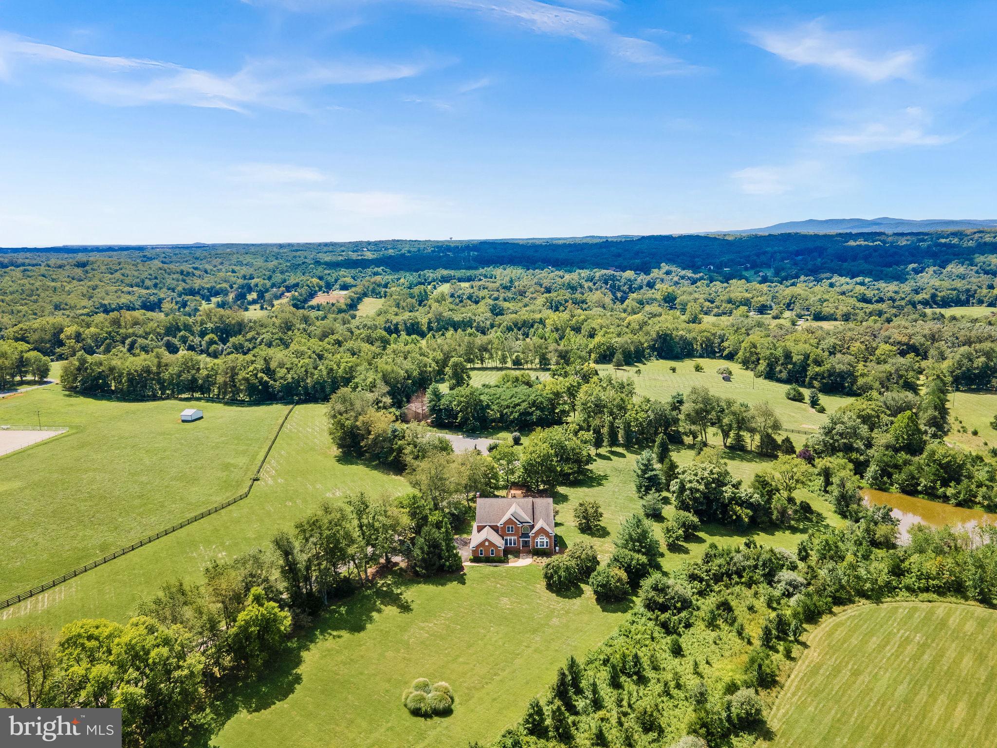 Searching for a haven that lets you wake up to panoramic views, serene seclusion, 50 acres to enjoy with Goose Creek frontage and a private pond?  Perched gracefully on a gentle knoll within the prestigious Red Cedar enclave of Conservancy properties, this timeless 6-bedroom, 5.5-bath brick estate delivers an urbane lifestyle with a rare blend of luxurious design and rural freedom, just minutes from downtown Leesburg and the Brambleton Town Center!

Enter a grand foyer where soaring ceilings and a striking staircase set a tone of sophistication. On either side, find a formal living room and an elegant dining alcove ready for memorable gatherings. Throughout the home, gleaming wood-flooring, tasteful millwork, wrought iron accents, bright windows, and a calming neutral palette (freshly painted) create a sense of classic refinement warmed by natural light.


Stylish and impressive, the gourmet-inspired kitchen has been outfitted with stainless steel appliances, plentiful cabinetry, luminous granite countertops, and a central island that encourages culinary creativity. Adjacent is a sunroom that can double as a large breakfast nook, with walls of windows offering those enviable morning moments. The nearby family room invites relaxation with its mellow brick hearth and sprawling backyard views, while a separate office or main level bedroom, offers privacy for remote work or overnight guests.

Upstairs, your stunning primary suite feels like the ultimate refuge, with an oversized walk-in closet and a luxurious ensuite with a frameless shower and separate soaking tub. Three additional retreats, including a Jack-and-Jill layout, offer comfortable repose for visitors or an oasis for practicing hobbies. The finished basement is a versatile sanctuary, featuring a kitchenette and bar, gaming corner, den with a fireplace, a guest bedroom with a full bath, and abundant storage.   


For the equestrian or outdoor enthusiast, the estate’s amenities are unrivaled. A traditional center aisle barn features six stalls (including wash and dry stalls), a tack room, hay loft, and adjacent paddocks. Ride year-round in the fenced, bluestone dressage ring (80 x 128) or explore the peaceful grounds with its private trails, Goose Creek frontage, and private pond. Three additional run-ins with water and a workshop with oversized bays, a flexible office, and an RV pad enhance the property’s functionality.

Beyond the lifestyle it offers, this home combines natural beauty with modern practicality, featuring public utilities, a laundry room, and an attached 3-car garage as well as New HVAC and Hot Water Heater. Located just a short drive from Dulles Airport, Brambleton, and Arlington, this one-of-a-kind residence is more than a refuge—it’s a destination. Come see how life expands when in a place where you can grow anything from your garden to your goals!