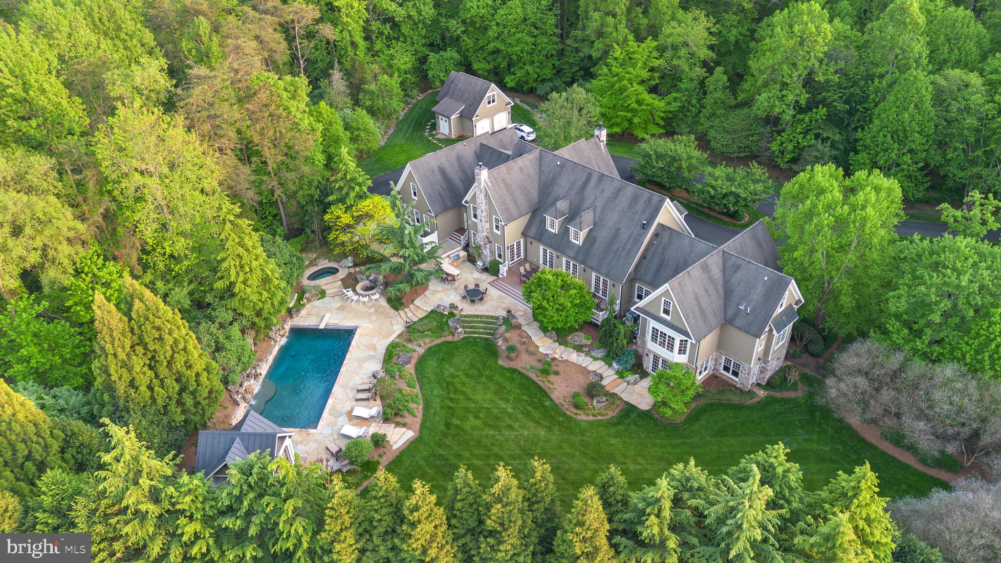 Welcome to this stunning custom-built estate on 5 tree-lined acres—an entertainer’s dream with a backyard paradise that feels like a private resort. Featuring a 22’ x 44’ rectangular pool, stone patios, a pavilion for covered lounging, and multiple spaces for outdoor dining and entertaining, this home offers unmatched indoor-outdoor living surrounded by mature landscaping and total privacy.

A long driveway winds through the wooded setting and leads to a grand circular drive. The exterior blends timeless charm with stone and cedar siding, setting the tone for what’s inside.

Step into a bright two-story foyer with coffered ceilings, chair rail, picture frame wainscoting, and elegant wood-trim accent walls. Adjacent is a formal sitting room with a stone gas fireplace and backyard views. Next to it, a double-story office finished entirely in oak offers a stunning library-like retreat with floor-to-ceiling wood, built-in shelving, and a staircase leading to a unique bonus room—ideal as a creative entertainment space or another bedroom.

The kitchen is the heart of the home, adjacent to the living area and separated by a striking arched opening. On the other side is a sunroom with a gas fireplace and French doors that open to the rear deck. Both the kitchen and sunroom overlook the backyard’s lush trees and pool. The kitchen features custom Brookhaven cabinetry, a Wolf 6-burner gas range with pot filler, Sub-Zero 36” paneled fridge, double wall ovens, and a walk-in pantry with Wood-Mode built-ins, a Sub-Zero wine fridge, and second dishwasher.

The main-level primary suite is a peaceful retreat with a large bay window overlooking the pool, two walk-in closets with wood built-ins, and a spacious bath—bright, airy, and private.

Upstairs offers five additional bedrooms, a loft area, and a bonus room with an office—ideal for guests, hobbies, or extended family.

The walkout lower level has two staircases and endless possibilities: an entertainer’s bar with dishwasher, mini fridge, and appliances; a climate-controlled wine cellar with built-in cubbies; and a theater room with surround sound and multi-level seating. A spacious bedroom with en suite bath overlooks the pool—perfect for guests.

The backyard is a showstopper. The large pool features two stone waterfall elements and a built-in ledge for in-water seating beneath the cascades. Nearby are a stone-surround jacuzzi, a fire pit area, and an outdoor kitchen with a stone exterior, built-in bar seating, and grill. A vaulted-ceiling pavilion with a stone feature wall and multiple patio areas complete the resort feel.

For car enthusiasts, the property includes seven garage spaces: an attached four-car garage with floor-to-ceiling built-ins, and a separate three-car detached garage with a finished upper-level workshop.

Located just 5 miles from Great Falls Village and minutes from Route 7, the Dulles Toll Road, Tysons, and D.C., this home offers both privacy and convenience. Zoned for the award-winning Langley High School pyramid.