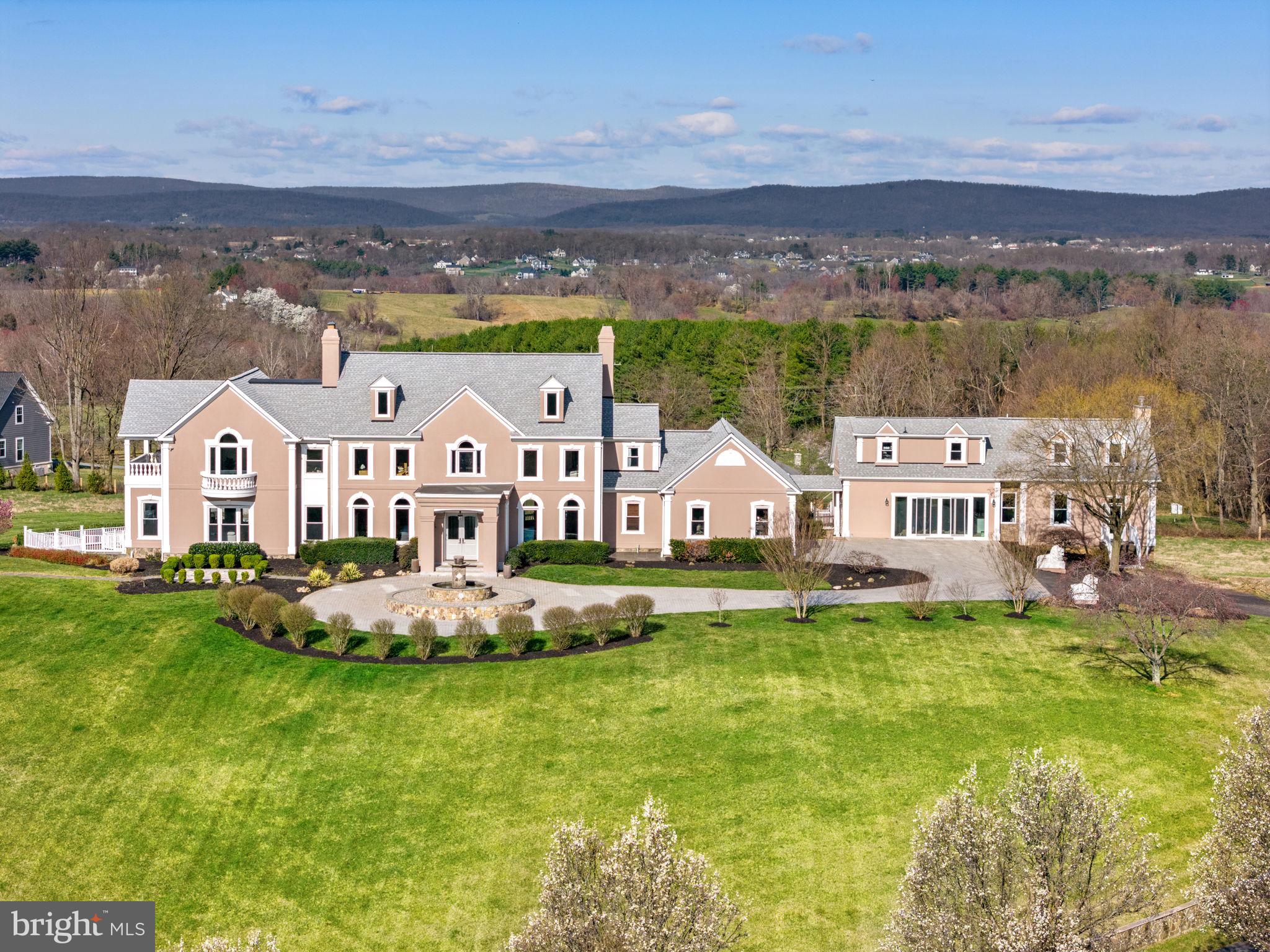 Step into ultimate luxury and comfort in this magnificent Beacon Hill Estate! A private drive surrounded by beautiful rolling hills and stunning mountain views,  leads you to the front of this home, where you are greeted by a tranquil fountain.  The light-filled, double door entryway welcomes you inside, leading into the 3 story foyer with grand wood staircase. Anchored by gorgeous fireplaces, ornate columns, exquisite lighting and stunning windows, the main level provides the perfect backdrop for lavish dinner parties and gatherings. The Chef-inspired kitchen is the true heart of the home, with  two-tone cabinetry accented by marble countertops and backsplash. Top of the line Wolfe and Sub Zero appliances make entertaining a breeze. Two islands provide additional storage and seating, as does the adjacent wet bar. 
The second level primary suite is a relaxing oasis, with a spacious sitting area that leads you into one of the two primary bathrooms, and two of the walk-in-closets, equipped with custom cabinetry. The primary bedroom is accented by a gorgeous fireplace, a private balcony and one additional walk-in-closet. Both primary bathrooms offer free-standing tubs and walk-in showers, both with stunning Moroccan-style tilework. Two additional bedrooms with attached en-suite bathrooms complete the second floor. The 3rd floor consists of two more bedrooms with en-suite bathrooms, providing lots of privacy for guests. 
The basement is where the less formal rooms reside, with several spaces that can be used to your liking. With health and wellness in mind, there is a full gym and a full bathroom with a sauna. Entertainment awaits you in the fully equipped theater room!
A fully finished guesthouse provides additional privacy for family and friends, with its own kitchen, bedroom, 2 full bathrooms and other flex space. 
With its several balconies and decks, there are many outdoor options to enjoy the stunning sunsets. Go for a dip in the inground pool and enjoy your private, lit tennis court as well. 
This stunning home is the perfect combination of 30+ private acres, yet 10 minutes from Leesburg, a close drive to Dulles Airport, Reston, Tyson’s Corner and DC! Many outdoor activities nearby for the nature lovers, as well as an abundance of dining and shopping options, wineries, and much more!