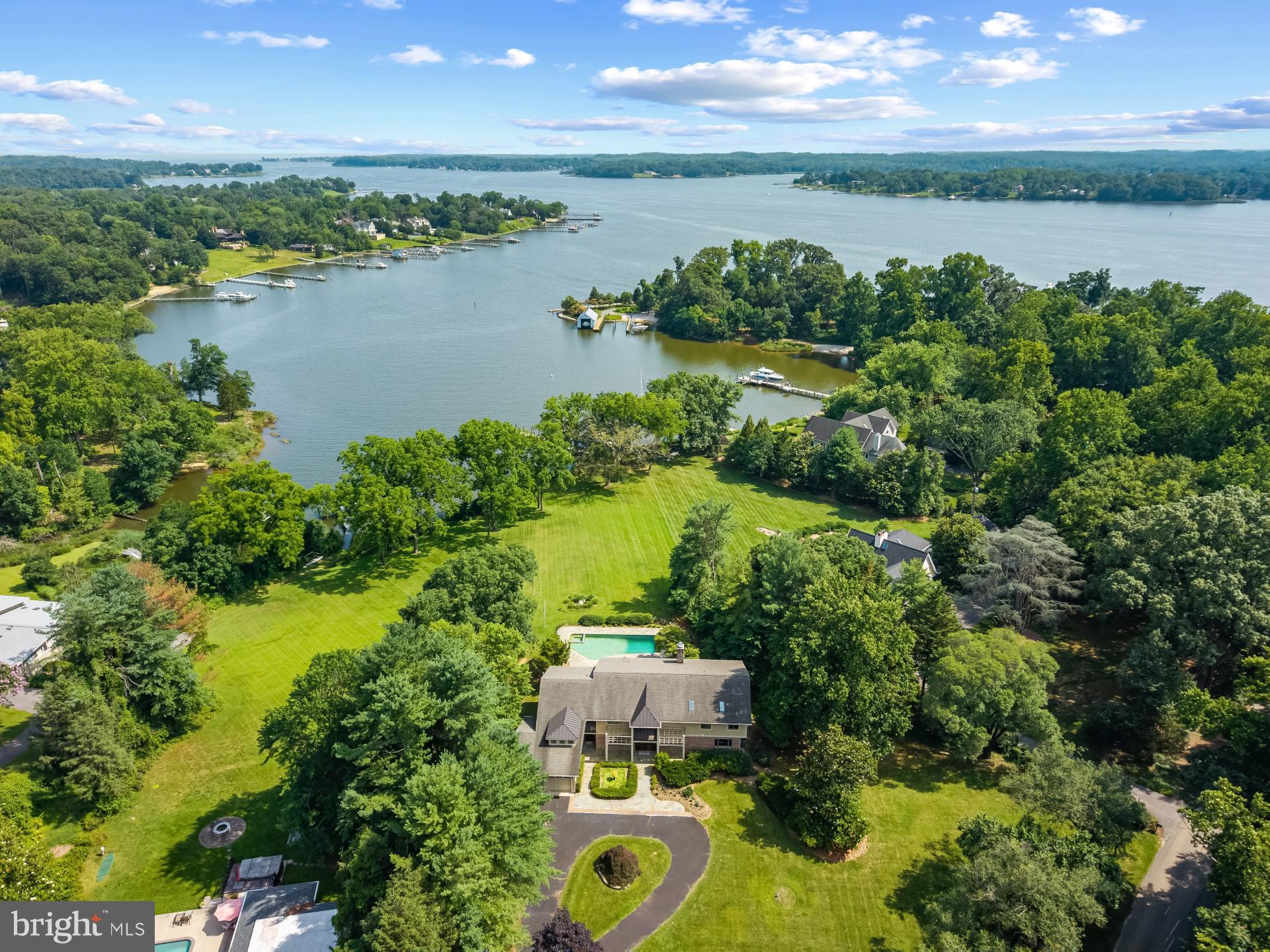 This stunning waterfront retreat offers privacy, breathtaking views of Crab Creek and the South River, and a waterside pool. The newly extended pier can accommodate a 50' sailboat. South-facing exposure and walls of windows let in tons of natural light and the sunlight sparkles off the serene waters at the shoreline. The beautiful renovation by Gate One Builders and new hardwood flooring created an open-concept main level featuring floor-to-ceiling windows that showcase the water. Relax by the pool, or visit the private pier with a covered slip and 6-foot water depth—perfect for boating to the Chesapeake Bay. Inside, the sun-filled living room boasts a stacked stone fireplace and beautiful hardwood floors, seamlessly connecting to the dining area and patio. The gourmet kitchen features Caeserstone waterfall countertops, a Wolf 6-burner range, Sub-Zero refrigerator, custom cabinetry, and a spacious island with a prep sink. The main level also includes a second primary suite, allowing for multi-generational living or aging in place. An office overlooking the garden provides a peaceful workspace. Upstairs, the primary suite offers a private waterside deck, a wet bar, and a luxurious spa bath with freestanding tub and oversized shower. Two additional water-view bedrooms each have their own bathrooms, and the oversized catwalk overlooking the living room makes a great office or reading nook. The lower level includes a game room that opens to the pool, a fifth bedroom, a sixth bathroom, and ample storage space.  Envision yourself enjoying the Annapolis waterfront lifestyle every day! Located just minutes from downtown Annapolis and quick access to commuter roads traveling to D.C., Baltimore, Eastern Shore and beyond. Welcome Home!