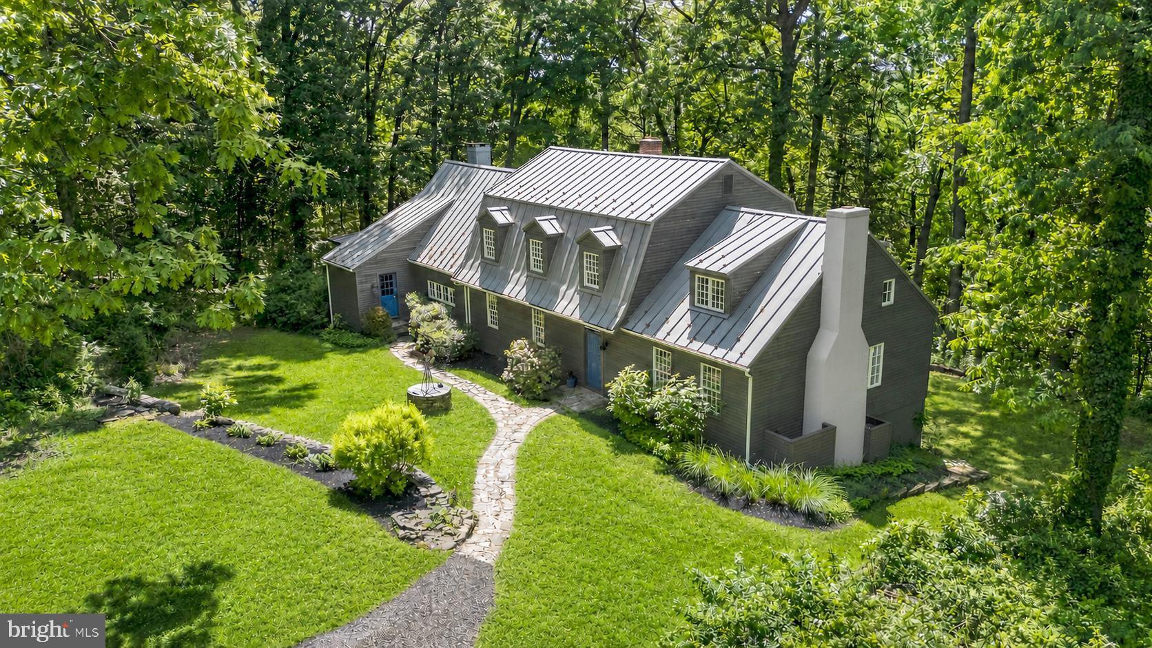 Nestled at the end of a completely private driveway on a breathtaking 5-acre parcel in desirable West Vincent Township, this stately farmhouse offers a rare blend of seclusion, character, and convenience within the Owen J. Roberts School District. Surrounded by rolling meadows and mature trees, the setting feels like a private retreat while remaining just minutes from Marsh Creek State Park, French Creek trails, charming local restaurants, farm markets, and the vibrant villages of Chester Springs and Birchrunville.  TA newer metal roof crowns the home, adding both timeless appeal and durability.
Step inside the spacious foyer and immediately appreciate the extraordinary mission-style wainscoting crafted from reclaimed wood salvaged from a historic Philadelphia bar.  No expense was spared with beautiful wide plank hardwood floors throughout.  The sun-drenched living room welcomes you with a hotel lobby size and vibe, including a stunning central fireplace and abundant natural light. Across the rear of the home, a cozy office with a wood-burning stove creates the perfect workspace with peaceful views and warm ambiance. The office flows seamlessly into the dining room, where newer French doors open onto the expansive rear deck. The country kitchen overlooks a generously sized great room featuring another fireplace, walls of windows, and direct access to the deck, all framed by tranquil wooded views.
Upstairs, the thoughtfully designed primary suite features a unique split bath layout for privacy and comfort. One side includes a private room with a gorgeous brand new walk-in shower, sink, toilet, and closet, while the opposite side offers a soaking tub, separate sink, and an oversized walk-in closet. This primary suite hallway is also home to another large walk-in closet/room that could be a nursery or full laundry room.   Two additional bedrooms, hall walk-inn closet and another full bath complete the upper level. Stretching across the back of the home, the sun-dappled deck is partially shaded by a lush, plant-covered pergola, creating an idyllic setting for entertaining or quiet relaxation. The walk-out basement  with radon remediation system remains unfinished and ready for your vision, offering endless possibilities for additional living space, recreation, or storage.   A standout feature of the property is the impressive detached garage added in 2014, showcasing beautiful natural wood finishes and exceptional craftsmanship throughout. Designed with both functionality and style in mind, the extra-long and extra-wide two-car garage offers ample space and ceiling height to comfortably accommodate two full-size trucks. In addition, a separate equipment garage with its own automatic garage door provides the perfect space for tools, lawn equipment, recreational vehicles, or workshop needs. Stairs lead to a spacious second-level storage area complete with windows, creating a bright and versatile space ideal for storage, hobbies, or future customization.  Property is in  French & Pickering Creeks Conservation Trust which will allow the construction of one barn.  Generator is fueled by a leased propane tank (Styer Propane).  GPS  is using Spring City rather than Chester Springs, legal address is Chester Springs.