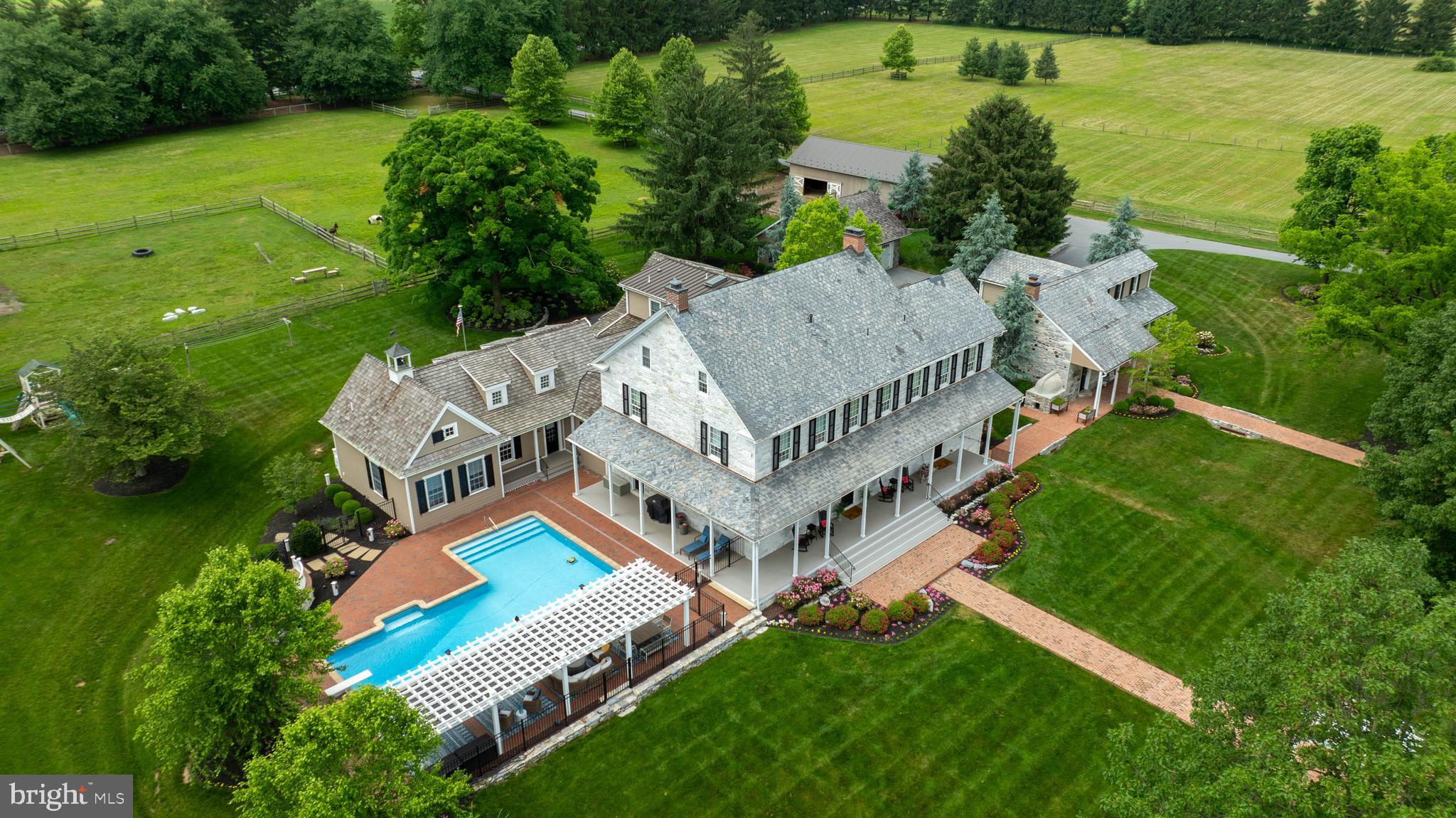 Welcome to High Cross Farm! Step back in time to a historic farm settled over 200 years ago. Two dwellings plus in-law suite, a bank barn, a pole barn, a horse barn and pastures sit on nearly 51 acres of beautiful farmland in the heart of Lancaster County. The stone farmhouse, built in 1819, has been lovingly renovated with the highest quality materials and workmanship, keeping true to period details. Original pine wood floors, graceful arches, a grand staircase, fireplaces, and vintage hardware and doors bring your senses to an era of long ago. The addition to the original home was constructed with reclaimed barn wood and stone, keeping with the time period to seamlessly blend old and new. A custom kitchen by Colonial Craft Kitchens soars with reclaimed beams in a peaked 2 1/2 story ceiling. The custom island is built from reclaimed barn wood with custom light fixtures designed specially for this space. Granite countertops, a farmhouse sink, high-end appliances, a coffee bar, and a butler’s pantry make this kitchen a cook’s dream. Three sitting areas, from casual to formal, invite family and friends to gather together for all occasions. The formal living room takes your breath away with white summer beams, a marble fireplace and built-in corner cupboard. The dining room offers another original corner cupboard and the perfect space for meals with family and friends. Upstairs, the luxurious primary bedroom and bathroom create a private haven with reclaimed wood beams in a lofty ceiling, a clawfoot soaking tub, and a designer glass shower. There are four more bedrooms and two full bathrooms, plus a second laundry on this floor. On the third floor is a spacious double bedroom and a special display of the original beam the builders used in construction. The farmhouse basement provides a movie room, personal exercise room, and a domed wine cellar. Outside, wander along the magnificent front porch to the pool and cool off in the crystal water or lounge under the pergola. Adjoining the farmhouse is a full in-law suite with a separate entrance. The home features one-floor living with an open plan kitchen and living room, and a vaulted ceiling with wood beams. There is a primary bedroom and bathroom with a handicap-equipped shower, laundry area, a walk-in closet, and an office or storage space. This bright and cheery home offers private accommodations for extended family or guests, yet is conveniently connected to the main farmhouse. The separate stone guest house was built in 1790. It has been fully renovated with four bedrooms, two full bathrooms, and a laundry. The living room, part of the original structure, includes a heated brick floor and restoration of the original hearth and beehive oven. A fully renovated bank barn provides stunning private event space. The upper level gleams with wood floors and crisscrossing beams, and is also equipped with powder rooms. The lower level houses seating for guests, a warm fireplace, and a fully-equipped kitchen. Outside is a large, brick patio for continued entertainment. The pole barn is divided into a garage, with room for RV and boat parking, and a climate-controlled workspace with an office, reception area, and powder room. The horse stable includes two horse stalls and a wash stall, and opens to fenced-in pasture. Walking trails invite you to meander to the pond with a flowing fountain, or sit around the firepit, or say hello to the animals. This picturesque, historical farm in the heart of Lancaster County blends expansive luxury living with idyllic country life.