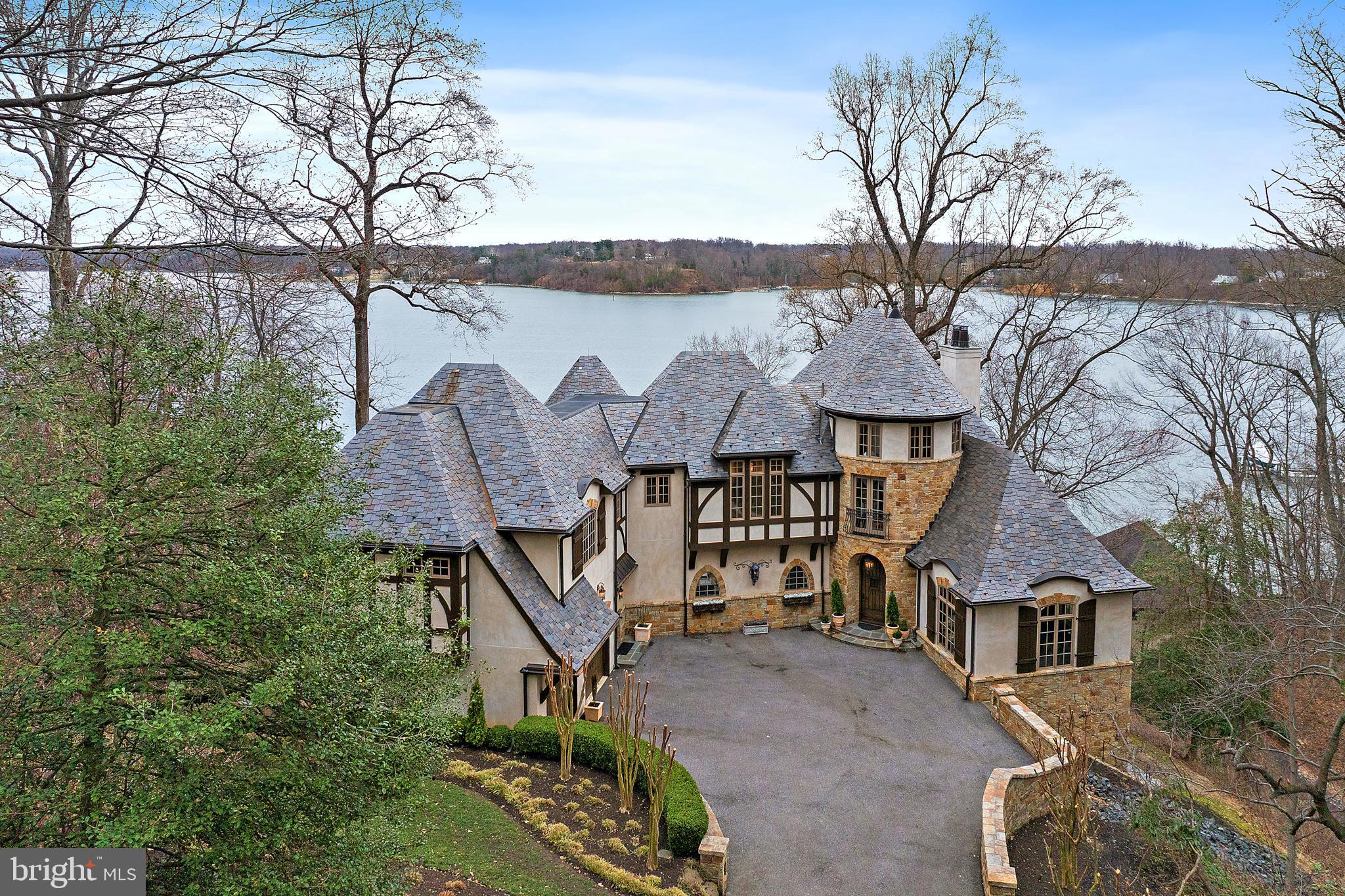Set on 4.5 picturesque acres along the Severn River, this exceptional Tudor–French Country estate designed by Scarlett Breeding of ABS blends timeless architecture with refined craftsmanship just minutes from downtown Annapolis. Panoramic river views define the property, complemented by a detached two-car garage with private guest quarters featuring a kitchenette and full bath. Outdoor living is equally compelling, with a fire pit, boathouse for convenient dockside storage, and a private pier equipped with a 20,000 lb boat lift—ideal for embracing true waterfront living. Access the dock via a scenic path and stairs or by private tram. Inside, light-filled interiors capture sweeping water views and flow effortlessly through a thoughtfully designed floor plan suited for both everyday living and elegant entertaining. A dramatic curved staircase anchors the foyer, leading to a main level that includes a gourmet kitchen, living room with a gas fireplace, bar, office, mudroom, two powder rooms, and a formal dining room. The chef’s kitchen is outfitted with a 6+ burner Wolf range, hammered copper sinks, dual dishwashers, expansive prep space, and a generous pantry. The living area opens to a spacious deck, perfect for waterfront gatherings. Upstairs, the primary suite offers a private retreat with its own balcony, wet bar, two walk-in closets, dual vanities, and a walk-in shower. This level also includes flexible bonus space, two additional bedrooms, a full bath, and a laundry room. The lower level expands the living space with two additional bedrooms, two full baths, a family room with fireplace and bar, and a game room—all with easy outdoor access and continued river views. All levels of this home can be accessed by an elevator.  Some of the well executed details in this home include wooden beams, arched doorways, curved walls, extensive stone work, intricate iron work, dramatic light fixtures, walnut flooring,  dramatic built-ins and the highest level of craftsmanship and execution.  A rare opportunity to own a meticulously crafted waterfront retreat, with over 6500 sq. feet of finished space, that seamlessly combines old-world charm with modern luxury.