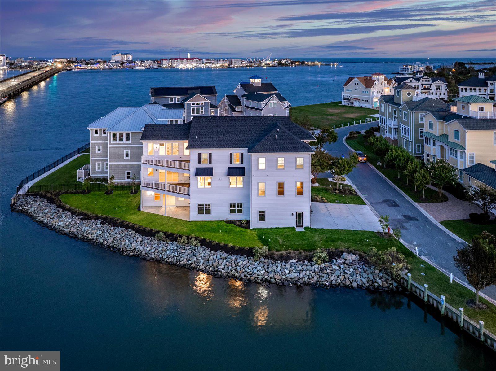 Stunning custom 5BR/5BA estate is located in the prestigious Estates at Inlet Isle Lane in West Ocean City.  This custom home showcases exceptional craftsmanship, a unique architectural style, and an unbeatable waterfront location. With panoramic views of the marina, bay, canal and ocean, this property offers the perfect setting to enjoy endless sunrises and sunsets. Boating enthusiasts will appreciate the deep-water slip that accommodates up to a 42-foot boat, providing easy access to the ocean through the inlet. The home’s exterior is sleek and modern, featuring clean white lines, stone finishes, and striking black accents that complement its coastal setting. Upon entering the first floor, you’ll find a spacious recreation room and a full bathroom—ideal for entertaining guests or relaxing after a day on the water. An elevator or staircase leads to the second level, where a gourmet kitchen awaits. This chef’s kitchen includes high-end appliances, quartz countertops, a custom coffee bar, and ample cabinetry, all set against a backdrop of wall-to-wall windows offering breathtaking water views. The adjacent family room features soaring ceilings, a dramatic floor-to-ceiling stone fireplace, and cedar wood accents that draw your eye to the expansive windows overlooking the bay. This open and airy space is perfect for entertaining family and friends. Also on this level is a luxurious primary suite complete with a large walk-in closet with custom shelving, a spacious custom shower, and a beautiful soaking tub. A second bedroom and bathroom are also located on this floor. The third level offers even more space to relax and unwind with a second family room/lounge area featuring another coffee bar and panoramic water views. This floor includes a second primary suite with its own spa-like bathroom, plus two additional bedrooms that overlook the marina.
Multiple decks on every level allow you to enjoy the fresh air and cool summer breezes from sunrise to sunset. The oversized garage provides plenty of space for large SUVs and all your beach gear, with potential to finish part of the space if needed. Located close to world-class marinas, golf courses, Assateague Island, the Ocean City Boardwalk, and some of the area’s best restaurants, this home offers the perfect blend of luxury, comfort, and coastal living. It’s a place where you and your loved ones can create memories that will last a lifetime.