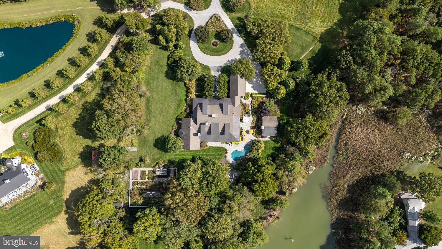 Set along the peaceful waters of Caulk Cove, this extraordinary waterfront estate offers luxury, privacy and natural beauty across more than 10 acres. The property features open farm fields and professionally landscaped, park-like grounds, with a tree-lined driveway creating a breathtaking approach to the residence. Built in 2013, the custom-designed home encompasses nearly 8,500 square feet of thoughtfully curated living space, positioned to capture sweeping waterfront views. A gracious front porch welcomes you into a grand foyer, setting the tone for the exceptional craftsmanship found throughout. The main level offers soaring 12-foot ceilings, rich hardwood floors, expansive windows and doors and custom millwork including crown molding, coffered and tray ceilings and elegant board-and-batten detailing. At the heart of the home, the living room serves as a remarkable gathering space with a dramatic floor-to-ceiling stone fireplace, custom built-ins, coffered ceilings, a wet bar and access to the rear porch. The kitchen is a stunning focal point, featuring a diamond coffered ceiling, custom handmade walnut cabinetry, two oversized islands, white and leathered granite countertops, and a Wolf six-burner, dual-oven range. A fully equipped butler’s pantry offers extensive cabinetry, generous counter space, a secondary refrigerator, dual dishwashers, a wine refrigerator and an electric oven. The open dining area flows seamlessly between the kitchen and living room. The primary suite is a private retreat with a tray ceiling, wood-burning fireplace, expansive walk-in closet with custom built-ins and vanity and a luxurious bath featuring heated floors, a jetted soaking tub, separate vanities, an open tile-and-glass shower and a private water closet. The suite is completed by a private sitting room with fireplace and wet bar, along with a private screened porch overlooking the gardens and serene waterfront. Four additional ensuite bedrooms each offer unique and luxurious bath designs. A well-appointed laundry room with ample cabinetry and generous counter space enhances everyday convenience and leads directly to a functional mudroom with access to the attached two-car garage. The second level features 9-foot ceilings and is anchored by a spacious family room with a stone hearth wood-burning fireplace and built-in window seating, flowing into a billiards area with wet bar, creating an ideal space for entertaining. The sixth bedroom currently includes custom built-in bunk beds but was originally designed as a home office and offers flexibility to be restored to its original use. The home’s exceptional design extends seamlessly outdoors, with a spacious screened porch leading to an open-air porch with a wood-burning fireplace and outdoor entertainment setup. Bluestone walkways and patios lead to a 20’ x 40’ lagoon-style Gunite pool with a waterfall feature, an outdoor kitchen and a waterside fire pit offering stunning sunset views over the cove. The property also includes a charming one-bedroom guest house with a luxury kitchen, open living area with fireplace and screened porch. A private dock with approximately 6’ MLW offers two boat slips, a floating dock and access to waterfront dining and premier fishing throughout the Chesapeake Bay and surrounding tributaries. Additional highlights to the home include a greenhouse with raised garden beds, a fenced garden area, professional landscaping with accent lighting, and a full irrigation system.  This exceptional estate is truly one-of-a-kind!