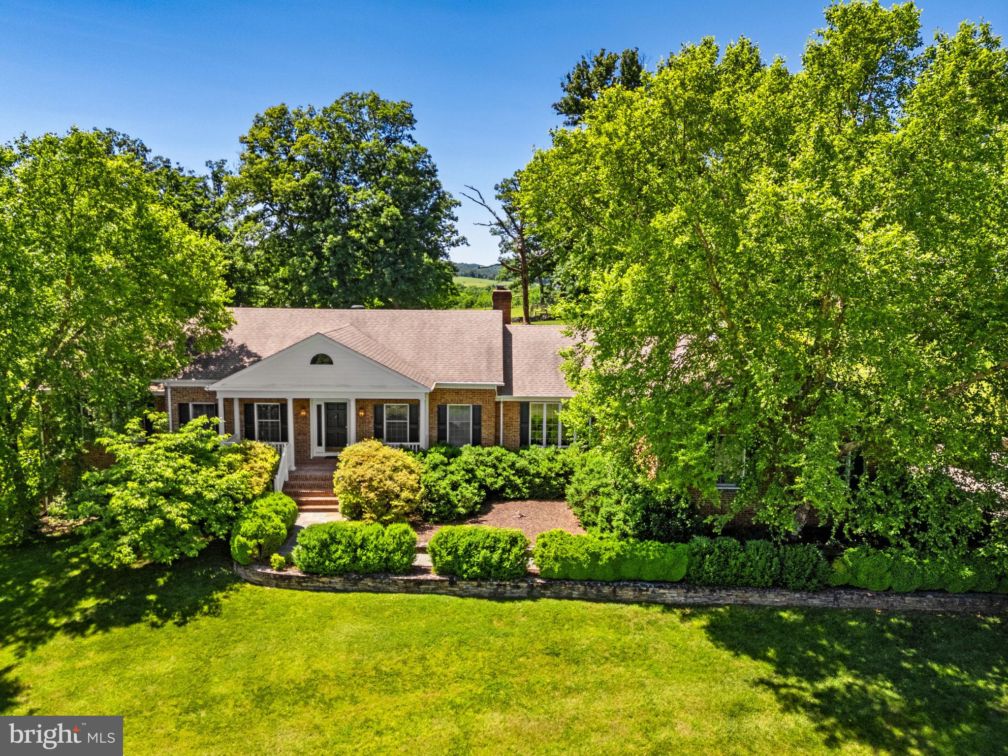 Just south of the charming village of Upperville, Stone Oaks is a beautifully maintained brick home privately situated on 14 acres with sweeping Blue Ridge Mountain views. A maple-lined driveway leads past open hay fields to the residence thoughtfully positioned on a hillside to capture spectacular sunsets and panoramic countryside vistas. A flagstone walkway framed by mature landscaping welcomes guests into a light-filled home featuring hardwood floors, generous living spaces, and a floor plan designed for both comfortable daily living and entertaining. The formal living and dining rooms enjoy beautiful natural light, while the updated kitchen opens seamlessly to a breakfast area, family room with fireplace, and renovated screened porch overlooking the landscape beyond. The main-level primary suite enjoys stunning mountain views and a luxurious bath. A guest bedroom and private office complete the first floor, while two additional bedrooms are located upstairs. The walkout lower level offers abundant storage and excellent potential for future finished living space. Just beyond the home is a detached all-brick two-car garage with water, electricity, and plumbing for a future bath, offering flexibility for workshop, studio, fitness, or guest space. A fenced vegetable garden with raised beds, electricity, and water provides an ideal setting for those seeking a small farm lifestyle. Surrounded by larger farms and protected countryside, Stone Oaks offers exceptional privacy while remaining convenient to Upperville, Middleburg, and the amenities of Virginia’s renowned horse and wine country. A rare opportunity to enjoy mountain views, peaceful surroundings, and a beautifully cared-for home in one of Fauquier County's most desirable locations.