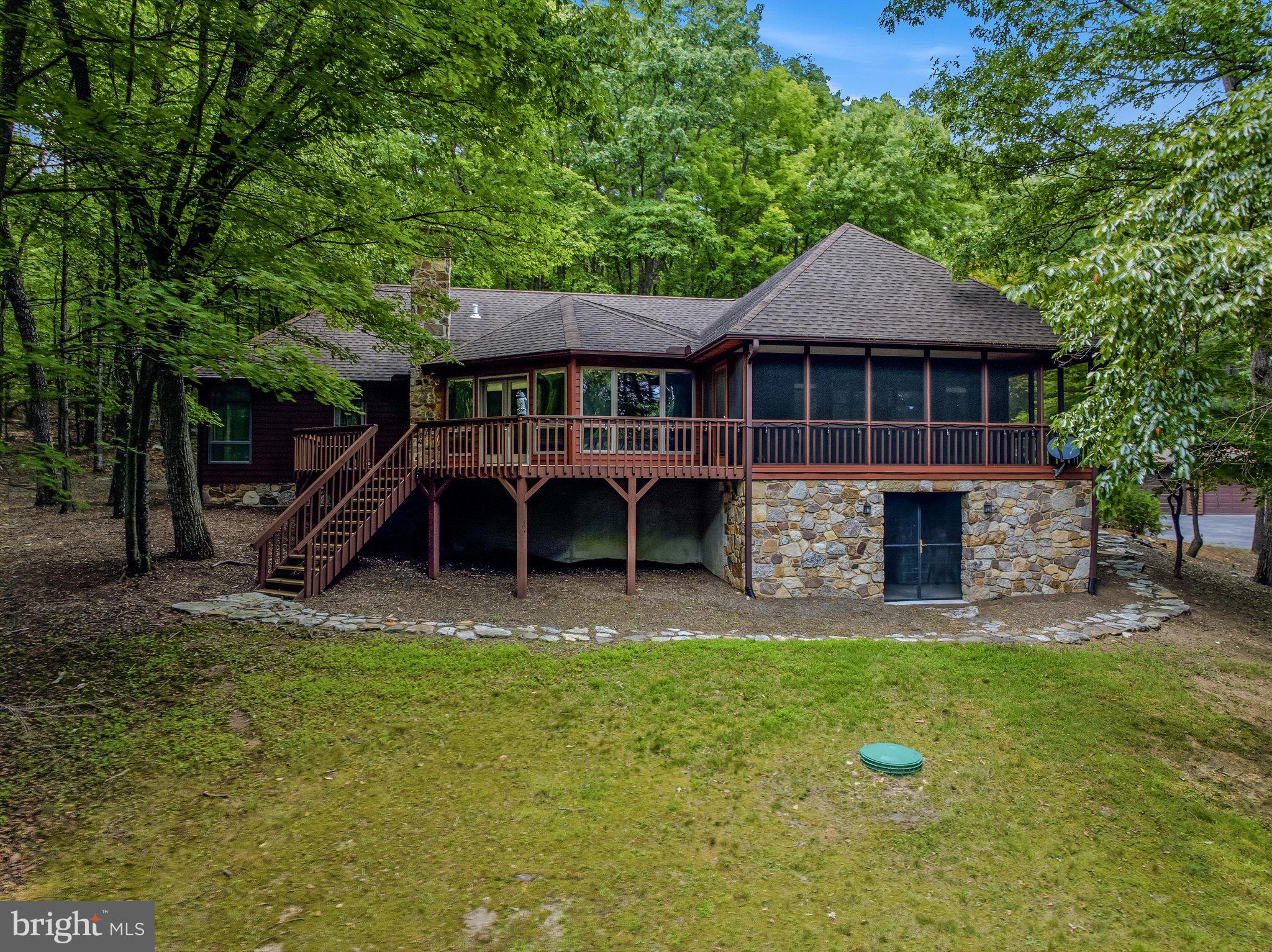 Discover this unique hidden gem on 4.22 wooded acres featuring a meticulously well-cared-for and updated cedar-sided 3-bedroom, 2-bath contemporary rancher with a paved, gated driveway and a detached two-car garage with 3rd bay workshop space. Designed to embrace the beauty of its surroundings, this home offers the perfect combination of comfort, privacy, and convenience.
The focal point of the home is the impressive floor-to-ceiling stone fireplace/woodstove, complemented by a wall of windows that fills the living area with natural light and provides access to the deck and screened porch—perfect for wildlife watching or simply enjoying the peaceful setting. The updated kitchen features Corian countertops, double ovens, and an open layout to the living/dining area, making entertaining easy and enjoyable.
The spacious owner's suite has access to the deck and includes separate his-and-hers walk-in closets and floor-to-ceiling windows leading into the ensuite bath with an oversized heated jacuzzi tub, double vanity, and walk in shower. Two additional bedrooms share an updated guest bath. You'll also appreciate the exceptional laundry room complete with a pantry, utility sink, and abundant storage.
The lower level offers a family room or office space, a utility sink, and additional storage. A clean, well-lit crawlspace provides easy access for maintenance. Additional features include dual 80-gallon water heaters, a regularly serviced Lennox heat pump, a new well pump installed in spring 2026, and enclosed storage beneath the deck for outdoor equipment. Cedar closet, custom blinds, recessed lighting and dimmer switches throughout.  New roof in 2008. Gas generator hooked into the house for extra peace of mind.
Whether you're searching for a full-time residence or a weekend getaway, this property checks all the boxes. Located just minutes from the outdoor recreation and amenities of Cacapon Resort State Park and the shops, restaurants, and attractions of Berkeley Springs, you'll enjoy the best of mountain living with convenience close at hand.