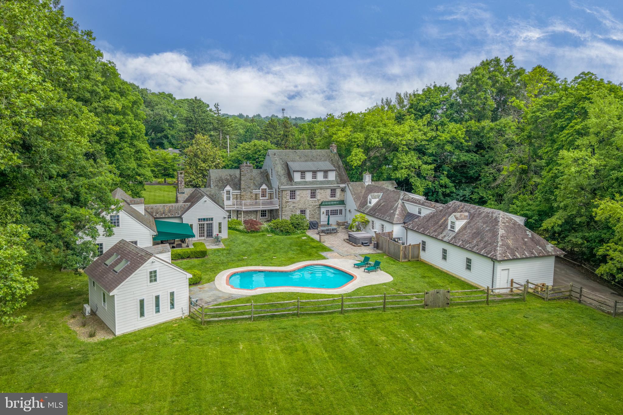 Presenting 107 E Mill Road, an exceptional Flourtown residence nestled on 2.28 private acres of mature trees, lush landscaping, and expansive lawn. Offering a rare sense of seclusion in a highly convenient location, the property combines peaceful surroundings with easy access to Flourtown, Chestnut Hill, and major roadways. Originally constructed in 1937, this distinguished Colonial has been thoughtfully expanded and enhanced over the years, including the addition of two substantial wings in 2000 and a beautifully appointed pool house in 2016. The result is a residence that offers impressive scale for entertaining while remaining warm, inviting, and functional for everyday living.
A gated circular front driveway leads to a slate walkway framed by mature trees. Inside, the center hall introduces the home's elegant yet inviting character. To the left, the formal dining room features classic wainscoting and oversized windows overlooking the front grounds. Beyond, the sun-filled kitchen offers terracotta tile floors, center island with seating, charming breakfast nook, and a bay window with views of the pool and rear yard.
Adjacent to the kitchen is an impressive recreation and entertaining space complete with a corner bar, beverage refrigerator, and ample seating. A rear staircase leads to a private office/bonus space and generous storage area above the game room and gym. A charming wine room with storage, full bath, and access to the attached three-car garage complete this wing.
The formal living room to the right of the center hall is anchored by a gas fireplace and framed by expansive windows that capture views of both the front and rear grounds. Nearby, the original wood-paneled study with slate floors, built-in shelving, and fireplace provides a cozy retreat.
Beyond the study, a dramatic two-story sitting room with vaulted ceilings and French doors opening to the patio connects to a versatile secondary living wing. This wing features a full kitchen, full bath, and an open-concept living area, offering exceptional flexibility for guests, extended family, or a private retreat. The lower level is dedicated to entertainment, featuring a home theater with projector and reclining seating for an immersive movie-night experience.
The second floor is accessed from the center hall staircase, where arched openings lead to the primary suite. This private retreat features a deck overlooking the grounds, a wall of custom built-in closets, and a bath with walk-in shower. Two additional bedroom suites, each with full baths, and a fourth bedroom complete this level.
The third floor provides exceptional flexibility with two additional bedrooms, a full hall bath, multiple walk-in closets, and a large cedar closet.
The lower level offers even more usable space, including terrazzo floors, abundant storage, a sauna, a spacious laundry room, and a comfortable lounge with fireplace that could easily serve as a fitness area, hobby space, or additional recreation room.
Outside, the grounds are truly spectacular. A relaxing setting awaits with an in-ground pool, hot tub, and multiple patios for dining and relaxation. A well-appointed pool house features a kitchenette, full bath, and stacked washer/dryer. The expansive level lawn provides ample room for recreation, outdoor gatherings, or a friendly game of football.
Offering a rare combination of privacy, acreage, and convenience, 107 E Mill Road is ideally situated just minutes from the shopping and dining destinations of Flourtown and Chestnut Hill, with easy access to Routes 309, 476, and Center City Philadelphia. Beautifully updated and maintained, this remarkable property is ready to welcome its next chapter.