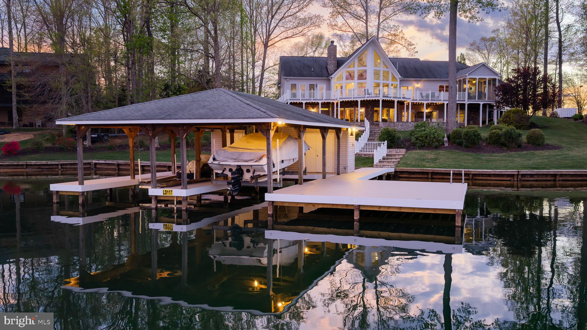 Gorgeous waterfront retreat on the private side of Lake Anna, ideally situated in the sought-after Noah’s Landing subdivision and offering breathtaking, unobstructed views along with high-speed fiber internet. With 180 feet of pristine, deep-water bulkheaded shoreline, this exceptional property is perfectly designed for the ultimate lake lifestyle. The impressive covered boathouse features all-new composite decking, two slips with electric lifts, a spacious sun deck with partial coverage for both sun and shade, and a convenient storage room—creating the perfect setting for relaxing, entertaining, and enjoying endless days on the water.
Back at the home, breathtaking lake views take center stage throughout this impressive 4-bedroom, 3 full bath, 2 half bath residence with over 5,400 square feet. The main level showcases soaring vaulted ceilings, a stunning wall of windows overlooking the lake, and a cozy gas fireplace. Enjoy a bright breakfast room, well-appointed kitchen with stainless steel appliances, and a separate formal dining room perfect for entertaining. A main-level office (or optional bedroom), mudroom, and two half baths add to the home’s functionality.
Upstairs, a charming loft provides the perfect space to unwind with a book or enjoy a quiet afternoon. The walkout lower level is made for gathering, featuring a massive family and recreation room with a stone wood-burning fireplace, a wet bar with full-size refrigerator, three bedrooms, two full baths, and ample storage. Outdoor living shines with an impressive patio, screened-in lakeside porch, expansive composite deck, and professionally designed hardscaping throughout. Additional highlights include two tankless water heaters, lake-fed irrigation, a paved driveway, and a 3-car garage. This exceptional property offers stunning views, an unbeatable location, and short-term rentals are permitted—making it an incredible investment opportunity or the lakefront dream home you’ve been waiting for. See Rental Projection in MLS Documents Section!