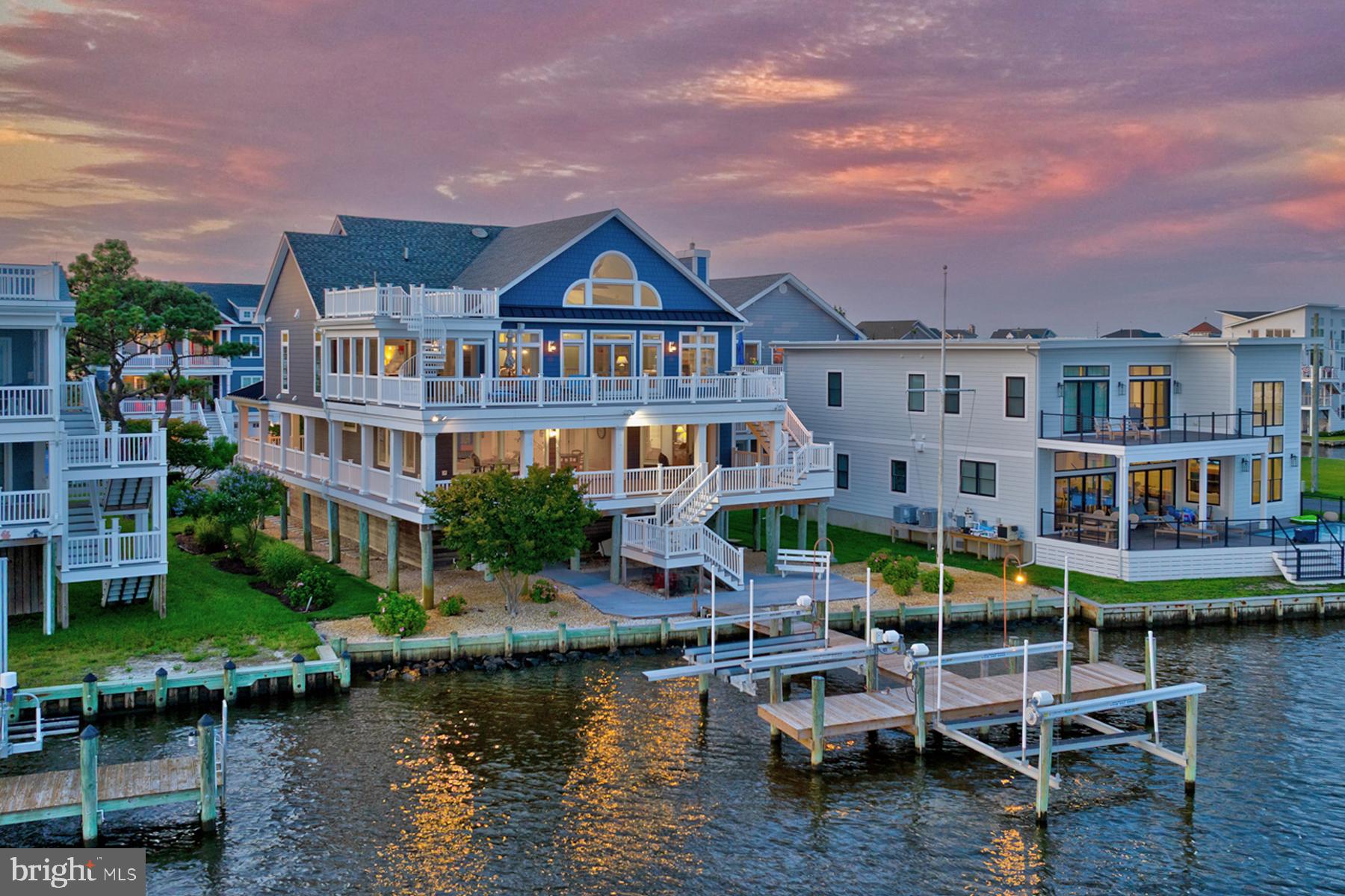 Exceptional Waterfront Retreat with Panoramic Southern Bay Views! This stunning, meticulously maintained waterfront residence offers sweeping southern exposure and expansive bay views, all within walking distance to the beach. Thoughtfully designed for boaters and coastal enthusiasts, this custom-built home showcases top-tier craftsmanship and attention to detail throughout. Boasting an open inverted floor plan to maximize water views, the home features 79 feet of bulkheaded waterfront, over 3,000 square feet of spacious decking and is ideally located on a quiet, non-thru street just minutes from downtown Bethany Beach. The main living level, accessible by elevator, is an entertainer’s dream, featuring an open-concept great room with soaring wood-planked cathedral ceilings, wide-plank hardwood floors, and a floor-to-ceiling raised-hearth fireplace. A wall of atrium sliders floods the space with natural light and opens to an oversized deck with sweeping water views. The gourmet kitchen is a chef’s dream, offering a center island with farmhouse sink, custom wood cabinetry, granite countertops, stainless steel appliances, beverage fridge, 6-burner range with pot filler, and a spacious walk-in pantry. Enjoy meals at the breakfast bar, in the elegant dining room, or alfresco on the screened porch with refreshing bay breezes. For breathtaking sunsets or stargazing, take the spiral staircase to the fourth-floor lookout deck, a perfect perch for cocktail hour. The primary suite is a serene retreat with private balcony access, a custom walk-in closet, and a luxurious spa-inspired bath featuring a frameless glass tiled steam shower, double vanity, and private water closet. The second level offers a cozy family room with coffered ceilings with wood inlay, ideal for games or movie nights, along with a second primary suite and three additional ensuite bedrooms, providing abundant space for large family gatherings and guests. Every room is designed to take full advantage of the tranquil coastal setting. Outdoor living is elevated with three levels of spacious decks and covered ground space, designed for relaxation and entertainment. Recent updates include new siding, an upgraded geothermal HVAC system, updated boat dock and dual lifts, and a whole-house water softener. The ground level includes generous storage areas, two outdoor showers, two covered parking areas, and a patio area overlooking the water. The elevated piling foundation ensures long-term peace of mind. With 80 feet of private bulkhead, two boat lifts, this property offers the ultimate coastal lifestyle. Schedule your private tour today and discover the exceptional comfort, elegance, and waterfront living this remarkable home provides.