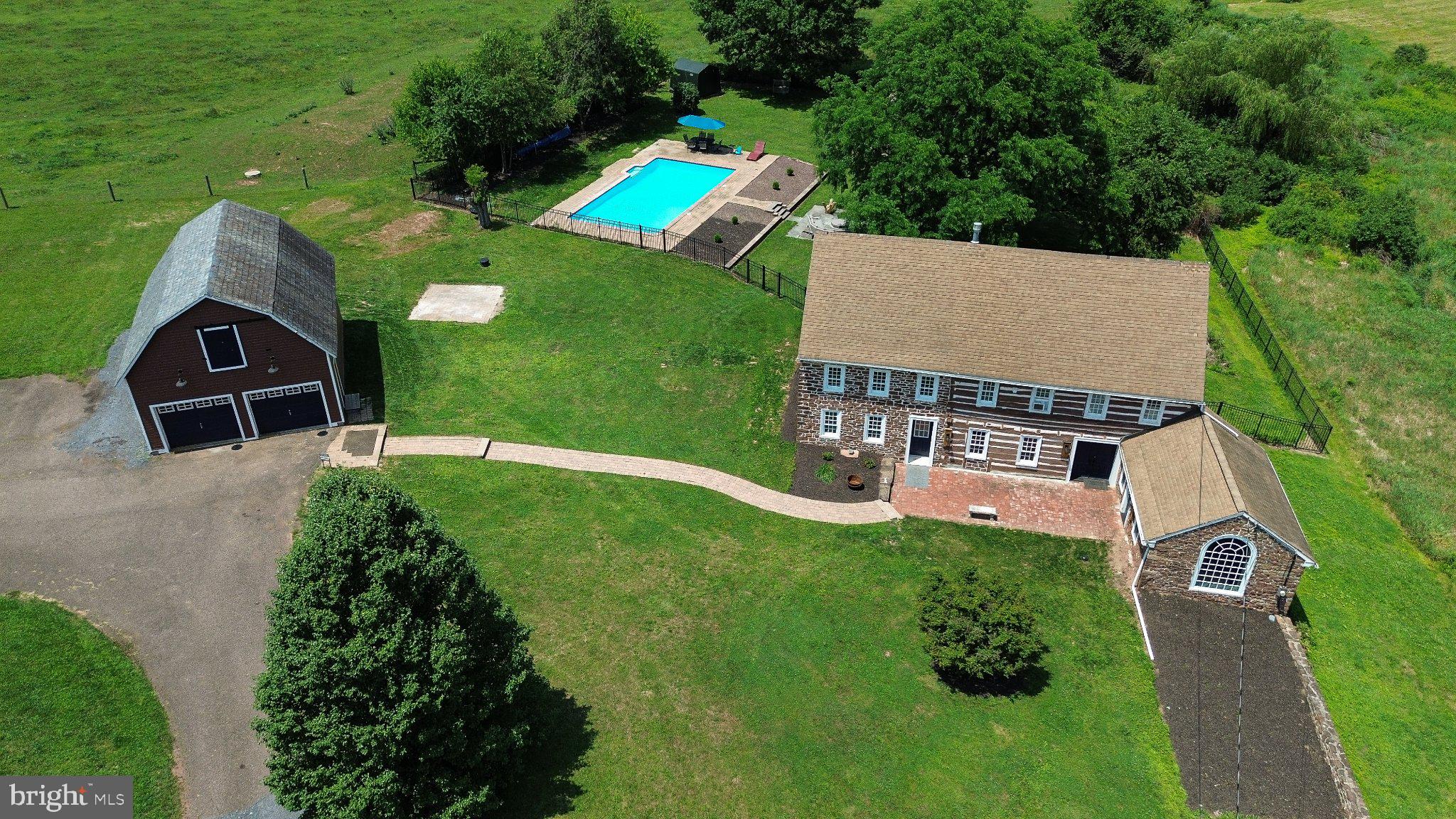 This log & fieldstone farmhouse was originally erected just after the birth of our nation in 1790, situated next to Cooks Creek & surrounded by picturesque farmland. Character & craftsmanship of yesteryear with modern updates & convenances gives this estate property the best of both worlds. As you approach the post & beam barn-garage & stroll down the paver walkway it is apparent that this property is extraordinary. Your eye is immediately drawn to the stunning fieldstone & massive logs that constitute the outer walls. The depth of the outer walls becomes clear when entering the double door entryway. Enter the original log portion of the home onto a massive piece of Uba Tuba granite, surrounded by gorgeous wide plank pine flooring throughout the large, open, living room. Exposed, hand hewn beams, posts & logs exude character and the fireplace offers warmth on cold winter nights. Walls that are not exposed stone or log, are framed, insulted & drywalled for efficiency. Step into, what is believed to be the original summer kitchen offering hand hewn, exposed beams and stone accent wall with huge arched window. Would make for an incredible formal dining room, game room, bar or office with separate outdoor entry. At the other end of house resides the heart of the home. The fieldstone addition (Added in 1811 by A.E. Moyer) gourmet kitchen has been completely renovated top to bottom including: Via Lattea granite island with farm sink, dishwasher, pendant lights, timber framed posts, 6 burner Forno range, white shaker cabinetry, & exposed stone corner wall. Meander through the massive 236 year old logs into the rear addition to the bright & airy family room flooded in natural light, pine wood ceilings, exposed log wall, & slider to the rear deck. With a 1st floor bedroom, this home gives the option for multi generational living. The bedroom features wood ceiling, exposed log wall, solid wood entry door & double barn door closet.  Across the family room & down the stunning hall with exposed stone, built in bookshelf, wood ceilings & accent wall & through the solid wood entry door into the stunning full bath featuring: custom reclaimed barn wood vanity with granite top, twin Moen facets, oversized shower with glass tile & door, tile floor, random width pine board accent wall & huge linen closet. Next door you’ll find a dream laundry room with granite folding top, shaker cabinetry, oversized linen closet, washer, dryer & chest freezer. Up the custom staircase with ornate spindles, Newel posts & chandelier to the upper level. Bedroom 2 offers plenty of space, featuring exposed log wall, beams & a full length closet. The master bathroom is cavernous featuring a gigantic soaking tub set in corrian, huge vanity with brass facet, oversized double door closet, glass door fully tiled shower & tile floor spanning the width of the house. The stunning master bedroom with soaring vaulted ceilings, exposed beams, stone access wall, his & hers closets & pumpkin pie spiral staircase to the attic landing. The original wide plank attic boards are a sight to be seen, with plenty of room for storage. Head down the spiral staircase to the original, stone basement with hand hewn floor joists, gigantic walk-in fireplace, modern wiring, 200 amp service, PEX & PVC plumbing, UV light, sediment filter, 3 zone tankless boiler & 4th zone kitchen radiant floor heat. Back to the family room and head out the slider to the composite rear deck with aluminum railings. The crown jewel of the yard is a 30,000 gallon in-ground pool featuring brick coping, blue & white tile and paver decking, perfect for relaxation on a beautiful summer day with farmland as your backdrop. Mature trees for shade, patio and fire pit area, this back yard oasis is ready for entertaining. Set in the country, yet just minutes to 309, 476 & 78 as well as fine dining and shopping. Welcome home!