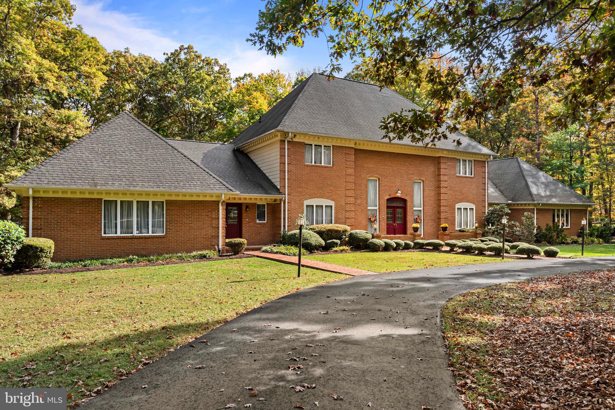 Welcome to this custom, all brick, French Colonial in the coveted and private Carriage Hills Estates neighborhood. This stately home is unlike anything on the market. With the large circular driveway and the stunning roof lines, this 5 acre property is a sight to see! The inviting brick front porch welcomes you inside to the grand 2 story foyer and dual staircase. Original high-quality oak hardwood floors, crown molding, wood beams and chandeliers surround you with character and warmth in the foyer, dining room and formal living room. The kitchen perfectly combines space and function with a center island, rich cabinets and stainless steel appliances. From the kitchen, the cozy family room is anchored by a handsome gas fireplace with doors that open to the rear 1000+sq foot brick patio. A discreet mini wet bar leads into the library where you can sit and read a great book. French doors invite you into the regal primary suite, located on the first floor. You will find 2 sitting rooms, a relaxing bedroom, and a grand ensuite and boudoir, which have to be seen to be appreciated.  From the foyer, wood steps, protected by plush carpet, connect you to the second level. Centered upstairs is another generous primary suite complete with a bathroom, a brick fireplace and multiple closets. To the right is a comfortable sized bedroom with an attached bathroom and to the left are 2 more bedrooms that share a bathroom. This beautiful lot is adorned with an assortment of mature trees, providing privacy and scenic views. Other things to note: There is an office inside the garage with its own entrance. Two half bathrooms are on the main level.  Character, charm, and room to spread out abound in this home.  An additional perk is county water and sewer service the home. If you value a home with quality construction, a unique floor plan, peaceful surroundings, and amazing possibilities, this one is a gem!