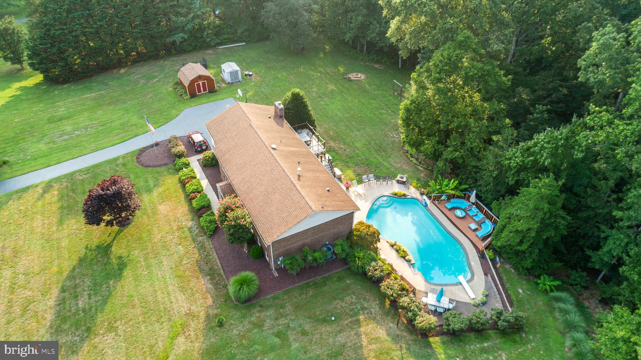 Tucked away on a private, low-traffic street with the peaceful feel of a cul-de-sac, this exceptional four-sided brick home offers more than 3,000 square feet of living space on a flat, mostly cleared four-acre lot. Located in sought-after Dunkirk, the property combines peaceful country living with convenient access to shopping, dining, commuter routes and the greater Washington, D.C., and Annapolis areas.

Double French entry doors—both fully operational—welcome you into a bright and inviting main level featuring random-width hardwood flooring throughout most of the space. The open floor plan and abundance of windows create a natural flow while filling the home with sunlight. A spacious dining area at the front of the home can comfortably accommodate a large table for holidays and special gatherings. The expansive front-to-back family room offers plenty of space for movie nights, entertaining or simply relaxing beside the wood-burning masonry fireplace.

The kitchen features an impressive collection of 42-inch, cathedral-topped cabinetry, granite countertops, a matching granite backsplash and upgraded stainless-steel appliances. These include a refrigerator with ice and water in the door, built-in microwave, dishwasher and solid-surface range. A deep stainless-steel sink, extensive cabinetry and generous counter space provide excellent functionality and storage. The extended countertop between the kitchen and family room includes an overhang with comfortable seating for four full-size chairs.

The spacious primary bedroom overlooks the pool and backyard oasis and includes two separate closets. Its beautifully updated private bathroom showcases an oversized shower with custom translucent tile extending from floor to ceiling and a full glass enclosure. Three additional bedrooms are located on this level, including one currently used as a home office. The hall bathroom offers a granite-topped vanity and a tub-and-shower combination.

The finished lower level significantly expands the home’s versatility. It includes a fifth carpeted bedroom, an updated full bathroom and a complete second kitchen with abundant cabinetry, a refrigerator, dishwasher, built-in microwave and solid-surface range. This flexible space is ideal for extended family, overnight guests, recreation or large gatherings. The HVAC system also includes oil heat backup for added peace of mind.

The garage is well equipped for projects, hobbies and storage, featuring a stationary utility tub, a large center-island workstation and convenient tool-storage space. The pool equipment is thoughtfully housed inside the home’s storage room, helping protect it from the elements and harsh winter temperatures.

The backyard is where this property truly becomes extraordinary. Extensive landscaping and stonescaping surround a custom gunite swimming pool that has been beautifully refreshed, with the coping and tile reinstalled approximately five years ago. Custom lighting around the pool and outdoor living areas creates a stunning atmosphere for evening gatherings.

Multiple outdoor entertaining spaces include a grade-level patio, an upper-level deck and a large, one-step platform deck positioned beside the tree line, where afternoon shade provides a comfortable place to relax. The patio and deck areas were redone within the past month. Several sheds offer additional storage, while a custom-built private cleanup station provides the perfect place to wash up after cookouts, seafood feasts and crab gatherings. Recreational trails cut through the rear portion of the property add yet another way to enjoy the expansive four-acre setting.

Offering five bedrooms, three full bathrooms, two kitchens, substantial brick construction and a resort-inspired backyard, this remarkable Dunkirk property delivers the privacy, flexibility and entertaining space that are increasingly difficult to find.