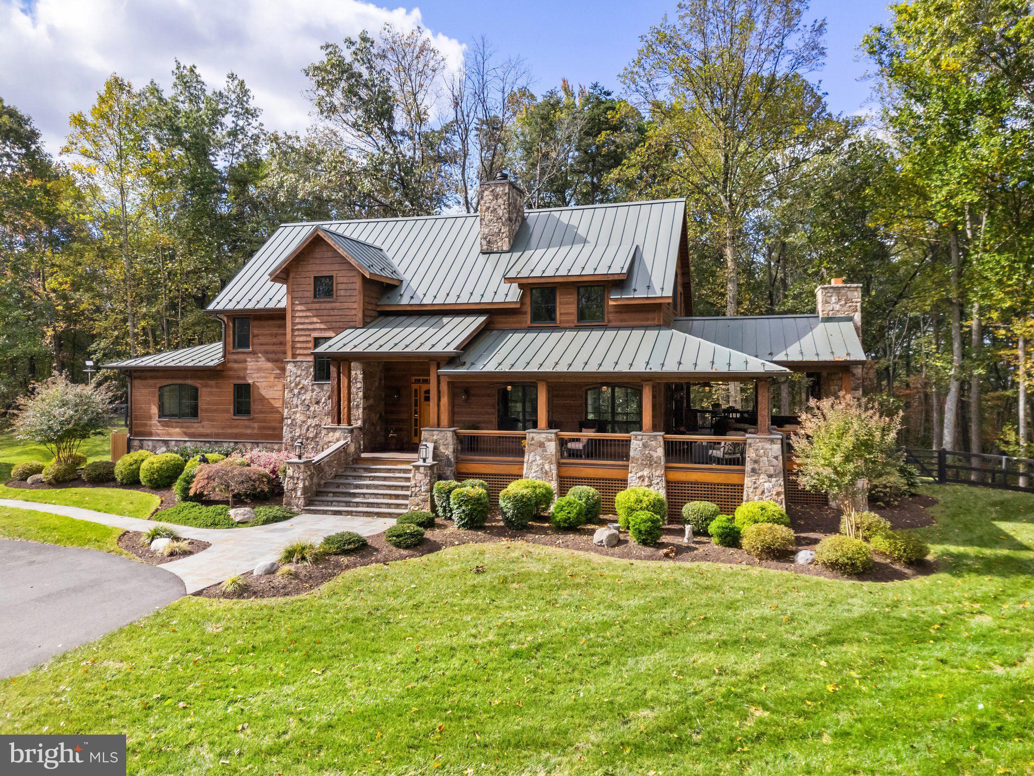Tucked away on 33 private, wooded acres in the rolling hills of Virginia’s Piedmont, this custom-built 2018 home offers a secluded retreat in the heart of wine and horse country, just minutes from the Village of Orlean and an hour from Washington, D.C. The paved drive stretches through serene, wooded views, leading to a gated entrance that opens to this incredible property, where nature truly abounds. Designed in a craftsman log style, the home features durable concrete log siding and a metal roof for longevity. A grand stone staircase, accented with lanterns, welcomes you to the expansive wraparound porch with Trex-style decking, iron spindles, and mahogany handrails. The outdoor living space is designed for year-round enjoyment, featuring a wood-burning fireplace, cathedral ceiling with heaters, recessed lighting, and a ceiling fan, plus a back stone patio with retaining walls and a hot tub, and a side stone patio with a firepit. Step inside, where the attention to detail sets the tone for the home’s exceptional craftsmanship. The heated stone floors lead into the Great Room, featuring a soaring cathedral ceiling, wooden beams, a floor-to-ceiling gas fireplace, and arched Windsor windows that bathe the space in natural light. The spacious Dining Room, illuminated by an impressive chandelier, flows into the Gourmet Chef’s Kitchen, where top-tier KitchenAid appliances, a spacious curved island with barstool overhang, a CopperSmith hammered copper range hood, and custom soft-close cabinetry create a stunning focal point. Granite countertops extend seamlessly up the wall as a backsplash, and a copper farm sink offers serene views of the private backyard. The main hall leads to a Half Bath with stone floors, a designer vanity with a vessel sink, and a Laundry Room featuring a washer/dryer, built-in dog kennels, and a PlexiDor dog door. A barn door leads to a private wing featuring the Owner’s Suite, a spa-like Primary Bath, and a versatile room that can serve as a Study, Sitting Room, Nursery, or extra Bedroom. This additional space includes custom built-ins and a French door opening to the expansive backyard patio. The Owner’s Suite offers heated stone floors, Windsor windows, a walk-in closet with custom organization, and a luxurious bath with double quartz vanities, heated tile floors, a walk-in shower with a leathered quartz accent wall, a jetted tub, and a remote-controlled shade. A wooden staircase, showcasing custom built-ins and a window seat, leads to the Loft, overlooking the Great Room. Bedrooms 2 and 3 each include heated floors, large closets, and upgraded en-suite half baths, sharing a spa-inspired bath with a separate shower and freestanding tub. The Finished Lower Level features a walk-out stone staircase, a Rec Room with professionally stained heated concrete floors, custom built-ins, a projector/screen, and built-in speakers, and a Game Room. Additional lower-level spaces include an Exercise Room, a Den/4th Bedroom, a Full Bath, and ample storage. Notable features: whole-house generator, outdoor shower, water filtration system, heated floors throughout, Windsor windows and doors, alder wood interior doors, and Starlink internet. The oversized 3-car garage includes a finished interior, an unfinished upstairs storage area ready for future conversion, a water heater, washer/dryer hookups, and a sink. The property also includes two additional outbuildings. A truly one-of-a-kind home, offering a private wooded retreat with modern comforts and timeless craftsmanship.