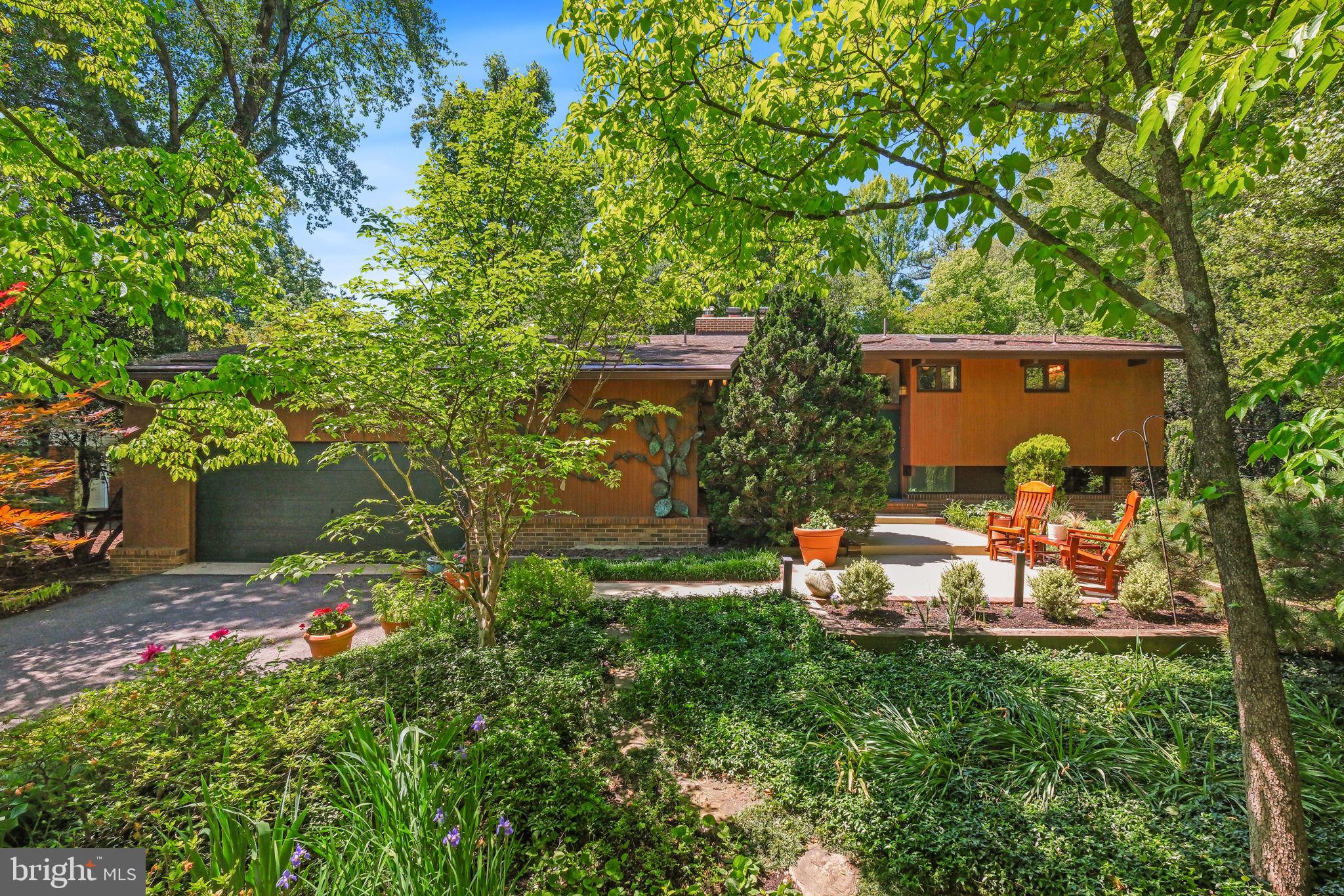 Mid-century modern design becomes a living work of art at 7908 Fenway Road—an extraordinary residence where architecture, landscape, light, and nature exist in constant dialogue. Like a painting carefully composed frame by frame, every room, every sightline, and every wall of glass was intentionally designed to capture the surrounding scenery and changing seasons. If Claude Monet had envisioned a modern home in 1983, it may have felt something like this—immersed in light, connected to nature, and crafted to make everyday living feel artistic and serene. Designed and built by Acorn Deck House Company, renowned for its decades-long legacy of creating architecturally distinctive custom homes, the residence reflects a philosophy centered on harmony between structure and setting. Exposed post-and-beam construction creates uninterrupted open spaces, while soaring wood-clad ceilings, skylights, and expansive walls of glass dissolve the boundary between indoors and outdoors. Sunlight filters through the home throughout the day, casting shifting patterns across warm natural materials and framing curated views of the surrounding gardens and landscape. Notable improvements include a new 50-year roof in 2018, new HVAC in 2022, chimney pointing in 2024, and a new hot water heater in 2026. A significant 2003 renovation by DRL and Associates reimagined the kitchen and bathrooms with a refined, high-end approach that complements the home’s original architectural character. Tucked along a quiet street in Bethesda’s highly sought-after Carderock Springs community, the home provides approximately 2,401 square feet across two levels, with 4 bedrooms, 2 full bathrooms, dual staircases, extra-deep closets with built-in organization systems, and multiple walk-in storage areas. The outdoor setting feels equally curated and immersive. A fully fenced private backyard unfolds like a botanical retreat, complete with exterior lighting, a large walk-down deck, flagstone walkways, a pergola with an adjacent millstone fountain, and professionally designed landscaping with flowering plantings, mature trees, and garden beds.  A private drive and front patio welcome you inside, where the main living space immediately reveals the home’s architectural impact. The great room and kitchen are anchored by a dramatic seven-foot freestanding brick fireplace and elevated by cathedral wood ceilings, skylights, hardwood floors, and contemporary monorail track lighting. Multiple glass doors create seamless transitions to the deck and gardens beyond, making the landscape feel like an extension of the interior living space. The gourmet kitchen blends craftsmanship and functionality with granite countertops, Dacor stainless steel appliances, an integrated paneled refrigerator, custom cabinetry, a deep farmhouse sink beneath a garden window, and extensive pantry storage with roll-out drawers and built-in organizers. Nearby, a secondary staircase connects to a landing with additional pantry and closet storage, garage access, and a side entrance to the front patio. Privately positioned on the opposite side of the main level, the primary suite serves as a peaceful retreat with vaulted ceilings, serene garden views, extra-deep closets, and a ceiling fan. An additional bedroom and a renovated full bathroom complete the main level. The lower level continues the home’s cohesive architectural aesthetic. Offering a spacious family room centered around a second brick fireplace provides built-in cabinetry and partial daylight exposure. Beyond, a flexible bonus area with extensive counter space and storage is ideal for use as an art studio, exercise room, or more. This level also includes 2 additional bedrooms, and a full bathroom. Ideally located near parks, recreation, nationally recognized golf courses, dining, shopping, and major commuter routes—and served by highly regarded public and private schools—7908 Fenway Road, is an immersive architectural experience.