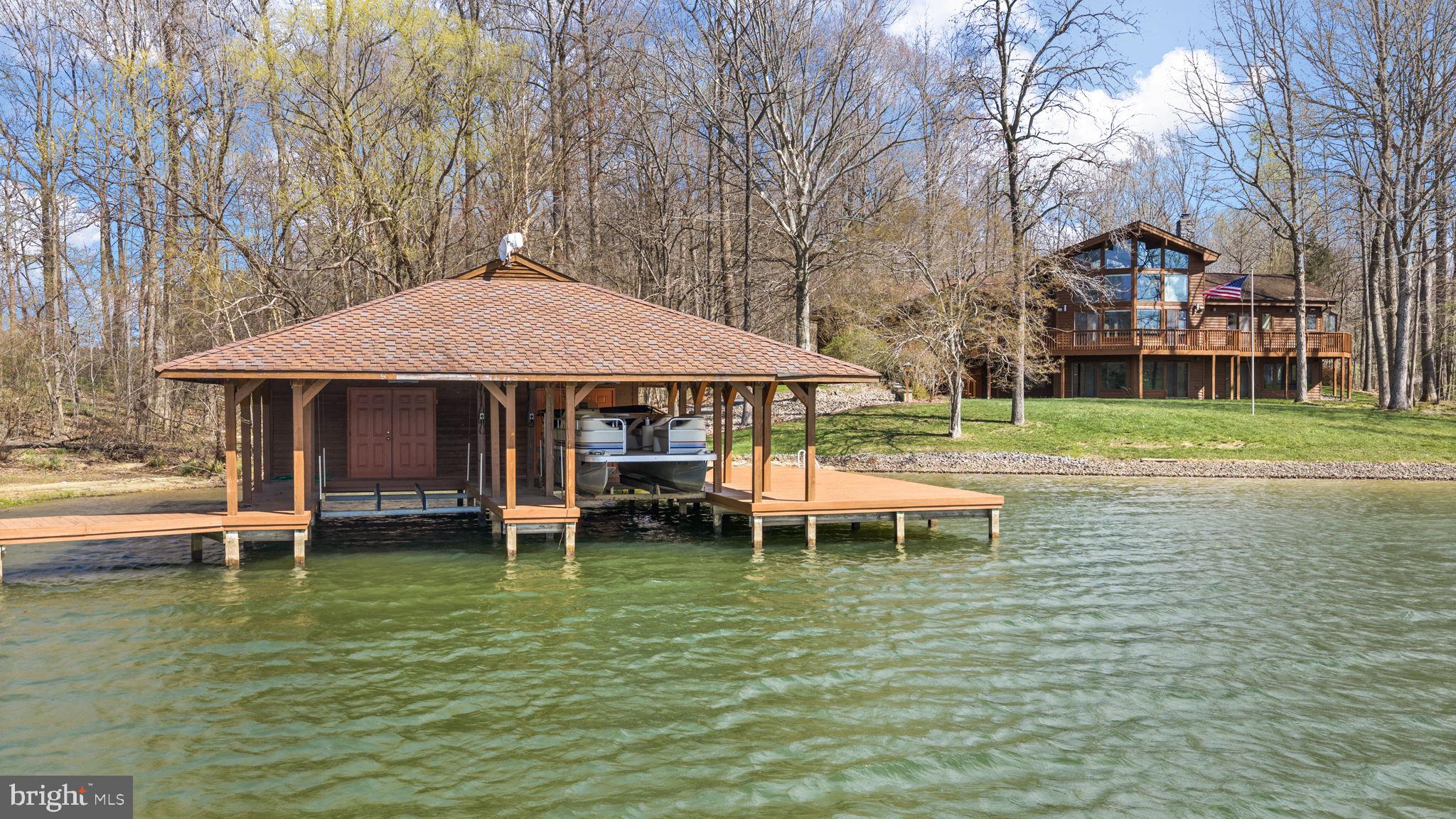 A rare and extraordinary opportunity at Lake Anna, VA! This stunning waterfront Lindal Cedar home on the private side of the lake offers the perfect blend of lake living and mini farm potential, all set on 6.49 picturesque acres. Approximately 700 feet of riprapped shoreline, plus a private pond, this one-of-a-kind property delivers unmatched waterfront living with breathtaking western sunset views. With over 4,400 square feet, 6 bedrooms, and 3.5 baths, there is room for everyone to relax and enjoy. Inside, the home showcases soaring vaulted wood ceilings, a dramatic wall of windows overlooking the lake, and a striking stone gas fireplace. The open-concept design seamlessly connects the family room, dining area, and kitchen—perfect for entertaining. The kitchen features granite countertops, a Jenn-Air double wall oven, and a Bosch dishwasher (just 2 years old). The main-level primary suite is complete with an atrium-style glass sitting area to soak in the views and a spacious walk-in California Closet system. Upstairs, a loft with a full bath offers flexible space for a bedroom, guest suite, or home office. The walkout lower level expands your living space with a large family room, four additional bedrooms, a full bath, and a utility/storage room—ideal for hosting guests or multi-generational living. Outdoor living is just as impressive, with a large upper-level deck and lower-level patio overlooking the water. Follow the path down to your covered boathouse with electric lifts, storage, and a sun deck. There is also a gazebo by the water. Additional highlights include a whole-house speaker system, geothermal heating, fully paid-off solar panels (just 3 years old), reverse osmosis and water filtration systems, a 2-car attached garage, and a paved circular driveway. For those dreaming of a mini farm, the property is half fenced and ready to go, with multiple outbuildings, barns, run-in sheds, and a separate well that services the outbuildings and livestock. Located in a small 7-lot subdivision with no current HOA dues (covenants and restrictions do apply), and a recently paved road with a future maintenance agreement anticipated. This is truly a once-in-a-lifetime Lake Anna retreat offering space, privacy, waterfront beauty, and endless possibilities.