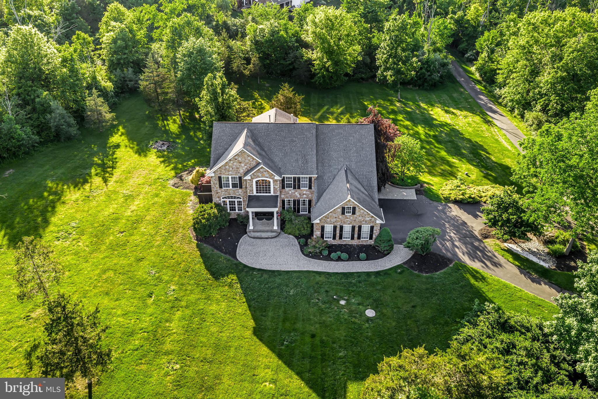 Welcome to 6723 Point Pleasant Pike, a beautifully appointed estate residence set on 3.51 acres in desirable Plumstead Township all within close proximity to the Delaware River and Ralph Stover State Park. This exceptional home offers an expansive and versatile layout featuring 4/5 bedrooms, 4.5 bathrooms and seamlessly blends timeless architecture with high-end modern functionality. Nestled in a serene Bucks County setting, the property delivers exceptional privacy and sweeping sunset views over a wooded backdrop, creating an ideal environment for both relaxing and entertaining.

A grand two-story foyer welcomes you through double front doors, showcasing rich hardwood flooring that extends throughout much of the main level and boasts a striking butterfly staircase that sets an elegant yet inviting tone. The thoughtfully designed layout connects formal and casual living spaces with ease, ideal for both everyday living and entertaining.

At the heart of the home is the expansive gourmet kitchen, featuring a large center island, stone peninsula with seating, maple cabinetry, high-end stone and granite countertops, a dedicated pantry, double wall ovens, and a gas cooktop. The kitchen flows seamlessly into the sun-filled breakfast room surrounded by floor-to-ceiling windows and a glass door that provides direct access to the expansive Brazilian Walnut deck overlooking the private rear backyard. The impressive two-story family room offers brand-new carpeting and a striking gas fireplace beneath soaring ceilings, creating a warm and inviting focal point.

The main level continues with a formal dining room featuring a convenient wet bar, perfectly connected to the kitchen which makes entertaining a breeze. A formal living room offers an additional refined gathering space, while a private first-floor office with French doors provides an ideal work-from-home setting. A newly updated half bath, first-floor laundry, and direct access to the oversized three-car garage complete this level.

Upstairs, newly carpeted hallways lead to four generously sized bedrooms. The primary suite is a true retreat, featuring an accent stone wall, two walk-in closets, and a beautifully updated five-piece en-suite bath designed for luxury and comfort. A spacious princess suite boasts its own private bath, while two additional bedrooms share a well-appointed Jack and Jill bathroom, offering both privacy and convenience.

The fully finished lower level expands the living space with a large living/recreation area and oversized custom wet bar with seating. A built-in refrigerator, sink and stone access wall serves as the centerpiece for the room and is an ideal extension of the home for entertaining and everyday enjoyment. Additional finished areas include a gym that can function as a potential fifth bedroom, a private office, a brand-new full bath, and multiple flexible spaces for media, fitness, or hobby space. Built-in storage benches and ample additional storage enhance the ability to put away items that are not needed everyday.
Off the main living area are French doors leading to the patio with built-in firepit. You will also encounter a tranquil fountain feature and paver walkway along with steps leading to the upper level deck. The grounds overlook peaceful natural surroundings, creating an ideal setting entertaining and also enjoying quiet evenings at home.

Located in Plumstead Township within the Award winning Central Bucks School District, and offering convenient access to New Hope, River, Stover Park, Doylestown Borough, and major commuter routes, this home delivers an exceptional blend of luxury, space, and location. This home represents a rare opportunity to own a truly distinguished Bucks County Estate with all the modern amenities that you will enjoy.
