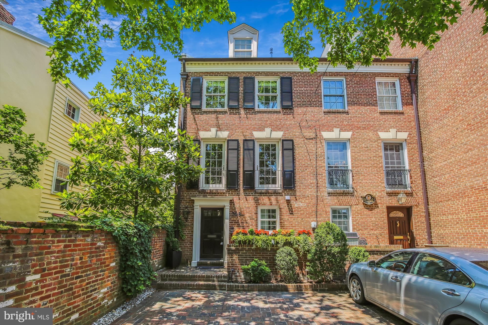 Welcome home to this meticulously maintained and updated four level townhome located in the very heart of Old Town Alexandria. Set back from the street in a quiet setting with a private brick-paved parking space just steps to your front door, which is illuminated by a gas lantern reminiscent of the earlier days of this historic city. As you enter the spacious foyer lined with an exposed brick wall and limestone floor your eye is immediately drawn to the inviting vista of the lush back patio.  As you pass through the gracious arch and down two steps, you enter into the high ceilinged Living room with double sets of tall French doors with light streaming in from the west. The large fireplace features a beautiful millwork surround and a gas log set for easy enjoyment. On the east wall the entry arch is repeated with a lighted display and entertainment center to the left and in the center, behind stunning antique arched doors, is a wet bar with a marble top, refrigerator and custom cabinetry and shelving to make for easy entertaining. The French doors lead you to a remarkable oasis in the city with a  two tiered brick patio highlighted by a stacked stone raised flower bed along the back. Lined with lush landscaping and trees, this fully fenced and lighted retreat also offers a garden storage shed tucked in a corner and a gate to the back easement. Also on this entry level and to the right of the foyer is a powder room for guests and a large foyer closet with customized cabinetry for additional storage and a bonus sink set in a granite counter ideal for cleaning up after gardening.   As you enter the second level,  to the right is an inviting Kitchen/Family room with exposed brick walls and a large picture window facing south flooding the space with light.   The back wall is lined with French doors leading to an iron balcony overlooking the back garden and to the right is a wood-burning fireplace with a lovely custom copper and glass door and a brick hearth.The kitchen walls are lined with custom cabinetry and marble countertops and the Sub-zero refrigerator is hidden behind matching doors.  The large custom island with marble countertop contains the Wolf electric oven and the microwave drawer by Sharp along with storage drawers and has room for casual dining. The six burner gas cooktop by Wolf sits under a custom range hood and the under cabinet lighting highlights the brick backsplash. At the front of this level sits a lovely Dining room with dentil crown molding and French doors and juliet railings bringing in the eastern daylight. The end wall is lined with custom cabinetry with a marble buffet and fabulous storage for all of your entertaining items.    The third floor offers a primary bedroom suite with an exposed brick wall on the right, a wall of custom closets and a sumptuous marble bath with a large soaking tub, large frameless glass shower with a rain head and a long double vanity. The second bedroom also offers an ensuite bath in marble with a frameless walk-in shower and custom shelving in the bedroom.  The fourth floor features a large third bedroom with a built-in Murphy bed so can serve as flex space as it has multiple storage closets and plenty of room for a desk or entertainment pieces. It also has a pull down stair to a floored attic for extra storage. Also on this level is a third full bath beautifully remodeled with additional storage in the eaves and a laundry closet with brand new Bosch washer and dryer.   Additional features include two zone HVAC and a gas tankless on-demand hot water heater. Both fireplaces have chimney liners and chimney caps and the roof was replaced in 2010. All rooms are wired for internet and sound and the electronic media controls are housed in the foyer closet. Recessed lighting and abundant storage are featured throughout the hose and both front and back exteriors have ground and uplighting.