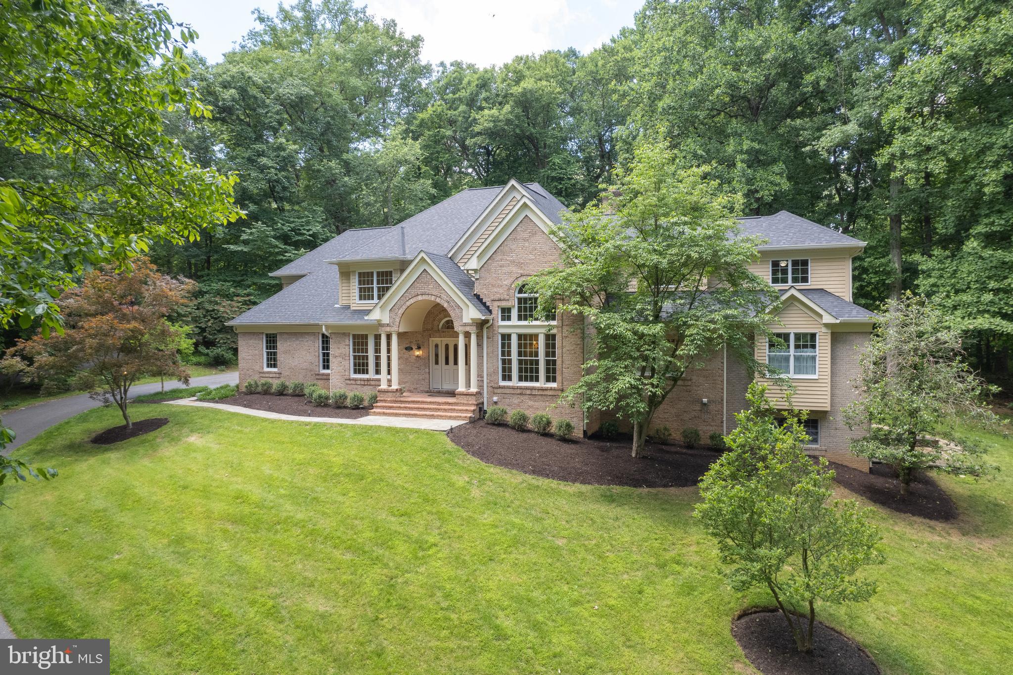 Fabulous brick transitional residence nestled on three wooded acres in the cul-de-sac community of Triadelphia Woods. Spacious and open flowing floor plan exudes elegance, quality design and workmanship. Opulence greets you upon entering the home with a grand foyer with two story vaulted ceilings, a formal living room with two story ceilings, a formal dining room dressed with all the trim, and newly refinished hardwood floors throughout the main level. A gorgeous, bright and new chefs-delight kitchen is dressed with 42" cabinetry, transoms, stainless steel appliances, quartz countertops and a breakfast room overlooking the back yard. Walk-out to screened-in porch and access the stylishly equipped butler's pantry, mudroom and half bath. The kitchen is adjoined to a magnificent great room adorned with two story ceilings, a brick wood-burning fireplace, ceiling fan, custom built-ins, and a wall of windows overlooking the walk-out to the beautiful rear stone patio and private yard.  The primary wing is housed on the main level and features a wet bar area with a wine cooler and ice machine, an office/library with a two-sided wood-burning fireplace shared with the primary bedroom suite. The primary suite features illuminated tray ceilings, plantation shutters on all the windows, a huge walk-in cedar California Closet, a laundry area, and a renovated bathroom with dual sinks, ceramic floors, separate tub and a huge walk-in shower. The second floor houses five huge bedrooms and three newly remodeled ceramic bathrooms, a second washer and dryer set and plenty of closet space. The fully finished walk-out basement offers a ton of flexibility as additional living space, an in-law or nanny suite or rental opportunity. The basement is equipped with at least one bedroom, a full bath, a spacious kitchenette with custom cabinetry, a family room with a gas fireplace, a billiard room, a media room with a projector and a 15' x 8' wall screen and stained concrete floors. There is also an additional room that has an abundance of natural light and walk-out to the patio and side yard. This lovely home provides great entertaining spaces inside and out. The property is served by private well and septic, propane gas heat, hot water and cooking, and 400 AMP electric service. Ample parking and storage is provided with an attached two car garage and a detached over-sized two car garage along with unfinished attic space that could be a future office, nanny suite or rental. 12' x 10' Log Playhouse also conveys.