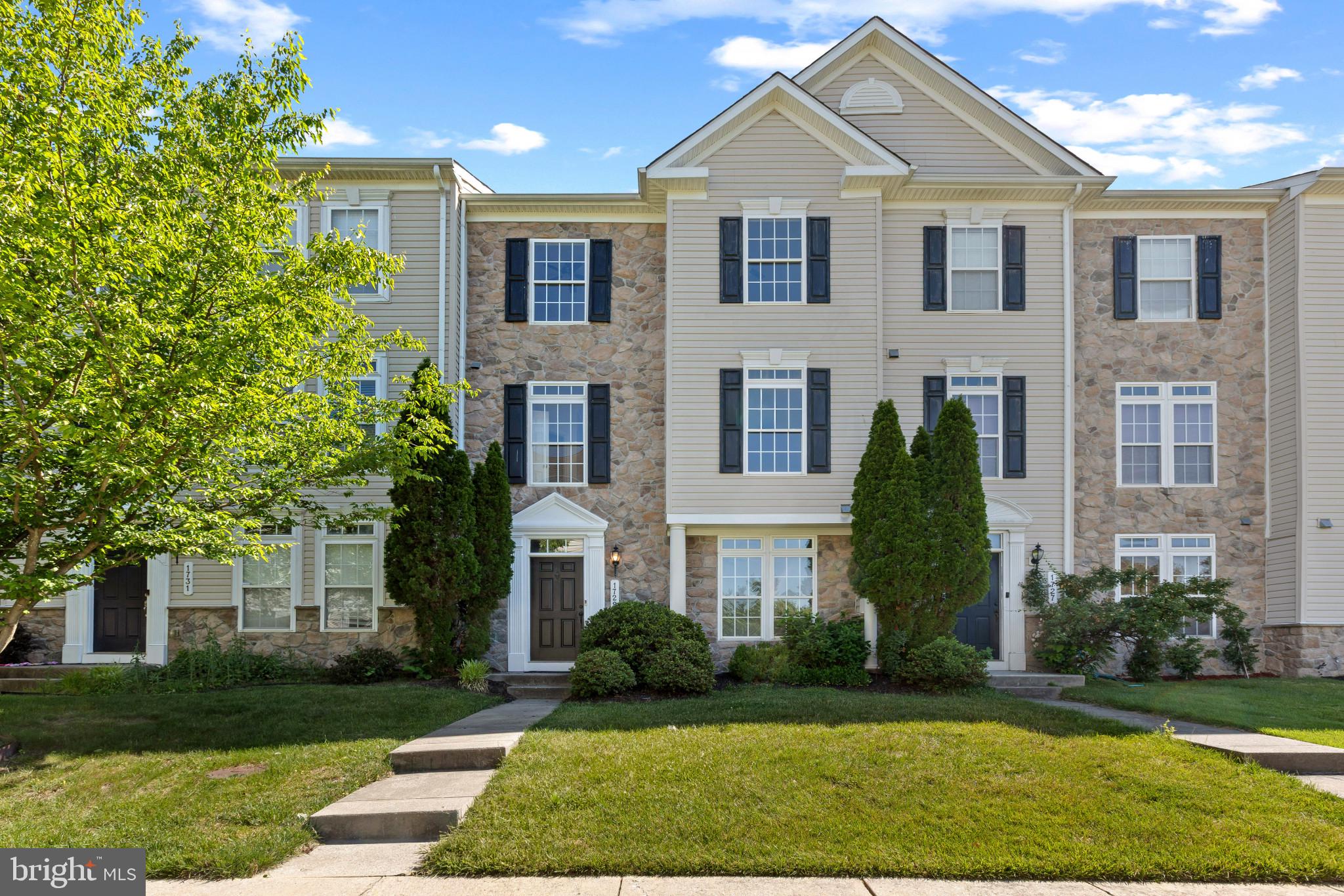 Beautifully maintained stone-accented Colonial-style townhouse offering 4 bedrooms, 2.5 bathrooms, and 2,088 finished square feet in sought-after Village of Dorchester. // A welcoming entry-level foyer features a coat closet, a well-appointed laundry room, and access to the attached 2-car garage. French doors open to a bedroom or versatile bonus room, ideal for a home office, study, or guest room. // Ascend to the open-concept main level, where hardwood floors flow throughout the spacious living room, dining area, and kitchen. The inviting living room is anchored by a gas fireplace and features a convenient powder room, while the dining area is enhanced by a chandelier and direct access to the deck. // The eat-in kitchen combines style and functionality with an island offering seating and additional storage, stainless steel appliances, rich wood cabinetry, a pantry, upgraded countertops, oversized windows, and abundant workspace. // Upstairs, three carpeted bedrooms and two full bathrooms provide comfortable accommodations. The spacious primary suite features a tray ceiling, a walk-in closet, and a private ensuite bath with a dual-sink vanity, soaking tub, separate shower, and private water closet. // Enjoy outdoor living on the deck with a privacy wall, creating the perfect setting for dining al fresco or relaxing outdoors. // Select photos have been virtually staged for illustrative purposes.