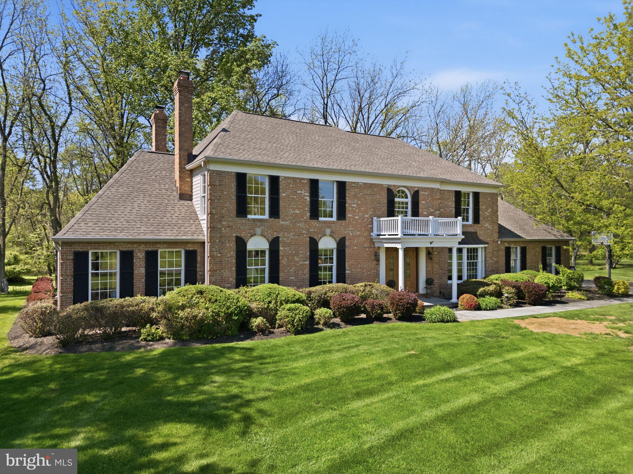 Nestled on a private wooded lot backing to a tranquil stream, this gorgeous brick Colonial offers timeless elegance and exceptional privacy, all within beautifully manicured grounds. A long, sweeping tree-lined driveway welcomes you home, while mature landscaping and meticulous lawns create a stunning first impression. Follow the bluestone pathway to the covered front entrance and step into the grand two-story foyer, where gleaming hardwood floors and a dramatic winding staircase set the tone for the sophisticated interior. Elegant picture frame wainscoting flows throughout the foyer, formal living room, and dining room, creating a refined atmosphere ideal for entertaining. The formal living room features a beautiful gas fireplace with a classic brick surround, while the adjacent first-floor office offers custom built-ins and an exposed brick accent wall, providing both warmth and character. The well-appointed kitchen is designed for both everyday living and entertaining, featuring abundant hardwood cabinetry, a center island for casual dining, custom finishes, extensive tile backsplash, double pantry, 2 dishwashers,  a Sub-Zero refrigerator, double wall ovens, a warming drawer,  built-in wine fridge in the beverage area. A bright, bumped-out breakfast area overlooks the serene wooded backyard, bringing nature indoors year-round. Flowing seamlessly from the kitchen is the spacious family room, complete with a cozy wood-burning fireplace and stately stone mantle. The sunroom is a true showstopper, featuring exposed brick and walls of windows that showcase breathtaking views of the expansive, private backyard. Completing the first floor is a dedicated laundry room, powder room, and convenient access to the attached three-car garage. Upstairs, solid wood flooring extends throughout all four bedrooms. Three generously sized bedrooms share a hall bath, while the luxurious primary suite offers a private sitting room, two oversized walk-in closets, and a spa-like ensuite bath complete with a soaking tub and skylight. The finished basement adds incredible versatility with durable LVP flooring, abundant storage space, and the potential for an additional bedroom, gym, or recreation area. Outside, enjoy peaceful outdoor living on the large composite deck that steps down to a paver patio and walkway, complete with a hot tub for year-round relaxation. The massive backyard offers exceptional privacy and endless possibilities for entertaining, play, or simply enjoying the natural surroundings. Ideally located for commuters, this exceptional home is just minutes from I-295 and close to Yardley and Newtown, offering easy access to acclaimed restaurants, boutique shopping, and year-round community events.