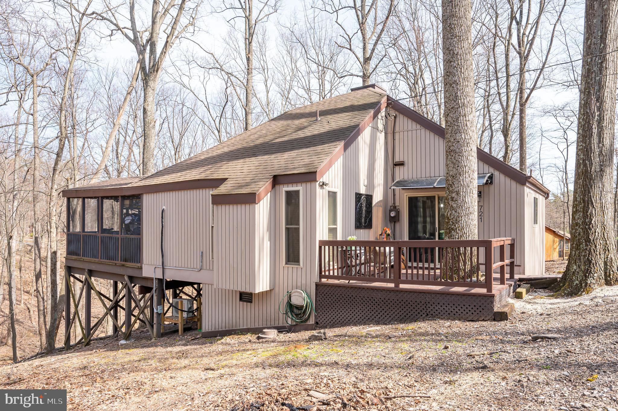 Come fall in love with this adorable home at The Woods! Nestled on a private wooded lot, you'll feel like you're on vacation as you listen to the serene sounds and sights of the back yard stream.  Spend your days watching the deer frolicking or listen to the birds sing from your private screened deck.  You'll find this home to be perfect for year-round living, a vacation home, or an investment rental. Inside, you will love the cozy open concept living space this home offers. The living room showcases a wood burning fireplace, a pellet stove, and access to the rear decks. The well-equipped kitchen boasts new cabinet paint, new butcher block counters, new lighting, a farm sink, and an island with seating space. Just off the kitchen, you will find the primary bedroom with attached recently refreshed half bathroom as well as access to the rear screened deck. A gorgeous remodeled full bathroom is also located off the main living area as well as a second bedroom with a washer/dryer hookup available. Upstairs features a third bedroom loft with plenty of storage space that overlooks the family room. This home has had many updates and upgrades over recent years to include: 50-year roof (2018), mini split system (2022), generator hookup (2021), pellet stove (2018), flooring (2021), water heater (2021), main bathroom remodel (2022), as well as updated windows, siding, and doors. Located just minutes from the Sleepy Creek Wildlife Management Area that includes almost 23,000 acres of land, a 205-acre lake, fishing, hunting, kayaking, hiking, camping, and other outdoor adventures. Class B membership is available for access to community amenities with an initiation fee.