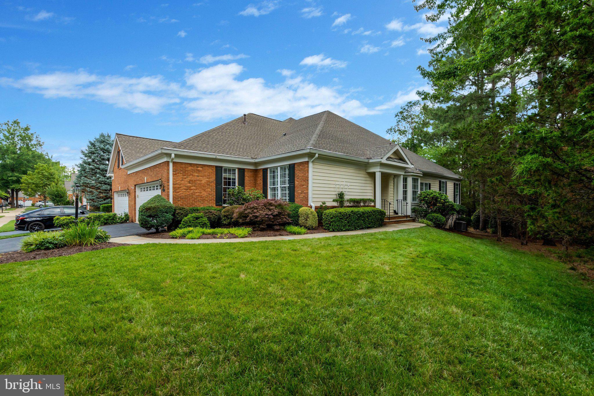 Welcome to this exceptional end-unit Glenhurst model patio home in the sought-after Regency at Dominion Valley, luxurious main-level living on a private landscaped lot with premium upgrades throughout. A beautiful paver walkway leads to the inviting covered front porch and into the elegant foyer, where hand-scraped hardwood floors extend throughout the main level. Additional custom features include plantation shutters, triple crown molding, ceiling fans, custom closet systems, and designer finishes throughout.
The formal dining room is enhanced by a stunning Waterford chandelier, while the formal living room features elegant Waterford wall sconces. The gourmet kitchen is designed for both everyday living and entertaining with granite countertops, tile backsplash, cooktop, double wall oven, upgraded cabinets with under mounted lighting, butler's pantry, and custom built-in pantry. The adjacent laundry room offers a convenient drop zone/built in pantry. The spacious family room is filled with natural light and opens through glass door to a covered deck with ceiling fans, overlooking beautifully landscaped grounds. 
The luxurious primary suite features a tray ceiling, an enormous custom walk-in closet, and a beautifully renovated spa-inspired bath with a soaking tub, oversized walk-in shower, separate heater, and designer finishes. A second main-level primary suite offers its own newly renovated en-suite bath with new cabinetry, tile, and elegant Listello trim.
The finished lower level provides exceptional flexibility with a large recreation room featuring a custom wet bar with refrigerator, an expansive office complete with built-in desk and cabinetry, two twin Murphy beds for additional guest accommodations, a full bath, cedar closet and an additional family room with French doors leading to a custom paver patio. A generous workshop with a wet sink and wood shelving provides outstanding storage and workspace. The oversized two-car garage is finished with custom-painted walls and epoxy flooring, adding a polished touch to this functional space.  Recent upgrades include renovated en-suite and second primary bathroom, 2021 water heater, roof 2025. This meticulously maintained home combines elegant craftsmanship, thoughtful custom upgrades, outstanding indoor and outdoor living spaces, and an exceptional resort-style lifestyle in one of Haymarket's premier active adult communities.
Residents of Regency at Dominion Valley enjoy an unparalleled country club lifestyle with a spectacular 30,000-square-foot clubhouse, indoor and outdoor pools, spa, state-of-the-art fitness center, aerobics studio, tennis and pickleball courts, walking and biking trails, parks, lakes, and a vibrant calendar of clubs, activities, and social events. Golf enthusiasts will appreciate the beautifully maintained Arnold Palmer-designed 18-hole Regency Course, offering an enjoyable and challenging experience for players of all skill levels, with optional golf memberships available.