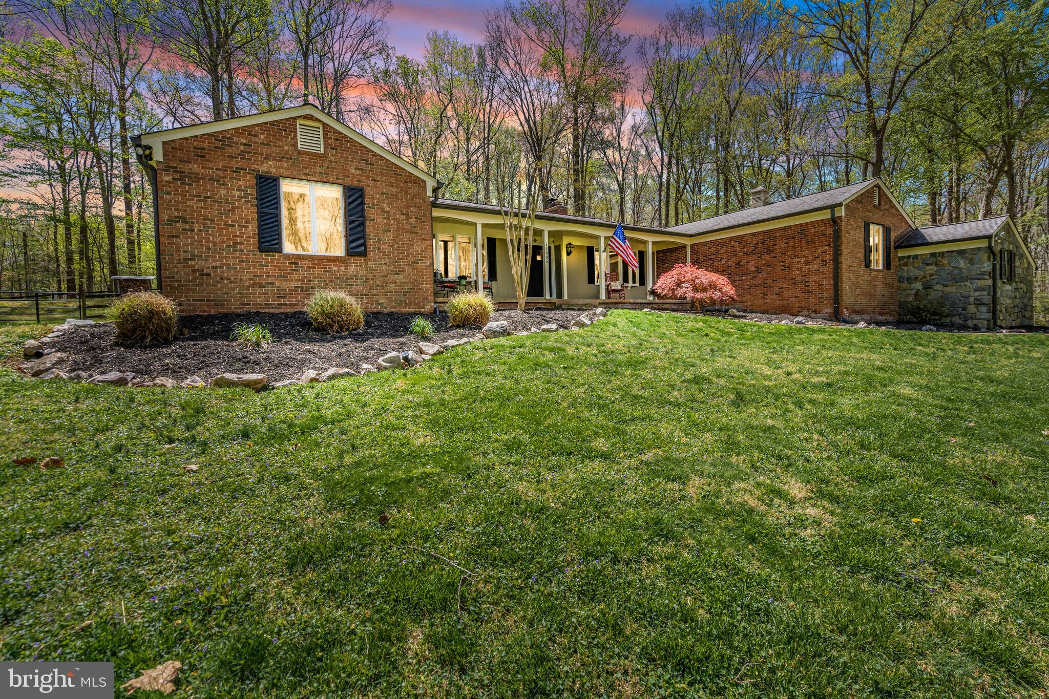OPEN HOUSE: Sunday, May 4, 1-4 PM
Discover this rare gem nestled on 5 serene acres in the peaceful, sought-after Singing Woods of Fairfax Station. A charming, private bridge crosses a scenic creek to this rare, stunning rambler, offering you a chance to own this unique piece of paradise. Inside, Brazilian hardwood floors and 2 impressive wood-burning fireplaces (with 4 back-to-back in total) give the home its warm character. Recent updates include a new HVAC system (2019), a new roof (2017), and Pella sliding glass doors in both the master suite and family room (2021), as well as new Pella front doors and garage doors (2015).

Discover cooking again in this cozy kitchen while the kitchen fireplace glows with flames.  Granite counters, a double-wall oven, huge pantry, subway tile backsplash, and large windows complete the kitchen with views of your gorgeous lot.

This spacious 3-4 bedroom, 2.5-bathroom home boasts an amazing primary suite with its own fireplace and doors leading to a private backyard patio.  Enjoy his/hers closets and a wonderfully updated primary bath.  Two other large bedroom and an hall bath with dual sinks complete the bedroom wing of this rambler.  A lower-level full bath, along with a recreation room/office/gym that the current owners have used as a non-conforming bedroom. Step out from either the master suite or family room onto the back patio, where you can enjoy the unparalleled beauty of this  expansive lot with direct access to nearby horse-riding/walking trails.  There’s also a custom drive-in shed perfect for storage or a potential workshop, plus multiple firewood storage bins around the property. The convenient, main level laundry room walks out to the backyard, with a large, oversized garage that offers additional space for storage or a gym.

The home is equipped with Andersen windows, and the concrete driveway pad outside the garage was recently replaced. Situated within the highly desirable Robinson High School pyramid, this home is in an ideal location—close to everything you need, yet you’ll feel like you’re living in the heart of the country.
