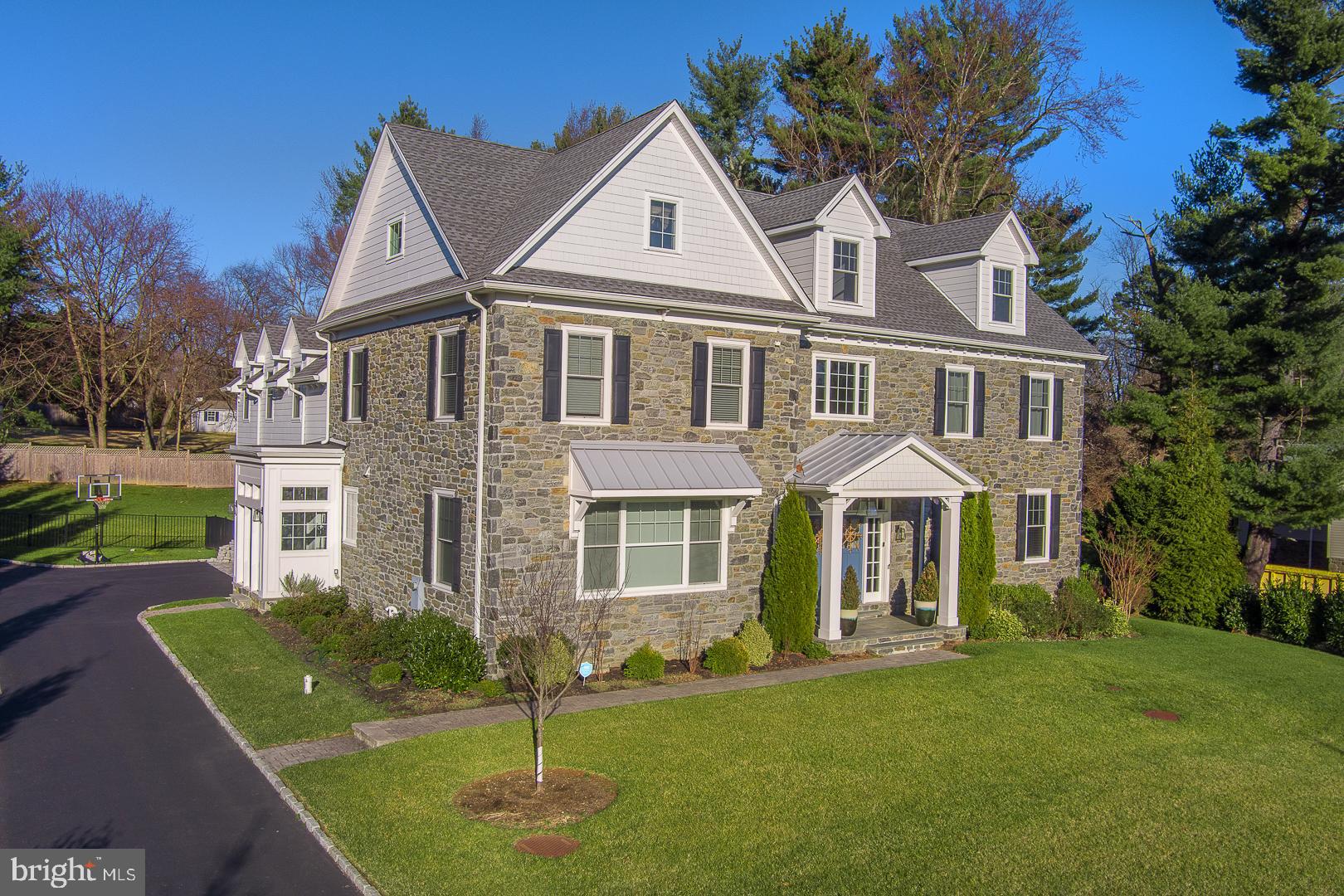 Welcome to 719 Conshohocken State Road, an exquisite Main Line colonial home that redefines luxury living. Nestled on a flat, 0.70-acre lot, this stately residence boasts six bedrooms, six full bathrooms, 1 powder room, and a generous 6,735 square feet of living space. Built just seven years ago, this stone-clad colonial masterpiece offers a perfect blend of timeless charm and contemporary elegance.
As you approach, be greeted by the double doors that open to a 2-story, light-filled foyer. A dramatic double staircase and a striking modern chandelier set the tone for the grandeur that awaits. The center hall seamlessly integrates the interior with the private backyard oasis, creating a sense of expansiveness and connection to nature.
The living spaces, adorned with subtle gray and white tones, feature generous-sized windows, gorgeous hardwood floors and French doors that invite natural light and provide views of the lush grounds. The formal living room and dining room showcase elegant yet contemporary architecture, boasting coffered ceilings, custom millwork, and large windows overlooking the front yard.
The heart of this home lies in the gracious family room, complete with a double fireplace, porcelain tile surround, custom built-ins, and French doors leading to the paver slate patio. Flowing effortlessly into the chef's kitchen, this space is designed for both functionality and style. The kitchen is a culinary dream with quartz countertops and a large quartz waterfall island, white shake style cabinets, a Thermador appliance package, chrome fixtures, breakfast nook and wonderful wet bar.  Completing the first floor is the convenient mudroom with access to the driveway, a three-car garage, and a powder room. 
Ascend the stairs to the second story, where a loft-like landing with built-in bookshelves and window seat, opens to five bedrooms, all with hardwood floors, large closets and airy interiors.  The Primary suite is a sanctuary of luxury, featuring vaulted ceilings, a sitting area, two sizeable walk-in closets, and a spa-like en-suite with a glass-enclosed shower, soaking tub, double vanity, and water closet. Four spacious bedrooms, one with an en-suite, a Jack and Jill bath, a full hall bathroom, and a large laundry room with built-in cabinets and sink finish this level.
The third floor presents a large, open second family/play room and a full bathroom. The lower level is an entertainer's paradise with numerous possibilities, including a recreation room, theater room, wine closet, fitness studio, a nanny suite with a full bathroom, a storage room, and direct access to the backyard.
Step into the ultimate outdoor retreat on the slate patio with a gas fireplace, surrounded by lush grounds and a sense of privacy and seclusion. This home is not just a residence; it's a triumph of style and sophistication that embodies the elegance and prestige for which the Main Line is renowned.
Conveniently located just minutes away from Center City Philadelphia, this home offers easy access to restaurants, shopping, parks, walking trails, and more. All of this is complemented by the distinction of being situated in the award-winning Lower Merion School District.
Experience the epitome of luxury living at 719 Conshohocken State Road – a home where every detail has been meticulously crafted to provide a lifestyle of unparalleled comfort and sophistication. Schedule your private tour today and step into a world of timeless elegance.