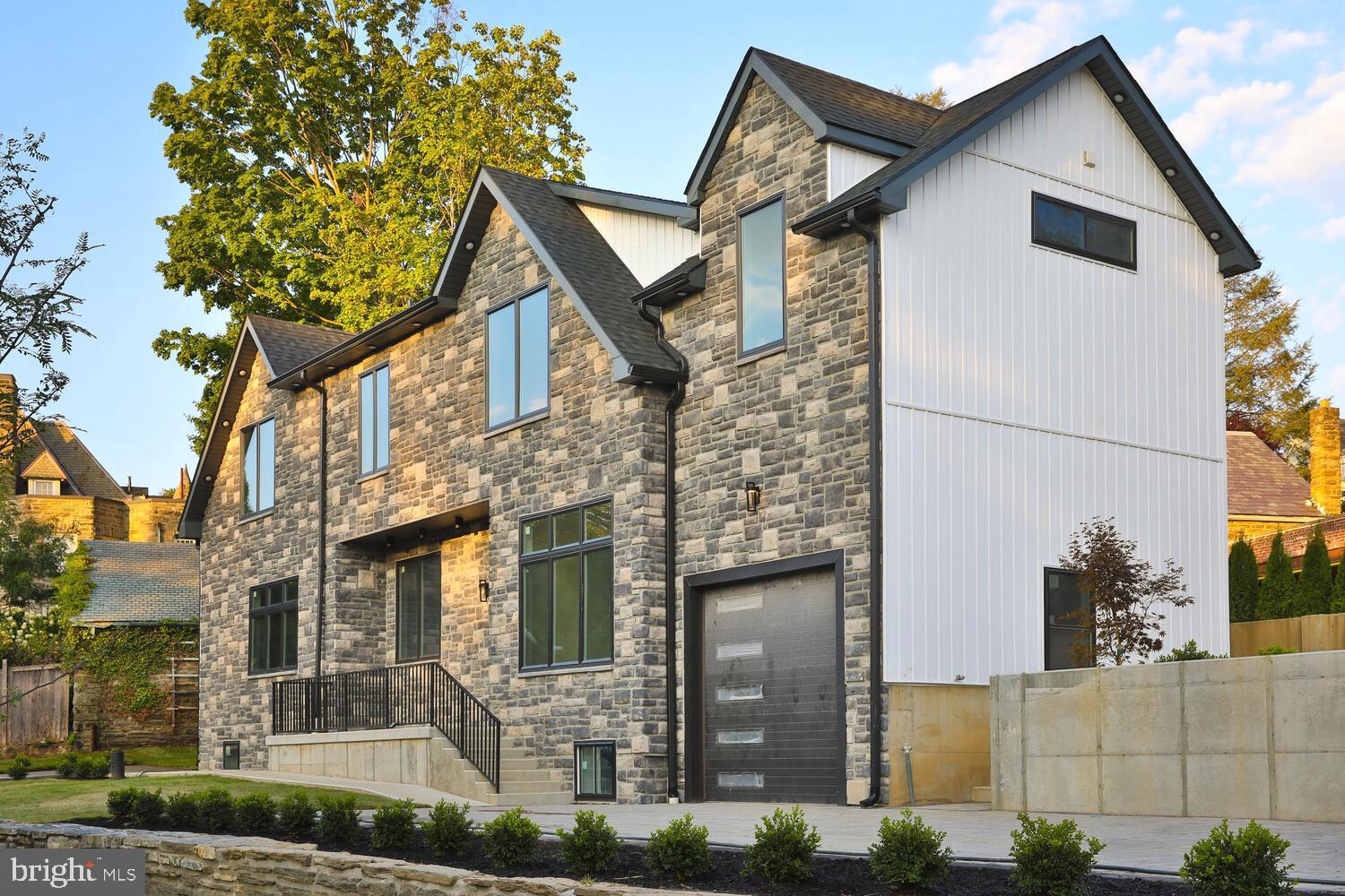 Welcome to your dream home in the heart of West Mount Airy, where historic charm meets modern luxury. This stunning new construction home, located on the grounds of the historic Nicholas-Goehring estate, is a rare find. With 5 bedrooms, 4.5 bathrooms, and a versatile study/bonus room, this home is designed with both comfort and functionality in mind.

As you approach, you'll be captivated by the elegant stone facade that complements the neighborhood's aesthetic. The extra-long and wide paver driveway, complete with a one-car attached garage, offers ample space for parking and convenience. 

Step inside through the large glass front door, and you'll be greeted by an open-concept foyer and living space bathed in natural light. The minimalist design, accented with sleek black hardware and Brazilian hardwood floors, exudes modern sophistication. The staircase, with its black metal railings and glass panels, serves as a striking centerpiece that spans from the basement to the second floor.

The heart of the home is the chef's kitchen, featuring custom two-tone cabinets, Dekton countertops, and top-of-the-line appliances, including a Cafe double-oven and a Sharp built-in microwave. The island, with seating for four, offers additional storage and a perfect spot for casual meals.

The living and dining areas are designed for both relaxation and entertainment, with a custom space for a recessed TV and fireplace, built-in ceiling speakers, and a stylized soffit with custom lighting that adds depth and definition to the space. A slider leads to the backyard, which has an elevated paver patio, a living fence, and a landscaped garden area, creating a serene outdoor retreat.

The basement is a showstopper with its exposed brick wall, 12' high ceilings, and large windows that flood the space with light. This suite includes a large bedroom, a bathroom with a walk-in shower, custom built-in shelving, and a dry bar with a mini fridge. 

The second floor offers a laundry room, powder room, and three bedrooms, including an ensuite. The primary suite is a luxurious haven, with a spacious bedroom, large windows, and a spa-like bathroom featuring a soaking tub, a glass-enclosed shower with dual shower heads, and a double sink. The custom walk-in closet with built-ins completes this exquisite suite.

This home is equipped with wireless internet boosters and smart lighting, ensuring every modern convenience is at your fingertips. The developer's dedication to quality construction and customer satisfaction guarantees that this home will exceed your expectations. Buyers can customize this home further with an add-on media package that would include TV and fireplace installation for the living room, primary suite, and basement, as well as the option to add a washer and dryer.

Don't miss the opportunity to own a piece of history reimagined for contemporary living in one of Philadelphia's most desirable neighborhoods.