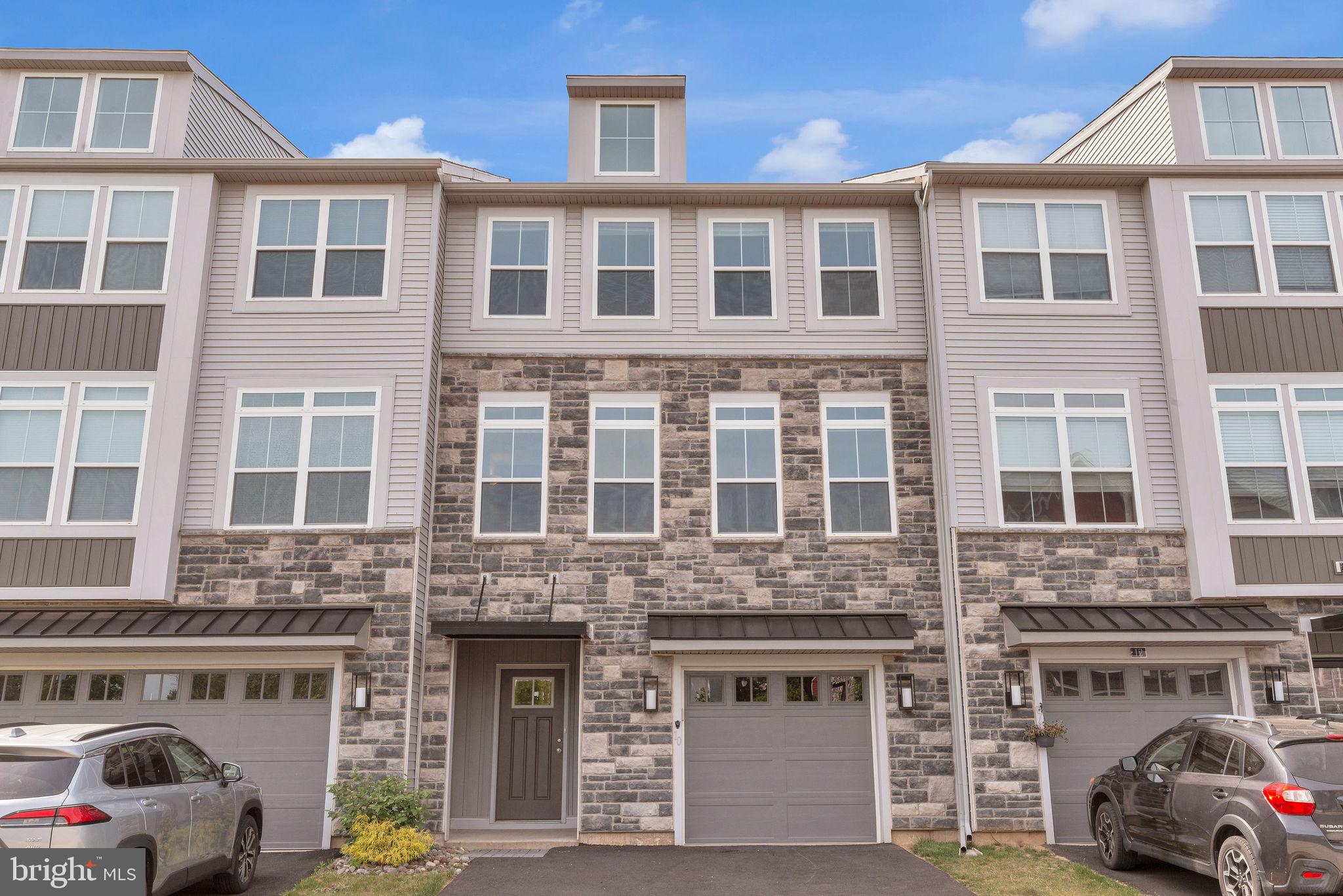 Welcome to modern luxury and effortless living at The Fields at Constitution Square! Built in 2022, this stunning 3-story townhome perfectly blends contemporary architecture with the warm charm of Bucks County. Boasting a striking stone-and-vinyl facade, an attached garage, and a sprawling, light-filled layout, this pristine home looks and feels brand new. Step up into a spectacular, sun-drenched main level designed with entertaining in mind. The gourmet kitchen serves as the focal point of the home, featuring rich chocolate-espresso cabinetry, premium granite countertops, a classic white subway tile backsplash, a sleek stainless steel appliance package, and a massive center island that serves as the perfect prep station and casual breakfast bar. A wide-open, seamless transition leads from the kitchen into expansive living and dining areas where warm, wood-look luxury flooring stretches across the entire level, anchored by beautiful 9-foot-plus ceilings, modern light fixtures, and walls of windows that flood the home with natural light, complete with remote controlled shades you can utilize with the touch of a button. Walk into your sunroom with bonus bump-out space conveniently near the kitchen and slide open the glass doors to your private upper-level deck, which offers an exclusive layout that makes it the only deck in the entire community to boast this level of privacy—ideal for morning coffee, evening cocktails, or grilling while overlooking peaceful, mature treetops without any rear neighbors looking in. The top floor hosts the tranquil sleeping quarters, complete with neutral carpeting and bright windows. The generous primary suite is a true sanctuary featuring an expansive bedroom layout, a large walk-in closet, an elegant ensuite bathroom with a dual-sink vanity and modern glass-enclosed shower, and a separate sitting room complete with a structural bump-out for added space and architectural detail. Generously sized secondary bedrooms offer great closet space and flexible options for a dedicated home office, nursery, or guest rooms, while a dedicated upper-floor laundry room makes chore day a breeze. On the ground floor, you will find an inviting foyer entrance, seamless access to the spacious garage, and a versatile downstairs bonus room with a half-bath featuring a beautiful space that radiates with natural light. This flexible lower-level area can be easily customized to fit your lifestyle, whether you need a secondary living room, a home gym, a media room, or a private home studio. Nestled in the highly sought-after Pennridge School District, this community offers a peaceful neighborhood vibe with fantastic walkability and close proximity to Perkasie’s vibrant historic downtown, local parks, jogging paths, boutique shopping, and craft breweries. Don't miss the chance to make this turn-key, contemporary masterpiece your own—schedule your private tour today!