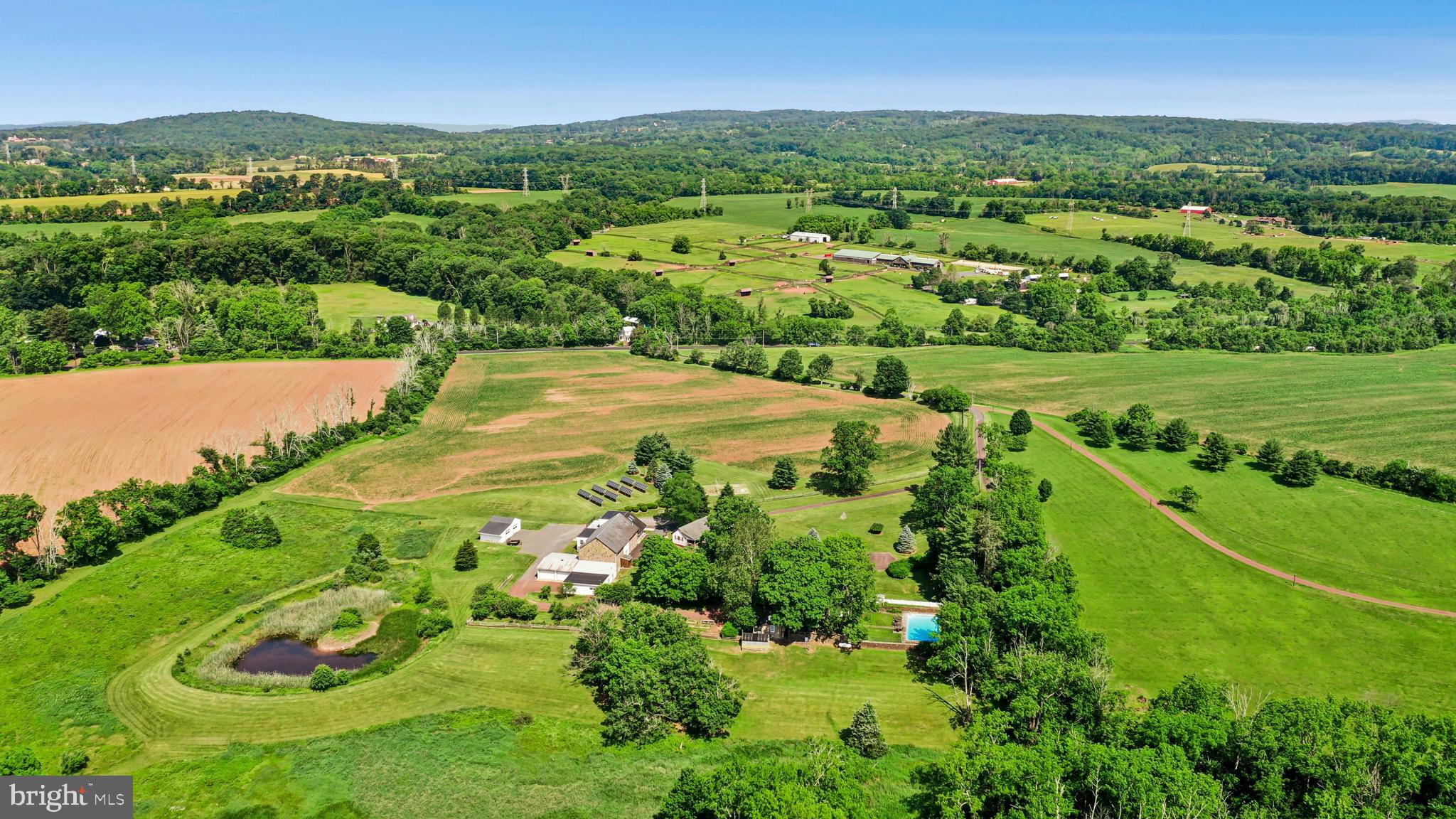 This stunning 150 acre Bucks County gentleman’s farm is the perfect family compound, weekend getaway or full-time estate. The main house, guest house and converted barn present an unparalleled opportunity in the picturesque Pleasant Valley … whose name was suggested by location after the William Penn 1737 Walking Purchase. Set well off the road at the end of a tree-lined drive, the land unfolds in layers of open, tillable ground and verdant woodlands, framed by the pristine Cooks Creek, and traversed by bridges and trails. A seasonal chorus of birds, deer and wild turkey creates acreage best described as a living landscape.
     The main home on the estate is a circa 1850 classic stone farmhouse. Updated over the years by conscientious stewards, the home’s modern conveniences have been tastefully and carefully blended with many original features. One former owner, a play and screen writer, shared weekends at his farm with Alfred Hitchcock and other notables. Things of culture, grace and romance abound.
     A stone settler’s cottage, breakfast room, formal dining room, living room and expansive sunroom boast walls of windows that overlook a party-sized terrace with stone walls and a canopy of trees. Surrounded by a white picket fence, the inground pool is just steps away and beckons on a warm summer day. Outdoor entertaining can be casual or elegant, intimate or grand - all the amenities are here.
     Family and friends will enjoy the guest house, fully independent from the main house. Vaulted ceilings frame cozy rooms that include a sunroom, office, two bedrooms and two baths. For those who love the magic of gardening, the property also features a greenhouse, a flourishing orchard, and raised garden beds.
     Preserving the farm’s history, the landmark 1800s stone bank barn was renovated and expanded in 2016 and offers extraordinary opportunities and flexibility for offices, studio space, home schooling, parties and hobbies. A two-story great room with exposed beams, stone walls and barn ladder attest to the barn’s legacy. The reimagined and expanded spaces include a full kitchen, two powder rooms, full bath, conference room, reception room and five offices.
     For all your vehicles, toys, equipment, and hobbies, the property offers an oversized three-car garage, a fully outfitted equipment garage with cabinetry and a workstation, plus an additional detached two-car garage.
     Embrace a country home without sacrificing convenience. Located just 20 minutes from the Saucon Valley Country Club, the Pennsylvania Turnpike, I-78, and New Jersey. New York City is ninety minutes and Philadelphia one hour. Savor the splendor of nature’s elegance and serenity with an abundance of privacy. Enjoy the luxury of unhurried comfort, peace, privacy and tranquility, interrupted only by nature’s wonderful sights and sounds.   Available on 37.5 acres for $3,950,000