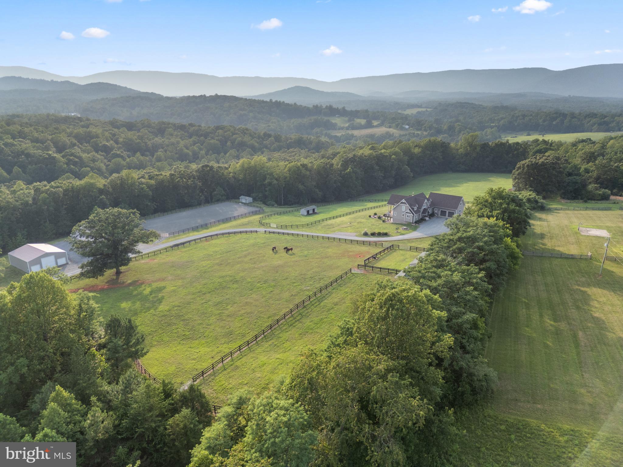 Set on nearly 80 private acres just outside Charlottesville, Virginia, this exceptional equestrian estate offers the perfect blend of refined country living, thoughtfully designed equestrian amenities, and breathtaking natural beauty. The custom-built mountain residence enjoys sweeping 270-degree mountain views and showcases stunning red oak timber-frame accents throughout the main living spaces.
Designed for both everyday comfort and effortless entertaining, the home features four spacious bedrooms, each with a walk-in closet, four full baths, and two half baths. The walk-out lower level includes a spacious bedroom with full bath, game room, half bath, family room, and opens to a covered patio complete with a recently installed outdoor kitchen and fire pit. Additional highlights include 10-stall barn, an oversized two-car garage with unfinished bonus space above, an expansive mudroom with built-in cubbies, a generous laundry room, indoor/outdoor dog kennels, and a large equipment storage barn.
The open-concept floor plan is filled with natural light, anchored by an impressive wall of windows and oversized picture windows that frame spectacular mountain vistas from nearly every room. At the heart of the home, a striking Tulikivi soapstone fireplace provides luxurious radiant warmth throughout the winter months.
The chef’s kitchen is equally impressive, featuring a 60-inch Viking double-oven range with six gas burners, griddle, grill, dual oversized convection ovens, a large breakfast bar with seating for four, and an oversized walk-in pantry with abundant storage for small appliances and provisions.
Built with quality and efficiency in mind, the home offers spray foam insulation, energy-efficient windows, a two-zone HVAC system, solid-core doors throughout, dual propane on-demand water heaters, and a radon mitigation system installed during construction. The durable Hardie Plank board-and-batten exterior and 50-year architectural roof provide years of low-maintenance ownership.
Equestrians will appreciate the property’s exceptional horse facilities. The custom center-aisle barn includes ten stalls, featuring six oversized 12’ x 18’ foaling stalls and four 12’ x 12’ stalls outfitted with Nelson automatic waterers and built-in fans. Inviting wash stall areas with hot/cold water,. The well-appointed tack room offers ample space for tack, trunks and equipment. Laundry room and dedicated feed space is always a must. Horses enjoy expansive fenced pastures with spacious 10’ x 28’ run-in sheds and automatic geothermal Miraco waterers. 
Adjacent to the barn is a professionally designed 100’ x 200’ all-weather riding arena, suitable for dressage, hunter/jumper, and any other discipline. Fully enclosed with classic three-board fencing, the arena includes dressage letters and jumps and is ready for immediate use. A nearby 42’ x 48’ storage barn provides ample space for hundreds of bales of hay, shavings, tractors, and additional equipment.
Beyond the equestrian amenities, the property offers endless opportunities to enjoy the outdoors. Acres of mature hardwood forest provide exceptional trail riding, hiking, ATV exploration, and abundant wildlife viewing, with frequent sightings of deer, turkey, bald eagles, fox, coyote, and black bear. A picturesque year-round stream meanders through the property, while a flourishing orchard produces multiple varieties of apples, peaches, pears, figs, and mulberries.
Even four-legged family members are exceptionally accommodated. The heated and cooled indoor/outdoor kennel features four interior runs with dog doors leading to two large, separately fenced outdoor exercise areas enclosed by six-foot black chain-link fencing.
Move-in ready and thoughtfully designed for both family living and equestrian pursuits, this remarkable estate offers privacy, exceptional craftsmanship, and an unparalleled lifestyle—all with no HOA or restrictive covenants. Possible division potential.